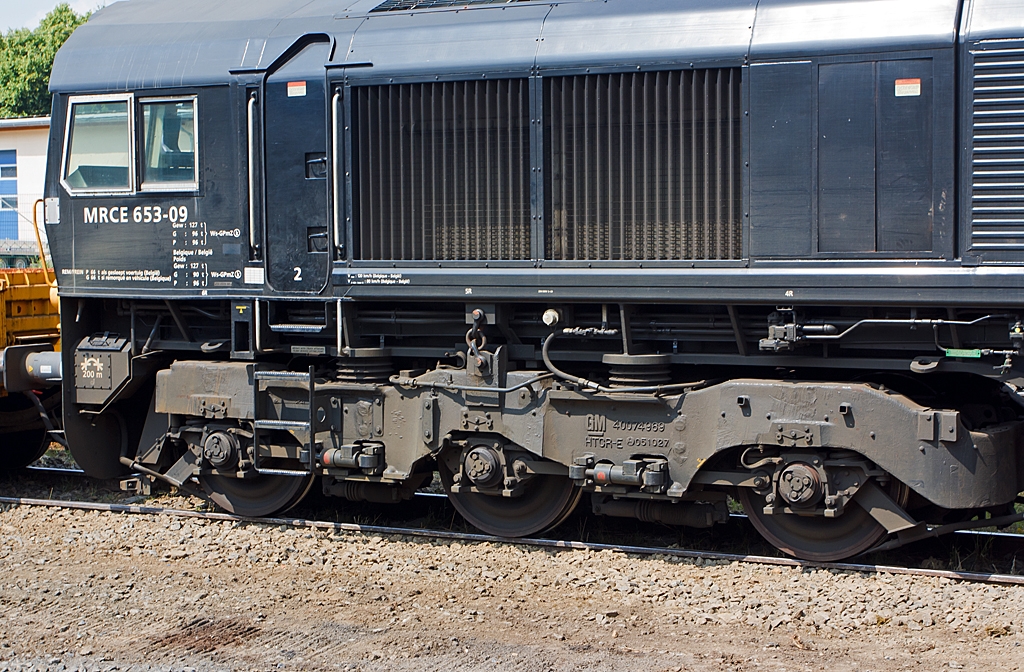 Detail eines mchtigen dreiachsigen HTCR-E Drehgestelles der Class 66.
Hier der MRCE 653-09 (92 80 1266 119-7 D-DISPO) eine EMD JT42 CWRM (Class 66/9) am 13.07.2013 in Ehringshausen (Lahn-Dill-Kreis).
Die dreiachsigen HTCR-E Drehgestelle verfgen ber gegenlufig radialgelenkte Endachsen, die Mittelachse ist seitenverschiebbar, diese ermglichen den Betrieb dieser insgesamt 6-achsigen-Lokomotive (sie haben 2 Drehgestelle) auf Strecken die in der Regel auf 4-achsige Lokomotiven eingeschrnkt sind.

Weitere Vorteile sind:
- Kleinster befahrbarer Radius der Lok ist so 80 m
- Die seitlichen Schiene-Krfte sind dadurch auch gesenkt
- Geringere Gefahr von Entgleisungen
- Reduzierter Verschlei der Komponenten, somit erstreckt sich das Drehgestell berholungsintervalle auf 1,6 Mio. km