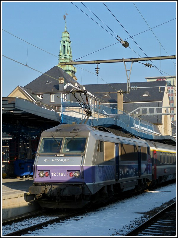 Entgegen unseren Befrchtungen nur noch orange farbene Loks vor dem IC 91 Vauban in Luxemburg zu sehen, war heute (01.02.2012) eine von Stefans Lieblings-Sybics zu Gast. Eine von den sechs BB 26000 im schnen  en voyage  Design zog heute den IC Vauban von Luxembourg nach Basel. Insgesamt gibt es 234 Loks dieses Typs bei der SNCF und sie lsten zum Fahrplanwechsel am 12.12.2011 die Loks der Srie BB 15000 (nez casss) vor der beiden Intercitys 90/91 Vauban und 96/97 Iris ab. 

Hier noch einige Informatinen zu der SNCF Srie BB 26000: Die SYBIC ist vornehmlich aus Stahl gefertigt und besitzt aufgrund ihres futuristisch-kantigen Designs eine sehr eigene Erscheinung. Besonders bemerkenswert mit Blick auf ihre Konstruktion ist die Tatsache, dass sie, wie bereits einige frhere franzsische E-Loks, so genannte Monomoteur-Drehgestelle besitzt, in denen jeweils nur ein groer Fahrmotor ber eine nachgeschaltete Getriebeeinheit alle Achsen des jeweiligen Drehgestells antreibt. Die Zugkraftbertragung zwischen Lokkasten und Drehgestellen erfolgt ber tief liegende Zug- und Druckstangen, whrend die Primrfederung auf Schraubenfedern und die Sekundrfederung auf Gummi-Stahl-Blcken beruht. Die Kraftbertragung vom jeweiligen Fahrmotor bzw. vom Verteilergetriebe auf die Radstze erfolgt ber Hohlwellen-Gummiringfeder-Antriebe. 

Im elektrischen Teil kommen bei der SYBIC auf GTO-Thyristoren basierende Traktionsstromrichter zur Anwendung, welche flssigkeitsgekhlt sind. Diese arbeiten mit einer Zwischenkreisspannung von 1,5 kV Gleichstrom und knnen somit whrend des Betriebs im franzsischen Gleichstromnetz ohne weiteres direkt aus der Oberleitung gespeist werden. Im Wechselstromnetz ist ihnen der Haupttransformator vorgeschaltet. 

Auf dem Dach sind zwei unterschiedliche Stromabnehmer angebracht, jeweils einer fr Gleichstrom (mit vier Schleifleisten) und Wechselstrom (mit zwei Schleifleisten). Fr die Bedienung stehen dem Lokfhrer eine einfache manuelle Zug- und Bremskraftsteuerung, das so genannte  dispositif de vitesse impose  (eine Geschwindigkeitssteuerung hnlich der deutschen AFB, aber ohne Koppelung mit der pneumatischen Bremse) und als Hilfe fr den Betrieb im 1,5-kV-Netz eine Leistungsbegrenzung zur Limitierung der Stromaufnahme zur Verfgung. Bedienelemente fr direkte und indirekte Bremse sind ebenfalls vorhanden. Die SYBIC besitzt Bordgerte fr die Zugsicherungssysteme RS bzw.  Crocodile  und KVB. 

Die BB 26000 ist unter dem Kunstnamen  SYBIC  gut bekannt, dieses wurde aus  synchrone  fr die Synchronmotoren und  bicourant  fr die Zweisystemfhigkeit gebildet. (Jeanny)
