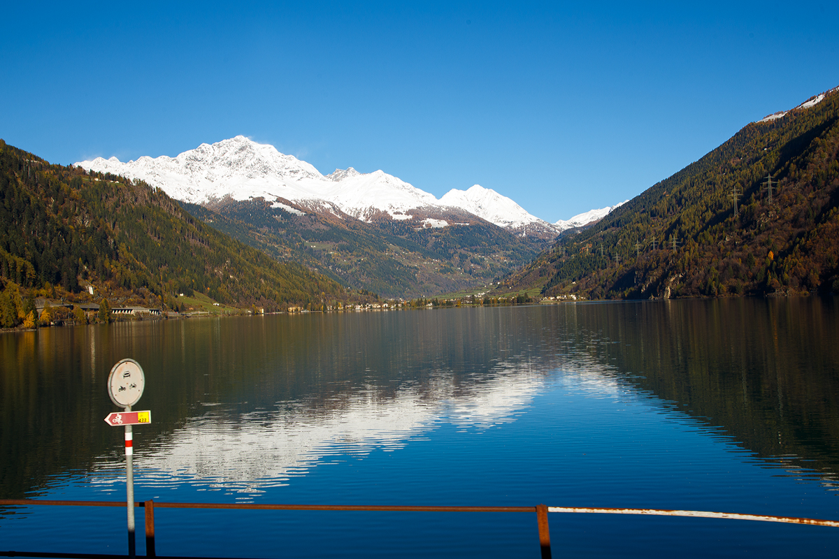 
Aus dem Zug heraus am 04.11.2019 in Miralago (deutsch: Seeblick) im Puschlav ein Seeblick über den Lago di Poschiavo hinweg auf die Berninagruppe. Die höchste Bergspitze ist der mit 4.049 m ü. M. hohe Piz Bernina, der einzige Viertausender der Ostalpen.

Hier links am westlichen Ufer des Sees entlang führt, auf einer Länge von 2 km, die in die Liste des UNESCO-Weltkulturerbes aufgenommen Berninabahn.
