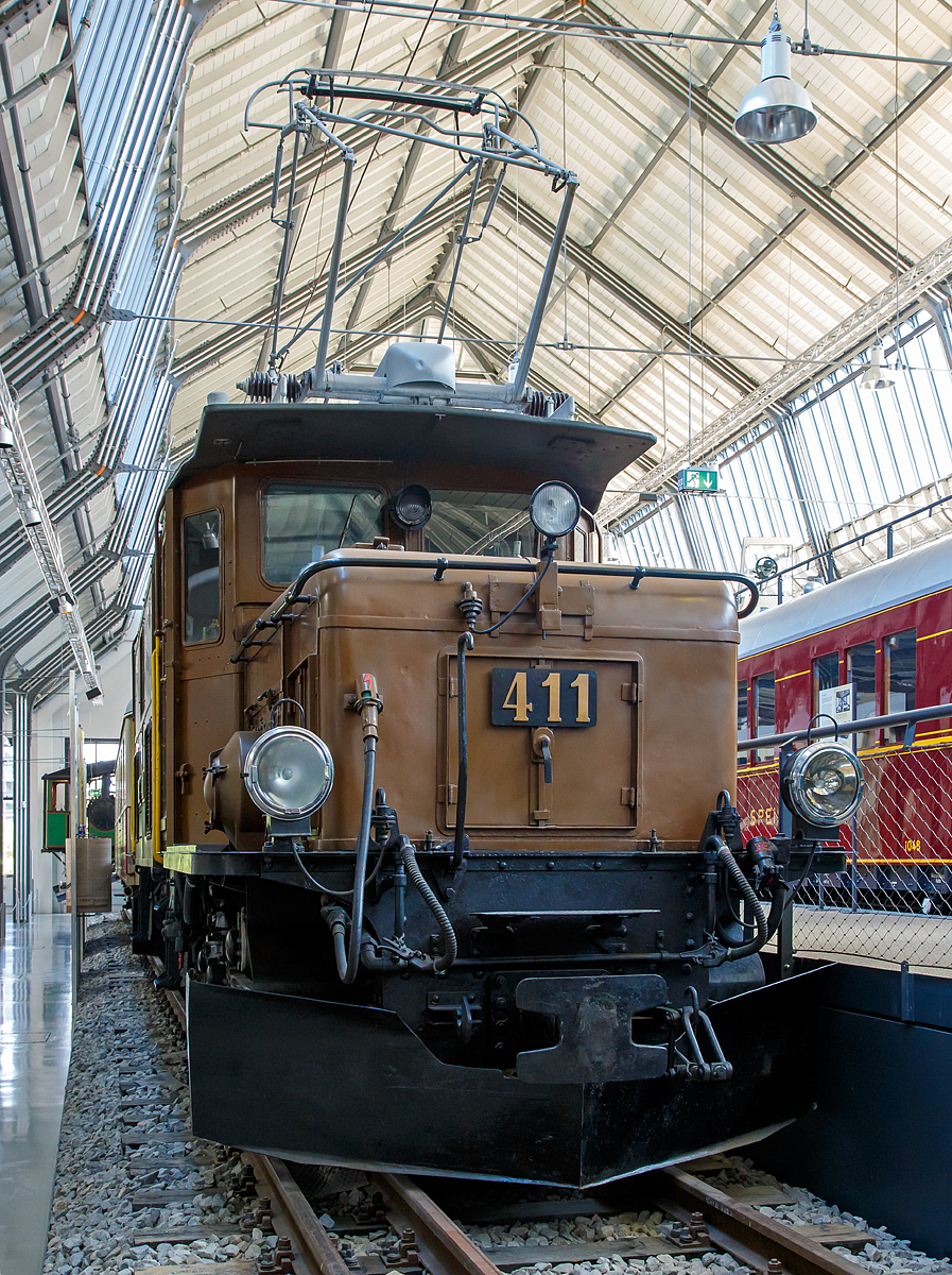 
Das Rhätisches Krokodil 411 bzw. die RhB Ge 6/6 I 411, ausgestellt im Verkehrszentrum des Deutschen Museums in München (Theresienhöhe), hier am 16.06.2018.

Die Ge 6/6 I ist eine Elektrolokomotivbaureihe der Rhätischen Bahn (RhB). Wegen ihrer Form und Konstruktion – sie ähneln den SBB-Krokodilen der Gotthardbahn – werden die C'C'-Lokomotiven von Eisenbahnfreunden auch Rhätisches Krokodil genannt, RhB-intern ist C-C die geläufige Bezeichnung.

Die Ge 6/6 I Rh.B. 411 wurde 1925 von A.G. Brown, Boveri & Cie. (Fabrik-Nr. 2241), der Schweizerische Lokomotiv- und Maschinenfabrik Winterthur (Fabrik-Nr. 3344), sowie der Maschinenfabrik Oerlikon gebaut.

Die fortschreitende Elektrifizierung des RhB Stammnetzes mit Einphasenwechselstrom (11 kV, 16 2/3 Hz) zwang die RhB Anfang der 20er Jahre des vergangenen Jahrhunderts zur Beschaffung leistungsfähiger Elektrolokomotiven.
1921 konnten die ersten sechs sechsachsigen Lokomotiven des Typs Ge 6/6 in Betrieb genommen werden. Diese Fahrzeuge, die seinerzeit als die leistungsstärksten Schmalspurlokomotiven der Welt galten, verdrängten schnell die Dampflokomotiven auf der Albulalinie. 1924 konnten vier, 1925 weitere zwei und schließlich 1929 nochmals drei Lokomotiven dieses Types in Dienst gestellt werden.
Mit Auslieferung der Ge 4/4 I und Ge 6/6 II wurden die als Rhätisches Krokodil bekannten Ge 6/6 I in den Güterzugdienst abgeschoben. Dennoch prägten diese Fahrzeuge über Jahrzehnte das Bild der RhB und gelten daher bei vielen Fans noch heute als die RhB-Lokomotive schlechthin.
Erst mit Verfügbarkeit der zweiten Serie der Ge 4/4 II wurde ein Großteil der Krokodile entbehrlich. Nur noch drei Exemplare verblieben auf dem Netz der RhB und stehen noch heute hauptsächlich für Sonderfahrten zur Verfügung.

Das eine oder andere RhB Krokodil blieb der Nachwelt als Denkmallokomotive erhalten. Lok 402 ist seit 1985 im Verkehrshaus der Schweiz in Luzern ausgestellt. Die Nummer 407 stand viele Jahre lang vor einem Zürcher Bankhaus. Sie wurde jedoch wieder nach Graubünden verfrachtet und steht heute auf einem Denkmal in der Nähe des Bahnhofs Bergün. Lok 406 wurde 1984 auf dem ehemaligen ABB Areal in Zürich Oerlikon aufgestellt und später im Werk Pratteln ausgestellt. Dieses äußerlich sehr gut erhaltene Exemplar ist leider nicht der Öffentlichkeit zugänglich. Nummer 413 wurde 1996 verschrottet. Nach einem Rangierunfall wurde die Ge 6/6 411 zusammen mit dem Salonwagen As 1154 im Juni 2001 an das Deutsche Museum in München als Leihgabe abgegeben.

TECHNISCHE DATEN der RhB Ge 6/6 I (Rhätisches Krokodil):
Betriebsnummern: 401 - 415
Hersteller - Kasten und Drehgestelle: SLM
Hersteller - Elektrik: BBC, MFO
Inbetriebsetzung: 1921 - 29
Anzahl Fahrzeuge: 15 (betriebsfähig 2, erhalten 6)
Spurweite: 1.000 mm
Achsanordnung: C'C'
Länge über Puffer: 13.300 mm
Breite: 2.650 mm
Drehzapfenabstand: 5.670 mm
Achsabstand im Drehgestell: 3.275 mm
Triebraddurchmesser (neu): 1.070 mm
Dienstgewicht: 65,9 t
Höchstgeschwindigkeit: 55 km/h
Anzahl Fahrmotoren: 2 vom Typ ELM 86/12
Getriebeübersetzung: 1 : 4,134
Max. Leistung am Rad: 940 kW
Stundenleistung: 794 kW (1076 PS)
Max. Zugkraft am Rad: 195 kN
Dauerzugkraft am Rad: 115 kN
Anhängelast: bei 45 ‰ 160 t / bei 35 ‰ 220 t
Fahrleitungsspannung: 11 kV, AC 16,7 Hz