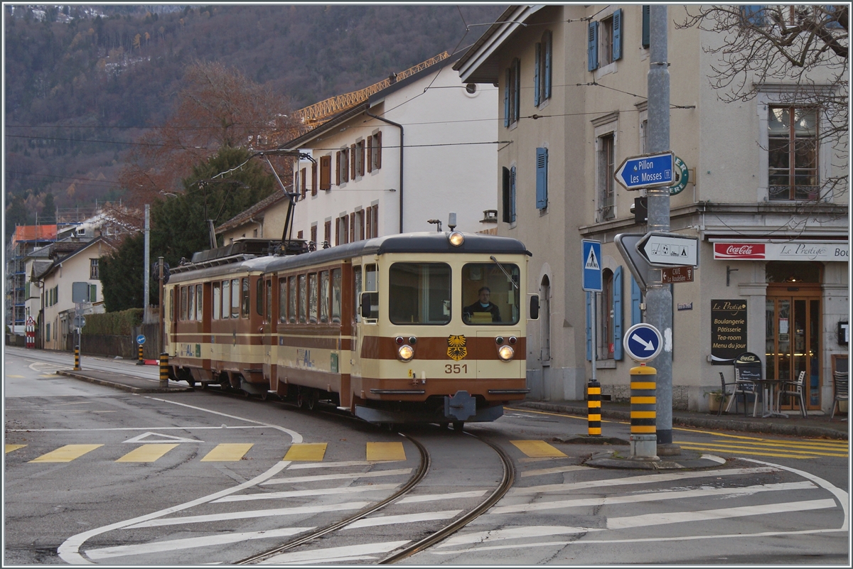 Der A-L Regionalzug 329 von Leysin nach Aigle bestehend aus dem Bt 351 und dem BDeh 4/4 302 haben den Halt Aigle-Place-du-March verlassen und berqueren nun eine Kreuzung um dann durch die Altstadt zum Bahnhof von Aigle zu kommen. 

5. Dezember 2021