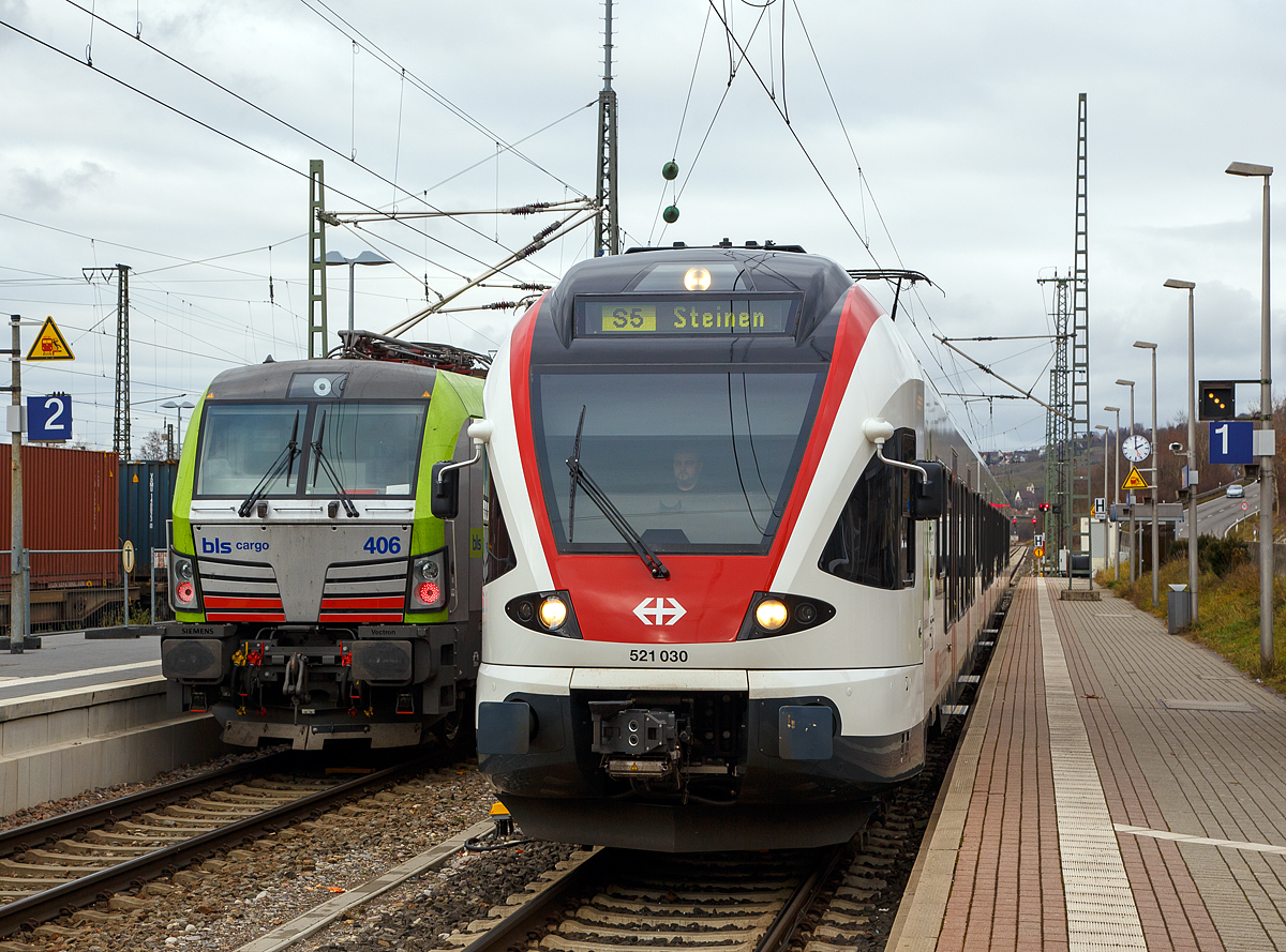 
Der Stadler Flirt RABe 521 030   Rpublique et Canton du Jura  der SBB GmbH steht am 28.12.2017 im Bahnhof Weil am Rhein, als S5 nach Steinen via Lrrach, auf Gleis 1 zur Abfahrt bereit. Er befhrt die Bahnstrecke Weil am Rhein–Lrrach  Gartenbahn  (KBS 734) und ab Lrach die  Wiesentalbahn  (KBS 735). 

Auf Gleis 2 fahren gerade zwei Re 475 der BLS Cargo durch.