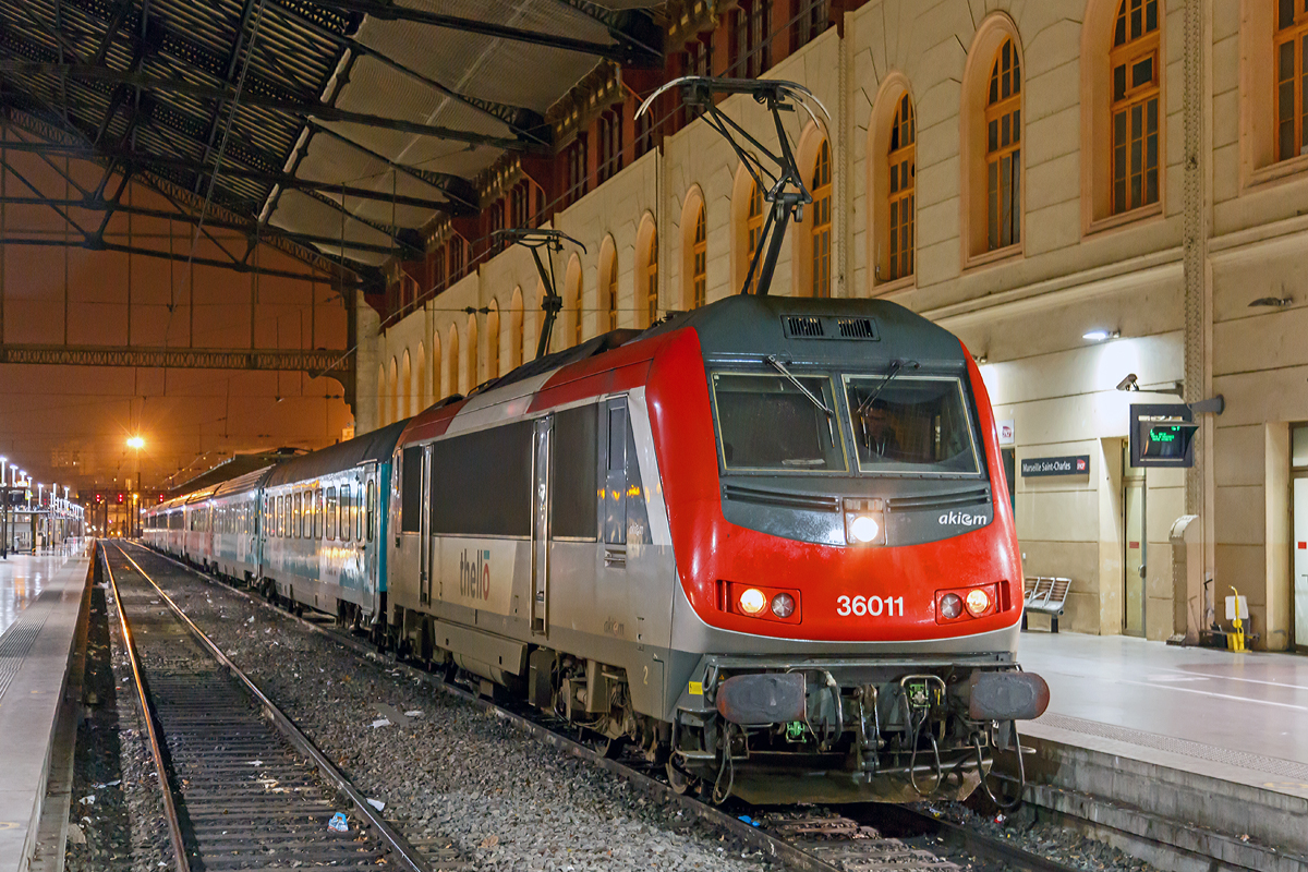 
Die Akiem 36011 (91 87 0036 011-1 F-AKIEM), eine Alstom BB 36000  Astride  (Asynchron Tricurrent Drive Engine), ist am 24.03.2015 gerade (um 22:29 Uhr) mit dem Thello EC 159 / EC 160 (Mailand - Genua  - Monte-Carlo - Niza - Toulon - Marseille-St-Charles) in den Endbahnhof Marseille St-Charles eingefahren.

Die BB 36000 ist eine Baureihe von elektrischen Lokomotiven der SNCF, mit dem Kosename  Astride  (Asynchron Tricurrent Drive Engine). Gebaut von Alstom (ehem. GEC-Alsthom), reihen sie sich ein in die Kategorie der europäischen asynchronen Mehrsystem-Lokomotiven. Mit ihren  großen  Schwestern, den BB 26000  Sybic  zählen sie zu den stärksten Lokomotiven der SNCF.

Die Astride besitzen drei unterschiedliche Stromabnehmer (1,5 kV Gleichstrom, 3 kV Gleichstrom und 25 kV 50 hz Wechselstrom). Diese Loks können in Belgien, in Luxemburg, in Italien, in Frankreich und neuerdings sogar in den Niederlanden verkehren. So sollte ein Lokwechsel an den Grenzen vermieden und eine Menge Zeit eingespart werden.

Nach der Bestellung von 264 Lokomotiven der Baureihe BB 26000  Sybic  entschied sich die SNCF für einen Kontraktwechsel. Daher bekamen die letzten 30 Neubau-Lokomotiven eine Drehstromausrüstung mit Asynchron-Motoren. Doch niemand zeigte Interesse an den neuen Loks. Genau zum selben Zeitpunkt wurden nämlich der Personenverkehr vom Güterverkehr bei der SNCF getrennt. Für den Personenverkehr wurde der TGV in den Focus gestellt und die meisten internationalen Nachtzüge abgeschafft. Der Güterverkehr zeigte auch kein Interesse an dieser polyvalenten Lok. Ebenfalls zu diesem Zeitpunkt, begann Alstom mit der Entwicklung der Prima, von der sie sich höhere Renditen erhoffte, sowohl in Frankreich, als auch im Ausland. Unter diesen Umständen war es schwer für die „Astride“ sich durchzusetzen, zu allem Übel litt sie auch noch lange unter verschiedenen Kinderkrankheiten.

Die insgesamt 60 gebauten BB 36000 „Astride“ wurden zwischen 1996 und 2002 ausgeliefert. Sie können eine gewisse Familienzugehörigkeit mit den BB 26000 nicht verleugnen, auch wenn die Ecken etwas abgerundet wurden und sie aerodynamischer ist, als die Sybic.

Obwohl sie Personenzüge mit 200, ja sogar 220 km/h ziehen kann, so wurde die „Astride“ doch vorwiegend im Güterverkehr zwischen Belgien und Italien eingesetzt. Dort ist ihre Geschwindigkeit allerdings auf 120 km/h begrenzt.

Im Oktober 2011 kamen die Loks mit den Nummern BB 36001,2,4,5,7,11 und 15 zu Akiem. Sie behielten zwar ihre  livrée multiservice , haben aber das SNCF Logo verloren. Drei von diesen Loks (BB36007, BB36011, BB36015) wurden bis 200 km/h getestet und fahren jetzt im internationalen Personenverkehr zwischen Paris und Venedig, sowie Marseille und Mailand. Diese Verbindungen werden von Thello, einer Tochtergesellschaft von Veolia betrieben.

Technische Daten der Baureihe BB 36000  Astride :
Betriebsnummern : 36001-36030, die 36331-36360 Italien tauglich, Mehrfachtraktion
Hersteller: GEC-Alsthom
Spurweite: 1.435 mm
Bauart: Bo'Bo'
Stromsystem: 1.500 V DC; 3.000 V DC und 25 kV, 50 Hz AC
Baujahre: 1996-2002

Länge über Puffer: 19.110 mm
Achsabstand im Drehgestell: 3.000 mm
Drehzapfenabstand: 10.400 mm
Breite: 2.926 mm
Höhe: 4.270 mm
Dienstgewicht: 89 t
Triebraddurchmesser (neu): 1.150 mm
Höchstgeschwindigkeit: 200 km/h (wenige 220 km/h)
Dauerleistung: 5.600 kW
Anfahrzugkraft: 320 kN
Anzahl der Fahrmotoren: 4 (4 FXA 4559 Alstom Asynchronmotoren mit Zwangsbelüftung)
