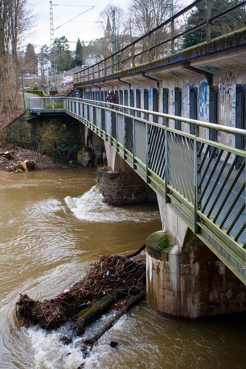 Die vom Hochwasser beschädigte Eisenbahn-Siegbrücke mit Fußgängersteg in Kirchen (Sieg), der Siegstrecke (KBS 460), hier am 03.01.2024.

Die Bahnstrecke Siegen - Köln wird zwischen Kirchen und Betzdorf bis min. Ende nächster Woche gesperrt bleiben. Das hat die Deutsche Bahn Dienstagnachmittag mitgeteilt. Durch das Sieg-Hochwasser gibt es Schäden an einer Eisenbahnbrücke in Kirchen (kurz vorm Bahnhof). Aufgrund der Wetterlage und der weiterhin anhaltenden Regenfälle sei die Sperrung erforderlich, so die Bahn-Pressestelle. Die Züge des RE 9 können wegen der Streckensperrung nur bis Betzdorf fahren. Zwischen Siegen und Kirchen verkehrt die Regionalbahn 90 der Hessischen Landesbahn, leider aber nur wenige und teils mit „kleinen“ LINT 27 Triebwagen. Da wäre wahrhaft mehr möglich und man müsste den SEV nur zwischen Betzdorf und Kirchen betreiben. Aber aufgrund aktuell hoher Krankenstände kommt es auf der Linie RE 9 zudem zu Einschränkungen bis 12.01.2024.

Ich konnte mir den Schaden an einen Brückenpfeiler selbst anschauen (Bilder folgen) und finde die Streckensperrung richtig, darüber ließ ich auch keinen mit Personen besetzten Zug fahren. Was wäre wenn ein Zug darüber fährt und dadurch einbricht. Wer will das verantworten!!! 

Am 29.12.2023 wollten wir mit der Bahn nach Siegen, durch die Reiseauskunft unter www.bahn.de sahen wir bereits das durch wegen einer beschädigten Brücke zwischen Betzdorf (Sieg) und Kirchen (Sieg) ist eine Brücke beschädigt. Die Züge der Linie RE9 aus Richtung Köln enden und beginnen demnach in Betzdorf (Sieg). Die Züge der Linie RE 9 aus Richtung Siegen Hbf enden und beginnen demnach in Kirchen, diese waren aber nicht zu sehen. Bis dahin gab es keine Informationen zur Dauer der Sperrung. Somit fuhren wir mit dem Auto nach Kirchen und fuhren dann mit der RB 90 der HLB (Hessischen Landesbahn) in einem LINT 27, wie die Ölsardinen, nach Siegen Hbf. Auf der Rückfahrt um 14:31 Uhr (ab Siegen) mit RB 90 fuhren wir in einem LINT 41.

Am 30.12.2023 fuhren wir nochmal nach Siegen, das Wetter war besser und unser Ticket war noch gültig. Die Rückfahrt von Siegen machten wir um 13:31 Uhr mit dem HLB RB 90 nach Altenkirchen, dem HLB VT 261 einem LINT 41, dieser war der erste Zug der wieder durchfuhr und die Brücke in langsamer Fahrt befuhr. 

Später hieß es: Die Brücke zwischen Betzdorf und Kirchen ist nach wie vor beschädigt. Die Strecke ist aber wieder befahrbar. Die Züge fahren in dem betroffenen Streckenabschnitt langsamer. Reisende müssen mit Verzögerungen rechnen und sollten ihre Reiseverbindung kurz vor der Abfahrt des Zuges überprüfen.

Nun ist aber der betroffene Streckenabschnitt wieder gesperrt, die Brücke kann nicht mehr befahren werden.
