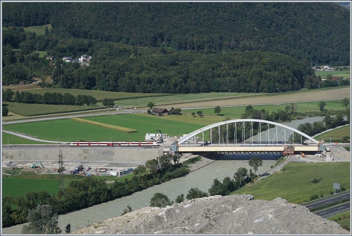 Die Suche nach einem besseren Fotostelle fr die neue Rhonebrcke fhrten mich an Nahe an den sicheren Abgrund. Doch Abschrankungen des Kieswerkes beachtend und so auf ffentlichem Grund bleibend, hat man einen ungefhrlichen und schnen Blick auf die neuen Rhonebrcke, die demnchst an ihren definitiven Standort verschoben werden wird. Auf dem Bild verlsst rt ein  Walliser Domino  die Brcke, welcher fr die seit Fahrplanwechsel teilweise fehlenden Halte der IR als RE zwischen St-Maurice und Aigle verkehrt.
26. August 2016