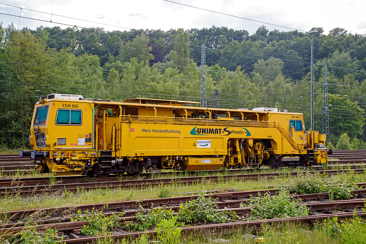 
Die Universal-Stopfmaschine Unimat-Sprinter ESM 866 der DB Netz AG (Schweres Nebenfahrzeug Nr. 97 43 52 006 17-1) steht am 04.06.2016 im Betzdorf/Sieg im Abstellbereich. Der Unimat-Sprinter ist eine von Plasser und Theurer entwickelte Stopfmaschine für Gleise, Weichen und Kreuzungen, speziell konzipiert für die rasche und präzise Behebung von Einzelfehlern. Daher auch die Abkürzung ESM = EinzelfehlerStopfMaschine.

Die Stopfmaschine (ESM – 08 – 275 / Sprinter) wurde 2000 von Plasser & Theurer unter der Fabriknummer 1169 gebaut und an die DB Netz AG geliefert.

Die typische Länge eines Einzelfehlers beträgt 9 bis 15 Schwellen, er kann sich in Einzelfällen aber bis zu 100 m weit erstrecken. Die Ursachen liegen nicht im direkten  Zusammenhang  mit  Nivellier-  und  Richtarbeiten oder Zugbelastungen, sondern vielmehr in punktuellen, scharf   abgegrenzten Schwächen im Unterbau, Frostschäden usw.
Da dieser Einzelfehler in einem völlig intakten Abschnitt liegt,  der keiner durchgehenden Behandlung bedarf, ist es viel zu aufwendig, solche Abschnitte zur Gänze zu bearbeiten. Die Behebung eines Einzelfehlers ist aber unumgänglich, da nicht  nur Gründe wie kostspielige Langsamfahrstellen dafür sprechen, sondern auch die Sicherheit des Fahrweges garantiert werden muss.

Der UNIMAT SPRINTER ist eine speziell für die Einzelfehlerbehebung entwickelte Stopfmaschine. Sie ist mit zwei Weichenstopfaggregaten mit jeweils vier Schwenkpickeln zur universellen Bearbeitung von Strecken und Weichen  ausgestattet. Das kombinierte Hebe- und Richtaggregat besteht aus einem Hebehaken, einer Richtrolle und einer Rollhebezange pro Schienenstrang. Für eine schnelle Überstellung zur Baustelle ist die Maschine mit einem hydrodynamischen Antrieb für eine Höchstgeschwindigkeit von 100 km/h ausgelegt. Flankenpflüge, die im Bereich des vorderen Drehgestells montiert sind und eine Kehrbürste am hinteren Ende der Maschine, sorgen nach den Stopfarbeiten für  die Herstellung des geforderten Schotterprofils.

Technische Daten der UNIMAT SPRINTER:
Spurweite: 1.435 mm
Achsanzahl: 4 (in 2 Drehgestellen)
Achsabstand im Drehgestell: 1.520 mm
Drehzapfenabstand: 10.500 mm
Länge über Puffer: 18.140 mm
Eigengewicht: 54t
Anhängelast: 40 t
Höchstgeschwindigkeit: 100 km/h
Zugelassen zur Mitfahrt: 4 Pers.
Kleinster befahrbarer Kurvenradius:  R 90 m      
Zugelassen für Streckenklasse: A und höher