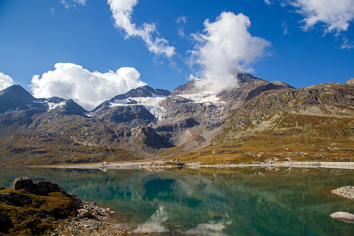Nun erreichen wir am 06.09.2021den Lago Bianco auf einer Höhe von 2.223 Metern über Meer. 

Hier oben bei der Staumauer befindet sich auch zugleich die Wasserscheide zwischen Donau und Po. In Richtung Süden (Tirano) fließ das Wasser in den Po und somit ins Mittelmeer, in Richtung Norden (St. Moritz) fließ das Wasser über den Inn in die Donau und somit ins Schwarze Meer.

Der Lago Bianco ist ein Stausee am Berninapass zwischen dem Valposchiavo und dem obersten Seitental des Engadins, dem Val Bernina, in der Schweiz. Er liegt damit auf der Grenze zwischen den Bernina- (westlich) und Livigno-Alpen (östlich). Früher bestanden im Gebiet des heutigen Stausees zwei natürlichen Seen, der größere Lago Bianco, , und der kleinere südlich anschließende Lago della Scala. In den Lago Bianco mündeten mehrere kleine Bergbäche von den Höhen der Umgebung. Die beiden Gewichtsstaumauern Scala (Südseite) und Arlas (Nordseite) wurden zwischen 1910–1911 errichtet, so dass sich ein Stausee mit einem Volumen von 18,6 Mio. m³ bildete.

Unmittelbar am Nordende des Lago Bianco liegt die kontinentale Wasserscheide zwischen den Einzugsgebieten des Po und des Inn-Donau-Flusssystems. Wenige Meter nördlich des Lago Bianco liegt der Lago Nero (Schwarzsee) am Oberlauf des Berninabaches, dem folgt dann der kleinere Lago Pitschen (Pitschensee).
