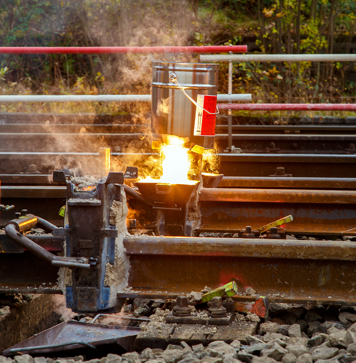 
Thermitschweißen am 31.10.2020 an der Hellertalbahn (KBS 462 / DB-Streckennummer 2651) hier Gleis 1 vom Bahnhof Herdorf.

Bild 5 – Nachdem die Form gefüllt ist, läuft der flüssige Rest (Stahl, Aluminiumoxid und Schlacke) in die seitlichen Schlackenschalen ab.