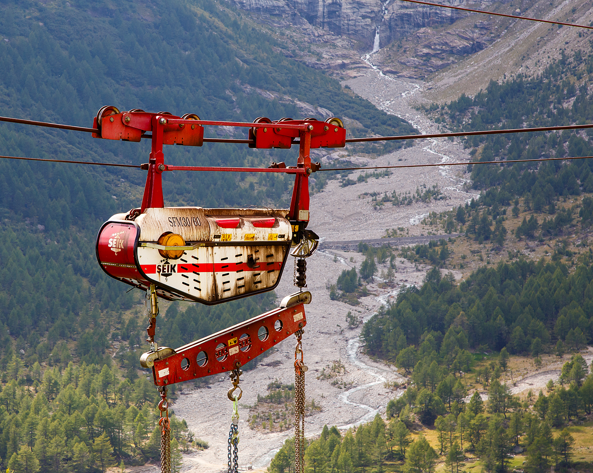 Unterhalb Alp Grüm werden die Alp Grüm der Berninabahn erneuert, daher gibt es eine Materialseilbahn von Alp Grüm hinab zu den Galerien, hier am 06.09.2021. So wird oben in Alp Grüm der Beton gemischt und dann mit der Seilbahn hinab gefahren. 

Die hier verwendete Bahn ist vom italienischen Seilbringungs-Spezialisten Seik (Truden). Der verwendete Wagen ist ein Seilkran vom Typ SFM 30/60.  In dem Seilkran befindet sich ein Verbrennungsmotor der das Hubwerk antreibt (dieser läuft nur bei der Hubbewegen) um wie hier den Betonkübel anzuheben und später wieder abzusenken. Die Hubkraft beträgt im Einzelzug 3t oder wie hier im Doppelzug mit dem Waagbalken 6t. Das Gesamtgewicht beträgt ca. 1t. Die Winde für das Zugseil kann nach Belieben (Bergseite – Talseite) platziert werden.