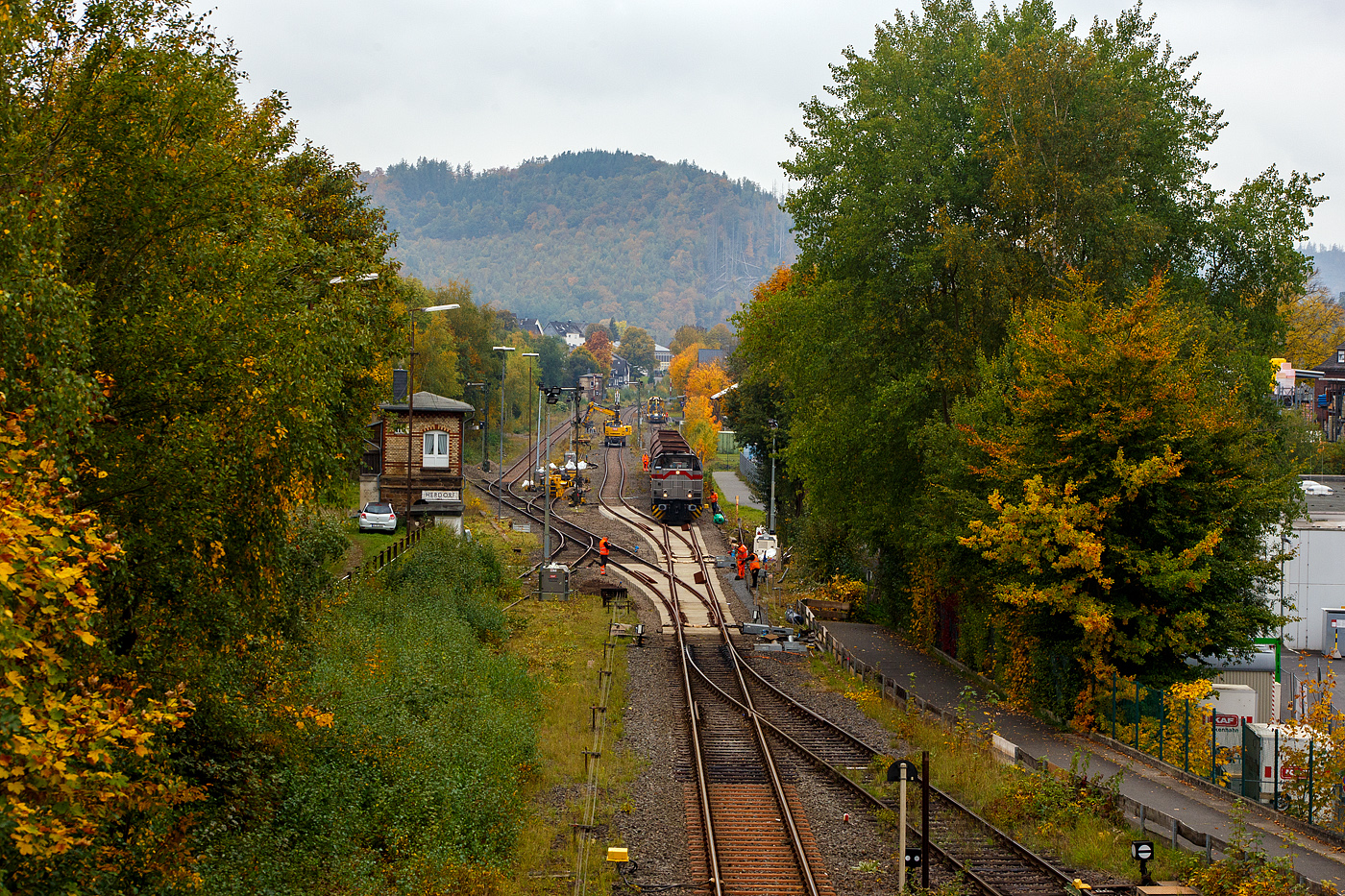 Blick auf den Bahnhof Herdorf und die Baustelle in Blickrichtung Betzdorf am 12 Oktober 2025. Die Weichen 25 und 26 sind beide eingebaut, müssen noch eingeschottert werden.

So steht die 277 809-0  Elmi“ (92 80 1277 809-0 D-KAF), eine Vossloh MaK G 1700 BB der KAF - Falkenhahn Bau AG (Kreuztal), steht mit einem Schotterzug bereit. Hinten beim Bahnhof haben die Schnellschotterplaniermaschine SSP 110 SW, Schweres Nebenfahrzeug Nr. 99 80 9425 068-0 D-DGU und die Universalstopfmaschine UNIMAT 09-475/4S, Schweres Nebenfahrzeug Nr. D-DGU 99 80 9424 001-2, den Bahnhof erreicht müssen aber nach das Einschottern abwarten. Beide Plasser & Theurer Maschinen gehören der Deutsche Gleisbau Union GmbH & Co. KG (DGU), Koblenz

Hier sieht man außerdem gut das Herdorf immer noch den Luxus von 2 Stellwerken besitzt. Vorne links das Weichenwärter Stellwerk Herdorf Ost (Ho) und hinten das Stellwerk Herdorf Fahrdienstleiter (Hf). Beide Stellwerke waren sogar hier bei der Baustelle ganztäglich besetzt.

Ich denke das bei den heutigen Verhältnissen im Bahnhof Herdorf, mit drei aktiven Gleisen und einer Anschlussstelle zum Rangierbahnhof der KSW Kreisbahn Siegen-Wittgenstein (Betriebsstätte FGE - Freien Grunder Eisenbahn) nicht mehr zeitgemäß ist. Es gibt mit Sicherheit heute Möglichkeiten die Aufgaben von einem oder dem anderen Stellwerk fernzusteuern. Früher mit bis zu 30 Gleisen und 3 Anschlussstellen musste es so sein, aber im heutigen Zustand