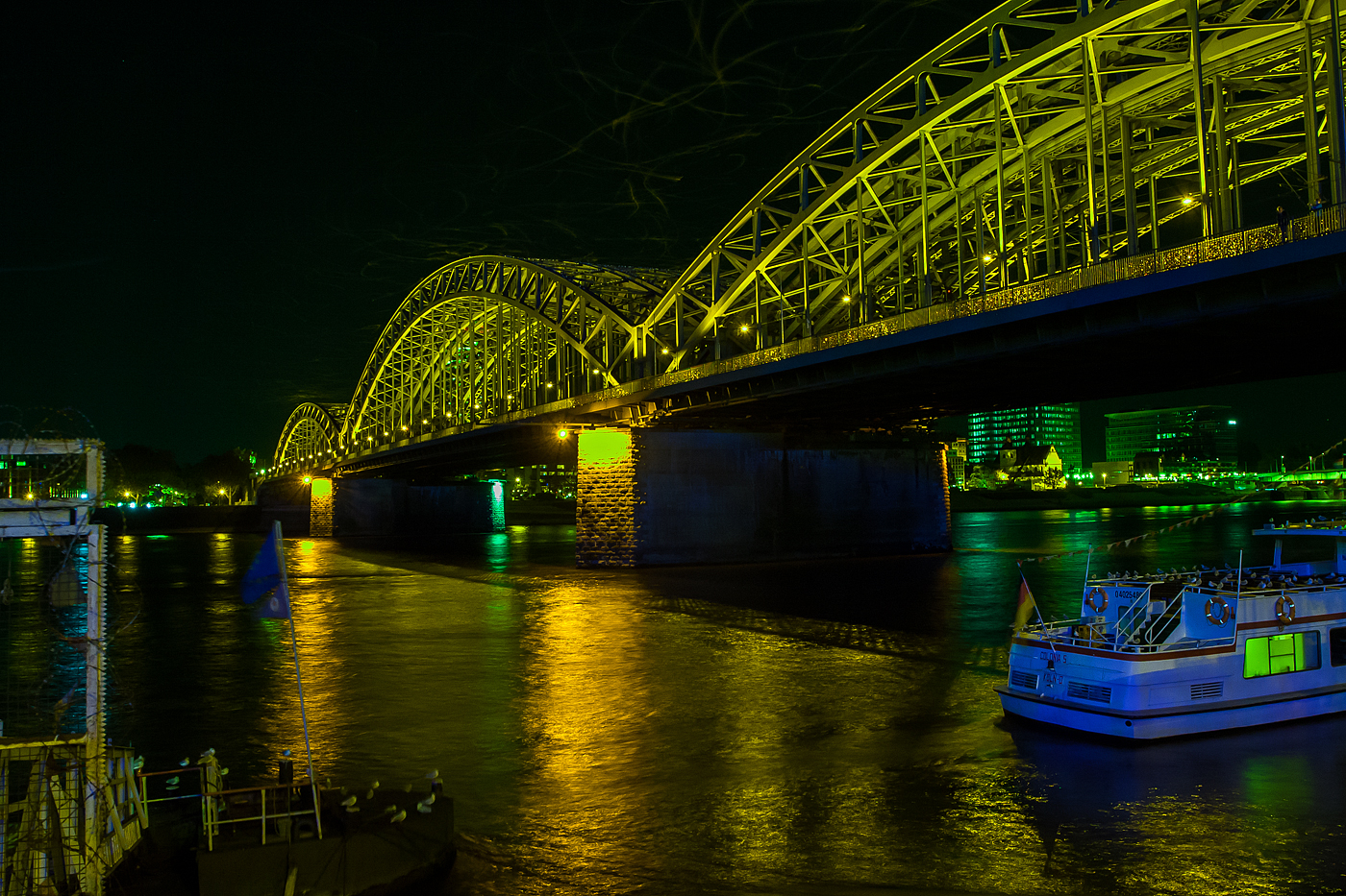 Blick auf die Hohenzollernbrücke in Köln am Abend (20:13 Uhr) des 18 Oktober 2014. Blickrichtung vom linken Rheinufer Rheinaufwärts, auf der anderen Rheinseite liegt Deutz. Mit etwa 1220 Zugfahrten pro Tag ist sie eine der meistbefahrenen Eisenbahnbrücken in Deutschland, nur an diesem Tag sah man bedingt durch einen Streik der GDL kaum einen Zug auf der Brücke.

Die Hohenzollernbrücke wurde von 1907 bis 1911 gebaut. Sie ersetzte die Dombrücke, die den Anforderungen des stetig zunehmenden Eisenbahnverkehrs nicht länger gewachsen war. Das Besondere am Bau der neuen Brücke war, dass sie unter laufendem Betrieb der Dombrücke errichtet wurde und diese nach und nach ersetzte. Sie bestand nach ihrer Fertigstellung aus drei nebeneinander liegenden Fachwerkbogenbrücken mit jeweils drei Bögen.

Die Hohenzollernbrücke ist die einzige Brücke in Köln, die nicht durch Bomben zerstört wurde. Vielmehr übernahm es die Wehrmacht am 6. März 1945 selbst, den herannahenden Alliierten durch Sprengung der Brücke eine Rheinüberquerung zu erschweren. Nach dem Krieg wurde bis 1948 zunächst eine der (zweigleisigen) Bahnbrücken wieder aufgebaut. Die Straßenbrücke wurde aus verkehrstechnischen Gründen nicht wiederhergestellt. In den Jahren 1956 bis 1959 und von 1986 bis 1987 wurde jeweils ein weiterer Fachwerkbogen hinzugefügt, so dass die Bahn heute über sechs Gleise auf der Hohenzollernbrücke verfügt. Die zwei nördlichen Gleise sind der S-Bahn vorbehalten. Bei der Hohenzollernbrücke gibt es zu beiden Seiten Geh- und Radwege, die von der Stadt Köln unterhalten und gepflegt werden, während sich die Brücke selbst, wie auch die Südbrücke, im Eigentum der Deutschen Bahn AG befindet.

Mit etwa 1220 Zugfahrten pro Tag ist sie eine der meistbefahrenen Eisenbahnbrücken in Deutschland.  Das Bauwerk gilt, zusammen mit dem Kölner Hauptbahnhof, als zentraler Engpass im Schienenverkehr in der Region Köln.

Technische Daten:
Typ: sechsgleisige Eisenbahnbrücke mit Geh- und Radwegen auf beiden Seiten
Bauart: drei nebeneinander liegende Fachwerkbögenbrücken
Baujahre: je eine Brücke 1946 bis 1948, 1956 bis 1959 und 1986 bis 1987
Spannweiten: 111,88 Meter - 167,75 Meter - 122,56 Meter, insgesamt 409,19 Meter
Gesamtbreite: 26,20 Meter
