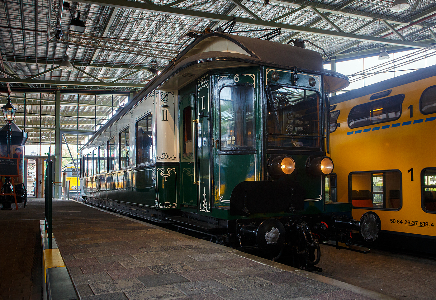 Der älteste elektrische Triebwagen der Niederlande, der ZHESM 6 mBC der Zuid-Hollandsche Electrische Spoorweg-Maatschappij (Südholländischen Elektrischen Eisenbahn-Gesellschaft), später NS BC 9911, am 24 Juni 2025 im Het Spoorwegmuseum (bis 2005 NSM - Nederlands Spoorwegmuseum / Niederländischen Eisenbahnmuseum) in Utrecht im ehemaligen Bahnhof Maliebaan.  

Der Triebwagen wurde 1908 von der Koninklijke Fabriek van Rijtuigen en Spoorwagens J.J. Beijnes (Königliche Fabrik für Kutschen und Eisenbahnwagons J.J. Beijnes) in Haarlem gebaut und bei der Südholländischen Elektrischen Eisenbahn-Gesellschaft mit der Nummer 6 (Serie 1 – 1) in Dienst gestellt. Die ursprüngliche elektrische Ausrüstung war von Siemens Schuckert (Berlin), die aber 1927 von Heemaf (Hengelo) ersetzt wurde.

Die Triebwagen basierten auf einem amerikanischen Design. Sie waren in Creme (oben) und Grün (unten) lackiert und mit einem Jugendstildekor versehen. Es gab 24 Sitzplätze (Samtpolstersitze) der 2. Klasse und 49 (Holzbänke) der 3. Klasse. Die Triebwagen wurden mit einer Anlage für 10 kV Einphasenwechselstrom in Dienst gestellt. In einem Drehgestell waren die beiden Fahrmotoren untergebracht, das andere Drehgestell enthielt den Luftkompressor, der unter anderem für die Bremse zuständig war. Die mBCs bedienten den Nahverkehr Rotterdam Hofplein – Den Haag HS – Scheveningen in der Regel als Zwei-Wagen-Zug.

Im Jahr 1921 ging das Rollmaterial in die neue NS (Nederlandse Spoorwegen) über. Die Nummer 6 wurde mehrfach umgebaut und um nummeriert. Im Jahr 1926 wurden die 23 ZHE-Triebwagen und 17 Mittelwagen auf 1500 Volt Gleichstrom umgerüstet. Der 6er erhielt versuchsweise eine Neuinstallation von Siemens und erhielt wieder das ursprüngliche Zweiklassensystem. 

Der Versuch wurde 1927 beendet, danach wurde der ET erneut mit einer anderen Installation, diesmal von Heemaf, ausgestattet. Außerdem erhielt er nun 4 Motore á 165 KW (225 PS), nun hatte er die Achsfolge Bo´Bo´ (anstatt Bo´2´), so wurde die Leistung erheblich gesteigert. Zudem erhielt er nun die Bezeichnung BC 9011, entsprechend der restlichen Serie BC 9001–9010.

Im Jahr 1930 wurde die mechanische Kilometererfassung eingeführt, die es erforderlich machte, allen Triebfahrzeugen eine eigene Nummernserie zuzuordnen. Für unsere ZHE-ler wurde dies zu BC 9901 – 9911. BC 9011 wurde jetzt zu BC 9911. Die Farbe wurde in den 1930er Jahren durch ein komplett grünes Farbschema ersetzt.

Im Jahr 1944 wurde BC 9911 mit den meisten anderen ZHE-Rollmaterial nach Deutschland gebracht. Nach der Befreiung kehrten die meisten von ihnen in die Niederlande zurück, aber 4 Triebwagen und 1 Waggon der ehem. ZHE blieben vermisst. Die verbliebene und zurückgegebene Ausrüstung hatte erheblichen Schaden genommen. Nur der BC 9911 (ex Nummer 6) war 1946 noch einsatzfähig. Einige kaputte Fenster wurden notdürftig mit Holz und kleinen Glasscheiben verschlossen. Zusammen mit dem Steuerwagen C 8043 bildete er den einzigen ZHE-Zug, der auf der Hofplein-Linie verkehrte.

Ab 1947 wurden auf der Hofplein-Linie nur noch Stromlinienfahrzeuge eingesetzt. Der BC 9911 wurde zum Dienstfahrzeug und transportierte Waggons mit Lagergütern zwischen der Zentralwerkstatt in Haarlem und dem Lijnwerkplaats Leidschendam, blieb jedoch unverändert. Erst später im Jahr 1949 erhielt der Wagen die Dienstnummer 157991.

1957 wurde der technisch vollständige Wagen dem Eisenbahnmuseum gespendet. 1994 fand in der Hauptwerkstatt in Haarlem eine umfangreiche Restaurierung statt, bei der auch das Fahrgestell nach einem früheren Unfall repariert wurde. Dabei musste die elektrische Verkabelung entfernt werden. Nach der Restaurierung wurden die ursprünglichen Farben und Jugendstildekorationen wiederhergestellt. Da der Wagen nicht mehr aus eigener Kraft fahren durfte und nur mit begrenzter Geschwindigkeit transportiert werden konnte, wurde das Antriebssystem nicht repariert. Allerdings sind noch alle elektrischen Komponenten aus dem Jahr 1926 vorhanden.

Der Triebwagen gilt als eines der Highlights des Eisenbahnmuseums.

TECHNISCHE DATEN:
Spurweite: 1.435 mm (Normalspur)
Länge über die Puffer:	18.600 mm
Achsfolge:	Bo'Bo, ursprünglich Bo'2' (1908 bis1927)
Höchstgeschwindigkeit: 80 km/h
Antriebmotoren: 4, ursprünglich 2
Leistung von 1908 bis 1927: 2 x 132 kW (2 x 180 PS)  
Leistung ab 1927: 4 x 165 KW (4 x 225 PS)
Stromsystem: 1.500 V DC, ursprünglich 10 k V 25 Hz Einphasenwechselstrom
Eigengewicht: 62 t
Sitzplätze: 24 der 2. Klasse (Samtpolstersitze) und 49 der 3. Klasse (Holzbänke)
