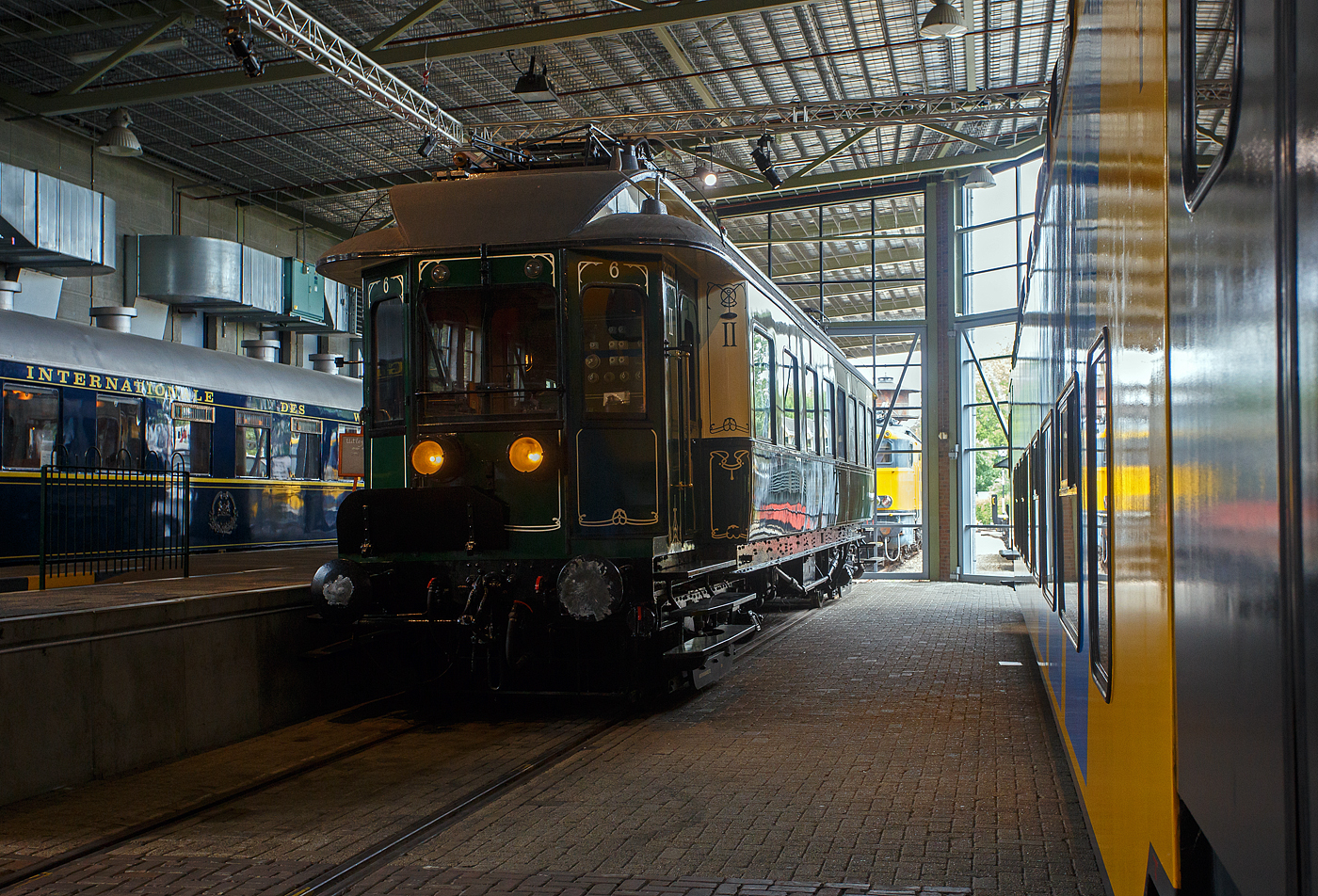 Der �lteste elektrische Triebwagen der Niederlande, der ZHESM 6 mBC der Zuid-Hollandsche Electrische Spoorweg-Maatschappij (S�dholl�ndischen Elektrischen Eisenbahn-Gesellschaft), sp�ter NS BC 9911, am 24 Juni 2025 im Het Spoorwegmuseum (bis 2005 NSM - Nederlands Spoorwegmuseum / Niederl�ndischen Eisenbahnmuseum) in Utrecht im ehemaligen Bahnhof Maliebaan.  

Der Triebwagen wurde 1908 von der Koninklijke Fabriek van Rijtuigen en Spoorwagens J.J. Beijnes (K�nigliche Fabrik f�r Kutschen und Eisenbahnwagons J.J. Beijnes) in Haarlem gebaut und bei der S�dholl�ndischen Elektrischen Eisenbahn-Gesellschaft mit der Nummer 6 (Serie 1 – 1) in Dienst gestellt. Die urspr�ngliche elektrische Ausr�stung war von Siemens Schuckert (Berlin), die aber 1927 von Heemaf (Hengelo) ersetzt wurde.

Die Triebwagen basierten auf einem amerikanischen Design. Sie waren in Creme (oben) und Gr�n (unten) lackiert und mit einem Jugendstildekor versehen. Es gab 24 Sitzpl�tze (Samtpolstersitze) der 2. Klasse und 49 (Holzb�nke) der 3. Klasse. Die Triebwagen wurden mit einer Anlage f�r 10 kV Einphasenwechselstrom in Dienst gestellt. In einem Drehgestell waren die beiden Fahrmotoren untergebracht, das andere Drehgestell enthielt den Luftkompressor, der unter anderem f�r die Bremse zust�ndig war. Die mBCs bedienten den Nahverkehr Rotterdam Hofplein – Den Haag HS – Scheveningen in der Regel als Zwei-Wagen-Zug.

Im Jahr 1921 ging das Rollmaterial in die neue NS (Nederlandse Spoorwegen) �ber. Die Nummer 6 wurde mehrfach umgebaut und um nummeriert. Im Jahr 1926 wurden die 23 ZHE-Triebwagen und 17 Mittelwagen auf 1500 Volt Gleichstrom umger�stet. Der 6er erhielt versuchsweise eine Neuinstallation von Siemens und erhielt wieder das urspr�ngliche Zweiklassensystem. 

Der Versuch wurde 1927 beendet, danach wurde der ET erneut mit einer anderen Installation, diesmal von Heemaf, ausgestattet. Au�erdem erhielt er nun 4 Motore � 165 KW (225 PS), nun hatte er die Achsfolge Bo´Bo´ (anstatt Bo´2´), so wurde die Leistung erheblich gesteigert. Zudem erhielt er nun die Bezeichnung BC 9011, entsprechend der restlichen Serie BC 9001–9010.

Im Jahr 1930 wurde die mechanische Kilometererfassung eingef�hrt, die es erforderlich machte, allen Triebfahrzeugen eine eigene Nummernserie zuzuordnen. F�r unsere ZHE-ler wurde dies zu BC 9901 – 9911. BC 9011 wurde jetzt zu BC 9911. Die Farbe wurde in den 1930er Jahren durch ein komplett gr�nes Farbschema ersetzt.

Im Jahr 1944 wurde BC 9911 mit den meisten anderen ZHE-Rollmaterial nach Deutschland gebracht. Nach der Befreiung kehrten die meisten von ihnen in die Niederlande zur�ck, aber 4 Triebwagen und 1 Waggon der ehem. ZHE blieben vermisst. Die verbliebene und zur�ckgegebene Ausr�stung hatte erheblichen Schaden genommen. Nur der BC 9911 (ex Nummer 6) war 1946 noch einsatzf�hig. Einige kaputte Fenster wurden notd�rftig mit Holz und kleinen Glasscheiben verschlossen. Zusammen mit dem Steuerwagen C 8043 bildete er den einzigen ZHE-Zug, der auf der Hofplein-Linie verkehrte.

Ab 1947 wurden auf der Hofplein-Linie nur noch Stromlinienfahrzeuge eingesetzt. Der BC 9911 wurde zum Dienstfahrzeug und transportierte Waggons mit Lagerg�tern zwischen der Zentralwerkstatt in Haarlem und dem Lijnwerkplaats Leidschendam, blieb jedoch unver�ndert. Erst sp�ter im Jahr 1949 erhielt der Wagen die Dienstnummer 157991.

1957 wurde der technisch vollst�ndige Wagen dem Eisenbahnmuseum gespendet. 1994 fand in der Hauptwerkstatt in Haarlem eine umfangreiche Restaurierung statt, bei der auch das Fahrgestell nach einem fr�heren Unfall repariert wurde. Dabei musste die elektrische Verkabelung entfernt werden. Nach der Restaurierung wurden die urspr�nglichen Farben und Jugendstildekorationen wiederhergestellt. Da der Wagen nicht mehr aus eigener Kraft fahren durfte und nur mit begrenzter Geschwindigkeit transportiert werden konnte, wurde das Antriebssystem nicht repariert. Allerdings sind noch alle elektrischen Komponenten aus dem Jahr 1926 vorhanden.

Der Triebwagen gilt als eines der Highlights des Eisenbahnmuseums.

TECHNISCHE DATEN:
Spurweite: 1.435 mm (Normalspur)
L�nge �ber die Puffer:	18.600 mm
Achsfolge:	Bo'Bo, urspr�nglich Bo'2' (1908 bis1927)
H�chstgeschwindigkeit: 80 km/h
Antriebmotoren: 4, urspr�nglich 2
Leistung von 1908 bis 1927: 2 x 132 kW (2 x 180 PS)  
Leistung ab 1927: 4 x 165 KW (4 x 225 PS)
Stromsystem: 1.500 V DC, urspr�nglich 10 k V 25 Hz Einphasenwechselstrom
Eigengewicht: 62 t
Sitzpl�tze: 24 der 2. Klasse (Samtpolstersitze) und 49 der 3. Klasse (Holzb�nke)
