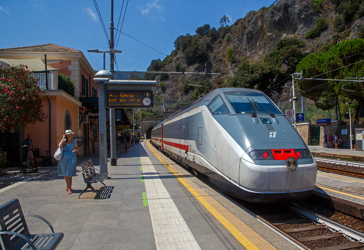 Der Bahnhof Monterosso Cinque Terre (komplette Bezeichnung der Gemeide Monterosso al Mare) an der Italienischen Riviera. Von den den Cinque Terre Bahnhfen hat Monterosso die lngsten Bahnsteige unter freiem Himmel, so halten hier auch Intercity-Zge. 

Das Fischerdorf Monterosso al Mare ist das nrdlichste Dorf und mit rund 1700 Einwohnern der grte Ort der Cinque Terre an der Italienischen Riviera. Monterosso erstreckt sich ber rund 1,5 Kilometer und ist zweigeteilt, die kleine Altstadt ist vom neueren Viertel Fegina durch einen ins Meer ragenden Felsen getrennt, auf dem sich der markante Wachtturm Torre Aurora aus dem 16. Jahrhundert erhebt. Durch den Felsen fhrt ein rund 100 m langer Fugngertunnel.

Hier verlsst am 22.07.2022 gerade, im Sandwich zweier E.414 (ehemalige Triebkpfe E.404 A der ersten ETR 500 – Monotensione), der Trenitalia InterCity IC 670 (Livorno – Pisa - La Spezia - Monterosso - Genova - Milano Centrale), den Cinque Terre Bahnhof Monterosso.