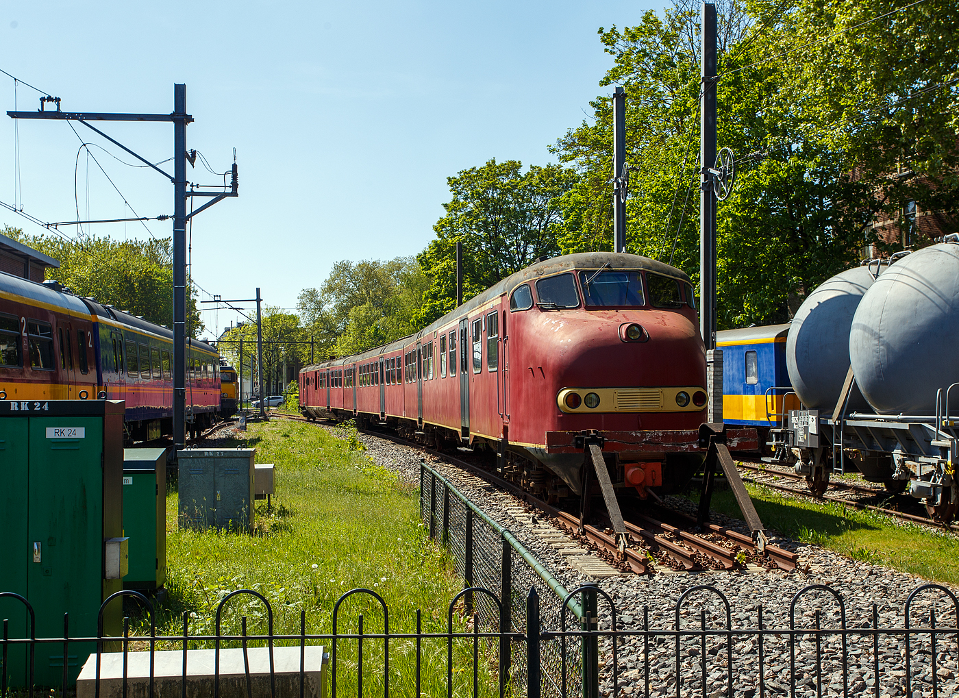 Der dreiteilige Dieseltriebzug NS 114, vom NS-Typ DE 3 – Plan U „Rode Duivel“ (Roter Teufel), am 29 April 2025 im Het Spoorwegmuseum (bis 2005 NSM - Nederlands Spoorwegmuseum / Niederländischen Eisenbahnmuseum) in Utrecht im Bahnhof Maliebaanstation. Ein sehr schönes Eisenbahnmuseum das zum Verweilen einlädt, leider fehlte uns dieses Mal die Zeit dafür. 

Der dieselelektrische Triebzug wurde 1960 von Werkspoor N.V. in Utrecht (NL) für die NS - Nederlandse Spoorwegen (Niederländische Staatsbahnen) gebaut und geliefert. 

Ab 1960 wurden gemäß dem Investitionsplan U der NS 42 dieselelektrische Triebzüge der Serie 111 bis 152 in Betrieb genommen, die die älteren dreiteiligen Dieseleinheiten (Mat'34 – DE3) aus dem Jahr 1934 ersetzten. Die Farbe war ursprünglich Tomatenrot, daher auch ihr Spitzname „Rode Duivel“ (Roter Teufel), auch wenn später ab 1968 „gelb“ wurden, Die Kopfform mit Nase und hoher Kabine wurde von der Materieel '54 abgeleitet. Je nach Verkehrsangebot konnten bis zu drei DE3-Triebzüge mit den automatischen Scharfenberg-Kupplungen kombiniert werden. Das Erscheinen des DE3 diente auch als Vorbild für den späteren Materieel ’64 und die Motorpostwagen der Baureihen 3001 – 3035. Die Dieselzüge waren für den Einsatz auf den nicht elektrifizierten Hauptstrecken wie Geldermalsen – Dordrecht, Zwolle – Emmen, Nijmegen – Venlo – Roermond und anderen Strecken vorgesehen. 

Die Züge haben eine Länge von 74,4 m, eine Breite von 2,78 m und wiegen 136 Tonnen. Die Zuggarnituren bestehen aus drei Wagenkästen. Die Züge ruhen auf sechs Drehgestellen, so ist die Achsfolge ist Bo'Bo' + 2'2' + 2'2'. In einem der Endwagen (mBDk) ist der Motorraum, so war dieser nur Hälfte für Passagiere zugänglich. Diese Endwagen hat zudem einen Gepäckraum von 9 m² und einer Tragkraft von 1.500 kg. Dieser Gepäckraum ist von außen über eine Schiebetür und vom Passagierraum zugänglich. Ein Zug verfügt über 202 Sitzplätze, aufgeteilt in 24 Plätze der ersten Klasse, 168 Plätze der zweiten Klasse und 10 Klappsitze.

Die dreiteiligen Dieseltriebzügen waren mit einem 16-Zylinder-Viertakt-V- Dieselmotor mit Büchi-Hochdruckaufladung und Ladeluftkühlung des Typs Werkspoor RUHB 1616 ausgestattet. Der Motor mit einer Ricardo-Wirbelkammereinspritzung ausgerüstet. Der Motorhubraum betrug 64,339 Liter (4,021 Litern je Zylinder, Bohrung Ø 160 mm x 200 mm Hub). Die Motorleistung betrug 1.000 PS (736 kW) bei 1.400 U/min, die Leerlaufdrehzahl lag bei 800 U/min. Dieser Dieselmotor trieb einen direkt gekuppeltem Hauptgenerator vom Typ Heemaf GMT 1040 an. Dieser Generator liefert eine Leistung von 625 kW bei einer Spannung von 700 Volt. Der erzeugte Strom treibt die 4 Vickers AEI-Traktionsmotoren vom Typ MV 139, oder Heemaf Typ GT 38-22 (mit gleichen Spezifikationen), an. Jeder E-Motor hat eine Leistung von 147 kW (PS) bei 700 Volt. Der Zug verfügt so über eine Gesamttraktionsleistung von 588 kW am Rad. Die Aufhängung dieser Motoren entspricht der Aufhängung einer Straßenbahn. Der Fahrmotor ruht auf einer Seite auf einem Stahlgussrohr, welches mit zwei Kegellagern auf der Achse gelagert ist. Das Motorgehäuse wird mit zwei Deckeln auf das Stahlgussrohr gummigelagert geklemmt. Der Antrieb der Motorwelle erfolgt über ein Ritzel, das ein Zahnrad auf der 
Radwelle antreibt. Das Übersetzungsverhältnis beträgt 17:65. Der Zug ist für eine Geschwindigkeit von 140 km/h ausgelegt, im Planbetrieb wurde eine Geschwindigkeit von 125 km/h gefahren. Zur Stromversorgung des Steuerstroms und der Beleuchtung sind am Hauptgenerator ein Generator und ein Hilfsgenerator der Firma Heemaf, Typ GMT 370/20, installiert. Der Antrieb erfolgt mittels Keilriemen. Mit einer Leistung von 30 kW liefert der Hilfsgenerator 145 Volt für Wechselrichter, Steuerstrom und Kabinenheizung. 

Der Triebzug ist mit einem Kraftstofftank mit einem Fassungsvermögen von 1.675 Litern ausgestattet. 

Ab 1968 wurden die Züge in der neuen NS Hausfarbe Gelb lackiert. Ab 1972 wurden die Schiebetüren durch die inzwischen von Mat ’64 eingeführten und erfolgreich erprobten Pendeltüren ersetzt. Lediglich die Schiebetür im Gepäckraum blieb erhalten.

1980 begann man damit die Werkspoor Dieselmotore gegen einen V-12-Zylinder-Viertakt-Dieselmotor mit Abgasturboaufladung und Ladeluftkühlung vom Typ MGO-175 BSHR vom französischer Hersteller SACM (Société Alsacienne de Constructions Mécaniques mit Sitz in Mulhouse, Elsass). Der Motorhubraum betrug nun 53,7 Liter (Bohrung Ø 180 mm x 175 mm Hub). Die Motorleistung betrug nun 1.430 PS (1.050 kW) bei 1.500 U/min. Dieser Austausch wurde notwendig, da Werkspoor 1977 die Herstellung von Teilen für den RUHB-Dieselmotor einstellt. Die Ersatzteilversorgung wurde bereits 1976 problematisch. Um genügend Motoren zur Verfügung zu haben, wurde ein neuer Lieferant gesucht und die Motoren von SACM. Neben dem Austausch des Dieselmotors wurde auch das Kühlsystem modifiziert. Durch den Motorentausch konnten 15 % Kraftstoff gespart werden und die neuen Motoren machten weniger Lärm.

TECHNISCHE DATEN:
Serie: NS DE 3 – Plan U „Rode Duivel“ (Roter Teufel)
Gebaute Anzahl: 42
Nummerierung: 111-152 (191-195)
Typ: dieselelektrischer Triebzug
Baujahre: 1960-1963
Ausmusterung: 2003
Hersteller: Werkspoor N.V. in Utrecht
Spurweite: 1.435 mm (Normalspur)
Achsfolge: Bo'Bo' + 2'2' + 2'2' (12 Achsen in 6 Drehgestellen)
Zusammensetzung: mBDk + B + ABk
Länge über Kupplung: 74.430 mm
Breite: 2.780 mm
Höhe: 3.770 mm
Treib- und Laufraddurchmesser: 950 mm (neu) 
Dieselmotor: 16-Zylinder Werkspoor RUHB 1616, ab 1980 12-Zylinder 
SACM MGO-175 BSHR (Beschreibungen s.o.)
Motorleistung: 736 kW (1.000 PS)
Übersetzung: 17:65
E-Antriebsmotoren: 4 Stück Vickers Typ MV 139 oder Typ GT 38-22 
E-Motordauerleistung: 4 x 147 kW = 588 kW
Höchstgeschwindigkeit: 125 km/h (Planmäßig) / 140 km/h (Konstruktiv)
Eigengewicht: 136 t 
Anzahl der Doppeltüren je Seite: 6
Sitzplätze (gesamt): 202
Sitzplätze in der 1. Klasse: 24
Sitzplätze in der 2. Klasse: 168
Anzahl der Klappsitze: 10
Gepäckraum: 9 m² mit 1.500 kg Nutzlast
Tankvolumen: 1675 Liter
Kupplung: Scharfenberg

