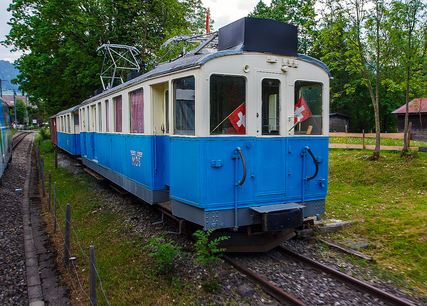 Der ehemalige MOB Triebwagen De 4/4 26 mit dem Personenwagen B⁴ 61 am 28 Mai 2012 in Saanen, aufgenommen aus fahrendem Zug. Der Zug ist seit 1994  abgestellt als Vereinslokal der Modellbahngruppe Obersimmental-Saanenland (MOS). 

Der Triebwagen wurde 1912 von SIG (Schweizerische Industriegesellschaft) in Neuhausen am Rheinfall, mit der elektrischen Ausrüstung von Alioth (Elektrizitätsgesellschaft Alioth - EGA) gebaut und als elektrischer Triebwagen mit 2.Klasse-, Gepäck- und Postabteil BFZe 4/4 26 an die MOB (Montreux-Berner Oberland-Bahn) geliefert.Mit der Abschaffung der 3. Klasse erfolgte 1956 Umbezeichnung zum AFZe 4/4 26, 1962 wurde zum ADZe 4/4 26 und 1971 zum BDe 4/4 26 (Postabteil entfiel). Bereits ab 1972 ging er zum Bahndienst, die Bänke und Gepäckträger im Abteil wurden entfernt, die Umzeichnung in De 4/4 26 erfolgte aber erst 1991 und 1994 wurde er dann an die Modellbaugruppe Obersimmental – Saanenland verkauft.

Geschichte:
Für die 1910 eingeführten Schnellzüge zwischen Montreux und Zweisimmen braucht die MOB ein geeignetes Fahrzeug, da man mit den BCFe 4/4 7–20 oft in Doppeltraktion fahren mussten. Aus diesem Grund bestellte sie diese vier Triebwagen. Weil sie nur im hochwertigen Verkehr eingesetzt werden sollten, besaßen sie nur ein 2. Klassenabteil. Dazu kam noch ein Gepäck- und ein Postabteil. Nach der Zusammenlegung der 1. und 2. Klasse im Jahr 1956, wurde das 2. Klassenabteil zum 1. Klassenabteil, und somit zum AFZe 4/4. Erst 1968/71 wurde dieses deklassiert und in ein 2. Klassenabteil umgewandelt, zugleich wurde auch das Postabteil aufgehoben, die neue Bezeichnung lautet BDe 4/4. 1979 kam es bei den letzten Triebwagen Nummer 25 und 26 zur Aufhebung des Personenabteils und die Fahrzeuge verkehrten als De 4/4. Der Triebwagen Nummer 24 wurde schon 1970 in den Xe 4/4 24 umgebaut. Der Triebwagen Nummer 25, wurde 1988 abgebrochen. Der Triebwagen Nummer 26 1994 der Modellbahngruppe Obersimmental-Saanenland übergeben, welche ihn beim Bahnhof Sannen als Vereinslokal aufstellte.

Technisches:
Die Fahrzeuge haben einen verblechten Holzkasten, der auf einem genieteten Stahlrahmen ruht. Die Kraftübertragung erfolgt über einen geschlossenen Tatzlager-Antrieb mit zweiteiligen elastischen Zahnrädern. Der Gleichstrom-Motor ist vierpolig ausgeführt und ist eigen-ventiliert. Die Übersetzung betrug bei Ablieferung 1:6,29. Bei 700 Volt an der Motorenklemme entwickelte die Motoren an der Welle eine Stundenleistung von 456 PS (336 kW). Die Steuerung der Motoren erfolgt direkt über die Fahrschalter. Auch liegt an den Motorenklemmen je nach Fahrstufe die volle Fahrleitungsspannung an. Sie besitzen zehn Fahr- und fünf Bremsstufen. Es war von Anfang an eine elektrische Widerstandsbremse eingebaut. Als Triebwagen und Zugbremse ist es eine Vakuum-Bremse der Bauart Hardy eingebaut, die auf alle vier Räder wirkt. Zusätzlich ist als Hand- bzw. Feststellbremse auf jedem Führerstand eine Handspindelbremse vorhanden. Die Fahrzeugbedienung erfolgt stehend. Die Höchstgeschwindigkeit betrug, bei der MOB erstmals ab Werk, 50 km/h. Jedes der 900 mm messende Triebrad hat einen eigenen Motor.

Das 2. Klassenabteil hatte 12 Sitzplätze, im Gepäckraum waren 9 Notsitze vorhanden, die beim Bedarf der 3. Klasse zugewiesen waren. Das Gepäckabteil war 7 m² groß und das Postabteil 6 m². Der Zugang zum Personenabteil erfolgt über eine geschlossene Plattform direkt hinter dem Führerstand und ist als Großraumabteil angelegt. Der Zugang zum andern Führerstand erfolgt über eine nur einseitig zugängliche Plattform hinter dem Führerstand. Beide Führerstände besaßen eine Stirnwandtüre. Das Post- und Gepäckabteil besaß auf beiden Längsseiten je eine innen liegende Schiebetüre. Zwischen Personen- und Gepäckabteil war eine Toilette eingebaut.

Umbauten:
Im Jahr 1926 wurden alle Fahrzeuge mit einer Sicherheitssteuerung für den Einmannbetrieb ausgerüstet. Um 1943/44 wurden beide Lyrabügel durch Scherenstromabnehmer ersetzt. Zugleich Neubemalung in blau-crème anstelle des ursprünglichen perlgrau-crème.

TECHNISCHE DATEN:
Hersteller: SIG / Alioth
Spurweite: 1.000 mm (Schmalspur)
Achsformel: Bo’Bo’
Länge über Puffer: 14.500 mm
Länge des Kastens: 13.500 mm
Drehzapfenabstand: 10.700 mm
Achsabstand im Drehgestell: 2.200 mm
Triebraddurchmesser: 900 mm (neu)
Höhe: 3.700 mm
Breite: 2.700 mm
Stundenleistung: 336 kW (456 PS)
Stundenzugkraft : 6,35 t (bei 18 km/h)
Übersetzung: 1:6,28
Höchstgeschwindigkeit: 50 km/h
Eigengewicht: 33,5  t
Fahrleitungsspannung: 850 V DC (Gleichstrom), ursprünglich 750 V DC
Stromabnehmer: 2 Scherenstromabnehmer
Sitzplätze: 12  (und 9 Notsitze im Gepäckraum) 
Gepäck- Postraumfläche: 7 m² / 6 m²
Bremsen: Hs / V / C / X
Kupplungen: Mittelpuffer mit einer Schraubenkupplungen (Zp 1)

Quellen: x-rail.ch, de.wikipedia.org
