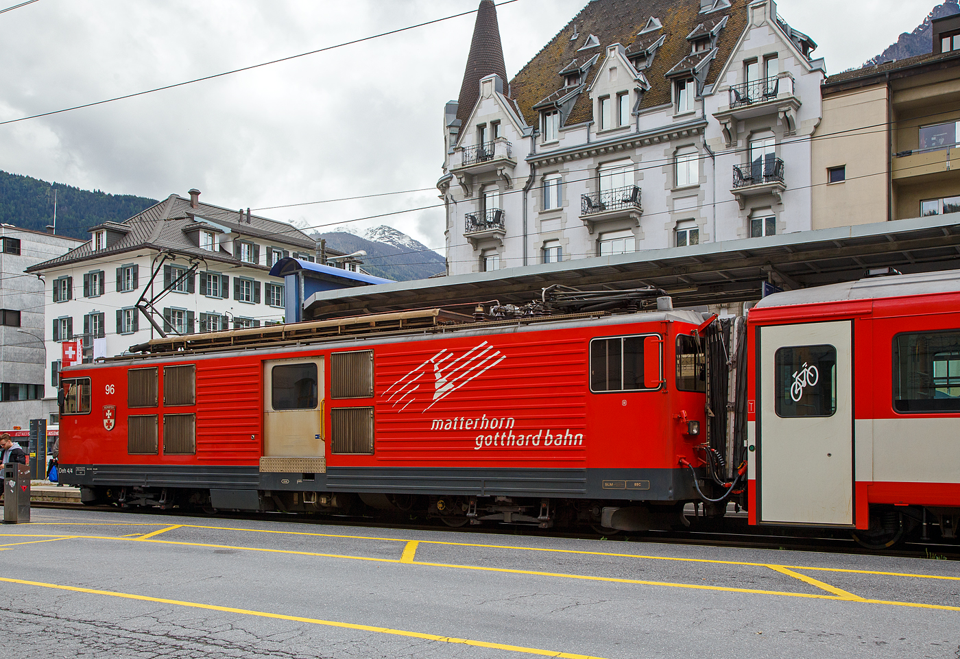 Der Gepäcktriebwagen Deh 4/4 II - 96  Münster   der Matterhorn-Gotthard-Bahn (MGB), ex FO 96  Münster   (Furka-Oberalp-Bahn), am 25.05.2023 mit einen Regionalzug von Andermatt nach Visp im Bahnhof (Vorplatz) Brig.

Der Elektrischer Zahnradtriebwagen wurde 1984 von SLM (mechanischer Teil, Lokomotivkasten) und BBC (elektrische Ausrüstung) gebaut.

Die vier 1980 bei der Furka- Oberalp-Bahn in Betrieb genommenen Gepäcktriebwagen sind für Adhäsions- und Zahnstangenstrecken konzipiert. Zwei weitere Einheiten wurden 1982 in Auftrag gegeben. Sie werden auf dem ganzen Streckennetz – maximale Steigung 179%o - als Triebfahrzeuge für Züge mit vier bis fünf Wagen eingesetzt. Der biege- und verwindungssteife, extrem leichte Kasten wurde in Stahl ausgeführt und die hohe Steifigkeit durch Strukturgebung erzielt. Dem leichten Innenausbau und der ergonomischen Führerstandgestaltung wurde ebenfalls besondere Aufmerksamkeit geschenkt.

Die Drehgestelle, die durch tiefliegende Drehzapfen über Traversen  mit dem Kasten verbunden sind, enthalten je zwei Antriebsmotoren. Die Betriebsverhältnisse erfordern drei unabhängige Bremssysteme.

Die ehemaligen Deh 4/4 I und II der FO (Furka-Oberalp-Bahn) werden im Einsatz nicht unterschieden, wenn nötig, dann anhand der Seriennummern 2.., 5.. und 9... Wobei sie sich optisch und technisch schon etwas unterscheiden. Sie werden hauptsächlich zusammen mit zwei Mittelwagen und einem Steuerwagen als fest gekuppelte Pendelzüge eingesetzt. Zwischen Disentis und Andermatt (Oberalp, 110‰) kann ein und zwischen Visp und Andermatt (Goms, 90‰) können zwei, im Sommer drei Verstärkungswagen angehängt werden. Zwischen Andermatt und Göschenen (Schöllenenschlucht, 179‰) sind keine Verstärkungswagen möglich. Die Pendelzüge sind innerhalb der Komposition mit der automatischen +GF+-Kupplung (GFN) verbunden. Für andere Verwendungen müssen die Kupplungen getauscht werden. Mindestens ein Triebwagen, früher waren dies meist Nr. 95 oder 96, dient als Ersatzfahrzeug für die übrigen Deh und wird auch allein für Überfuhren eingesetzt. Früher wurden auch Güterzüge nach Göschenen geführt.

TECHNISCHE DATEN:
Spurweite: 1.000 mm
Achsformel: Bo’Bo’
Länge über Puffer: 15.500 mm
Drehzapfenabstand: 8.800 mm
Achsabstand im Drehgestell: 2.790 mm
Größte Breite: 2.683 mm
Größte Höhe (bei abgesenkten Stromabnehmer): 3.880 mm
Leergewicht: 49,5 t (davon Mechanischer Teil 28 ,5 t)
Dienstgewicht: 51,0 t
Maximale Zuladung: 1,5 t
Gepäckraum Fläche: 10 m²
Höchstgeschwindigkeit: Adhäsion 60 km/h / Zahnstange 30 km/h
Stundenleistung: 1.032 kW
Dauerleistung: 936 kW
Stundenzugkraft am Rad: 117,2 kN
Dauerzugkraft am Rad: 101,2 kN
Maximale Zugkraft am Rad: 247,2 kN
Stromsystem: 11 kV 16,7 Hz AC
Anzahl der Fahrmotoren: 4