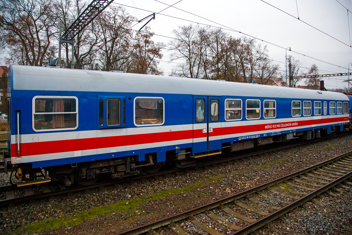 Der Gleismesswagen CZ-SZCZ 99 54 93-62 005-9 der Sprva eleznic (SCZ) steht am 24.11.2022 hinter der Vectron 193 901-6 bei Karltejn (deutsch Karlstein, zum Bezirk Beroun). Aufnahme aus dem Zugheraus.

Das staatliche tschechische Eisenbahninfrastrukturunternehmen hie bis Januar 2020 SDC - Sprva elezničn dopravn cesty (deutsch: Verwaltung der Eisenbahn-Verkehrswege) und wurde Sprva eleznic (SCZ) unbenannt.

Der Gleismesswagen dient zur Messung der geometrischen Parameter der Gleise. Er wurde von der niederlndischen Firma ER aus einem vom VEB Waggonbau Bautzen 1989/90 gebauten ČD-Schnellzugwagen der Gattung Bymee umgebaut. 

Die geometrischen Parameter des Gleises werden berhrungslos alle 0,25 m des abgefahrenen Gleises abgetastet. Die Messgrenergebnisse werden in dynamische und quasistatische Anteile der Gleislage unterteilt. Dynamische Gren reprsentieren Lngshhe, berhhung, Gleisrichtung, Spurweite, Einbruch mit optionaler Basislnge. Quasistatische Gren reprsentieren Krmmung, Hhe und Spurweite. Das System zur Messung einzelner geometrischer Parameter verwendet Beschleunigungssensoren, Winkelgeschwindigkeiten, induktive Wegsensoren, ein laseroptisches System mit CCD-Kameras (zur Spur- und Richtungsmessung). Die Messwerte werden von einem Computer verarbeitet mit einer bersicht ber die unmittelbaren Mngel der Abschnittsauswertung. Individuelle Dateien ermglichen die Weiterverarbeitung im Auswertezentrum. Der Messwagen ist auerdem mit einem Videosystem ausgestattet, das die gemessene Strecke kontinuierlich aufzeichnet.

TECHNISCHE DATEN:
Spurweite: 1.435 mm (Normalspur)
Anzahl der Achsen: 4 
Lnge ber Puffer:  26.400 mm
Drehzapfenabstand: 19.000 mm
Hhe: 4.050 mm
Breite: 3.140 mm
Achsabstand: 8.000 mm
Eigengewicht: 43.245 kg
Hchstgeschwindigkeit: 160 km/h 
Bremse: DK-PR (D)
Kleister befahrbarer Gleisbogen: R = 150 m
