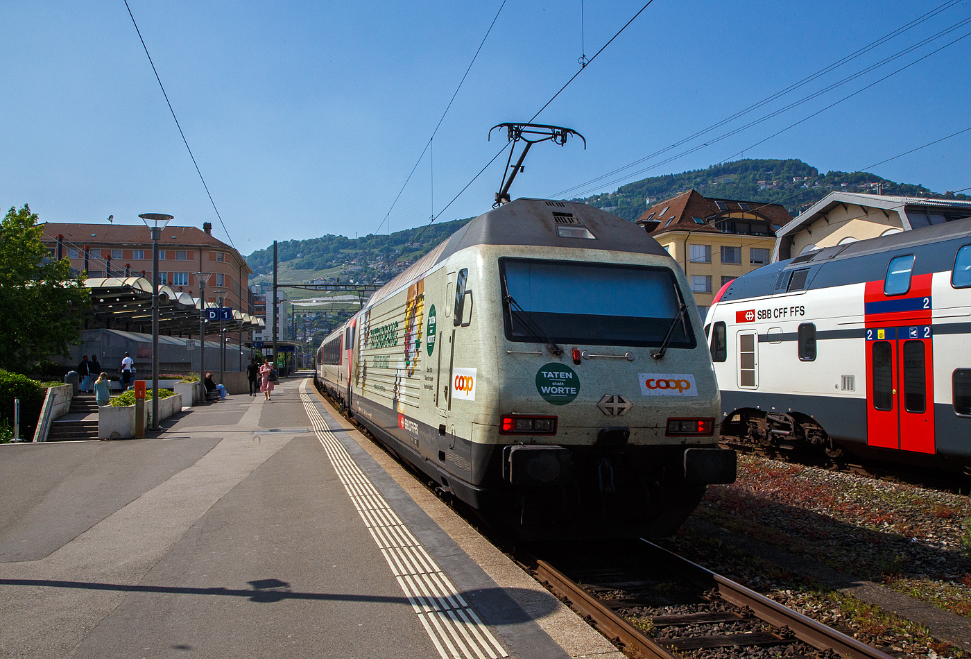 Der IR 90 von Brig nach Genève-Aéroport (Umlauf IR 1724) verlässt am 26 Mai 2023 den Bahnhof Vevey und fährt weiter in Richtung Lausanne bzw. Genf. Da der Zug recht lang war wurde im Sandwich gefahren, geführt von der SBB Re 460 069-8  Verkehrshaus  und hier im Bild am Zugschluss von der Werbe-LOK2000, der SBB Re 460 041-7  Mendrisiotto  (91 85 4 460 041-7 CH-SBB) mit der COOP Werbung.

Die Re 460 041-7 wurde 1993 von der SLM (Schweizerischen Lokomotiv- und Maschinenfabrik in Winterthur) unter der Fabriknummer 5518 gebaut, der elektrische Teil ist von der ABB (Asea Brown Boveri). Im SBB Werk Yverdon-les-Bains erfolgte 2018 die vollständige Modernisierung LOK2000, so soll sie fit für die nächsten 20 Jahre sein.

Seit 2021 trägt die Re 460 041-7 die COOP-Werbung mit der Aufschrift:
TATENDRANG 
BEWEGT DIE SCHWEIZ
TATEN statt WORTE - Über 395 Taten für mehr Nachhaltigkeit.

Modernisierungs-/Refit-Programm der LOK2000 (Re 460):
Zwischen 2015 und November 2022 unterzog die SBB alle ihrer 119 Re 460 Lokomotiven (LOK2000) einem Refit-Programm (Modernisierung) im SBB Werk Yverdon-les-Bains (VD). Dabei wurden unter anderem die auf dem GTO-(Thyristor)-Halbleiter-Technologiestand der 1990er-Jahre basierende Leistungselektronik (GTO- Traktionsumrichter) durch IGBT-Traktionsumrichter (insulated-gate bipolar transistor) der neuesten Generation von ABB ersetzt, welche die Fahrmotoren mit Strom speisen und Bremsenergie zurückgewinnen. Die SBB hat damit, in Zusammenarbeit mit der ABB, die gesamte Flotte Re 460 modernisiert und hat diese auf den neuesten Stand der Antriebstechnik gebracht. Die gesamte Flotte spart dank neuen Traktionsumrichtern und weiteren technischen Optimierungen jedes Jahr rund 30 Gigawattstunden Energie ein, das sind fünf Gigawattstunden mehr als ursprünglich erwartet. Die Energieeinsparungen entsprechen dem durchschnittlichen Stromverbrauch von 10.000 Schweizer Haushalten. Die Umrüstung auf modernste IGBT-Technologie und mit Wasser statt Öl betriebene Kühlsysteme der Umrichter ermöglicht eine Senkung des Energieverbrauchs und sorgt für einen ökologischeren und sicheren Bahnbetrieb.

Geschichte und Beschreibung:
Die SBB bestellte im Zusammenhang mit den Projekten Bahn 2000 eine erste Serie von 12 Universal-Hochgeschwindigkeitslokomotiven, noch als Re 4/4VI – 10701 bis 10712 bestellt. Diese Bestellung wurde noch vor Beginn der Konstruktionsarbeiten auf 24 erhöht. Für den alpenquerenden Güterverkehr wurde von der Eidgenossenschaft eine weitere Serie von 75 Lokomotiven (auch als 'Hupac'-Lokomotiven bekannt) in Auftrag gegeben. Die vorgegebenen Liefertermine für dieses Los waren derart kurz, dass die SLM an die Kapazitätsgrenze ihrer Werkstätte gelangte. Es wurden deshalb dreißig Lokkasten an Krauss-Maffei in München untervergeben 

Im Hinblick auf die geplante Hochgeschwindigkeitsstrecke wurden nochmals zwanzig Lokomotiven nachbestellt, was die Serie auf 119 ansteigen ließ. Die im Volksmund Lok 2000 genannte Lokomotive hat eine Höchstgeschwindigkeit von 230 km/h und eine Leistung von 6,1 MW und ist für den Schnellzugs- wie Güterverkehr ausgelegt. Um die Gesamtmasse von 84 Tonnen nicht zu überschreiten musste ein gesickter Leichtbaukasten konstruiert werden, dessen Form vom Designstudio Pininfarina entworfen wurde.

Um auf den Strecken durch die Alpen den Radverschleiß gering zu halten, haben die Lokomotive radial einstellbare Achsen erhalten. Auch auf dem Gebiet der elektrischen Ausrüstung wurde Neuland beschritten. Zwei Ebenen Steuerelektronik für das Fahrzeug und den Antrieb sind eingebaut. Über das Fahrzeugleitgerät wurden zu viele Elemente gesteuert, wie Scheibenwischer oder Signalhorn. Dies führte anfänglich zu vielen Störungen und oft blieben Lokomotiven auf der Strecke liegen. Erst die Verbesserung der Programmierung erlaubte es die Zuverlässigkeit so zu erhöhen, dass es kaum mehr zu Ausfällen führte. Als Feststellbremse wurden in den Drehgestellen Permanentmagnetschienenbremsen eingebaut. Auch hier gab es am Anfang übermäßig viele Störungen und die Lokomotiven klebten regelmäßig an den Schienen fest.

Um den Schiebedienst auf den Gebirgsstrecken weniger personalaufwendig durchzuführen, wurden mehrere Lokomotiven mit einer amerikanischen Funkfernsteuerung ausgerüstet und als Ref 460 bezeichnet. Damit konnte von der Zugspitze aus eine am Zugschluss eingesetzte Lokomotive ferngesteuert werden. Die Divisionalisierung der SBB erlaubte es nicht mehr groß davon zu profitieren, denn alle Lokomotiven wurden dem Personenverkehr zugeteilt und der Einsatz vor Güterzügen war somit beendet.

Die Re 460 blieb nicht ein Einzelstück und entwickelte sich zu einer Lokomotivfamilie. Eine erste Bestellung wurde von der BLS für acht Lokomotiven gemacht. Die BLS Re 465 hat im Gegensatz zur Re 460 vier statt zwei Stromrichter. Jeder Motor hat dadurch seine eigene Regelung um die Eigenschaften im Bergeinsatz zu verbessern. Weiter können die BLS-Lokomotiven mit allen gängigen Schweizer Lokomotiven in Vielfachsteuerung verkehren. Das erlaubte es bei der BLS den Lokomotiveinsatz flexibler zu gestalten. Die SBB bestellte ebenfalls zehn Re 465, die bei Ablieferung schon das blaue BLS-Design hatten, aber erst später von der BLS übernommen wurden. Nach Finnland konnten auch in zwei Serien Lok 2000 verkauft werden. Dort sind sie als Sr2 bezeichnet. Nach Versuchsfahrten in Norwegen im schwierigen Winterdienst bestellten die NSB die fast baugleichen Lokomotive EL18 2241 bis 2262. Eine letzte Lieferung umfasst zwei Lokomotiven für Hongkong. Sie werden an jedem Ende eines Doppelstockzuges eingesetzt. Dies sind die letzten von SLM in Winterthur gebauten Fahrzeuge. Die Re 460 ist bis auf weiteres die letzte Vollbahn-Streckenlokomotive, die komplett von schweizerischen Unternehmen konstruiert und gebaut wurde. Der Lokomotivbau in der Schweiz wurde inzwischen aus wirtschaftlichen Gründen eingestellt. Einzig Stadler Rail stellt in der Schweiz noch Lokomotiven für den Rangier- und für den Zahnradbetrieb her.

TECHNISCHE DATEN der Re 460:
Nummerierung: 	Re 460 000–118
Anzahl: 119
Baujahre: 1991–1996
Hersteller: SLM - Winterthur / ABB (Asea Brown Boveri)
Design: Pininfarina
Hersteller Lokkasten: teilweise (30 Stück) Krauss-Maffei (München)
Spurweite: 1.435 mm (Normalspur)
Achsformel: Bo'Bo'
Länge über Puffer: 18.500 mm
Höhe: 4.300 mm
Breite: 3.000 mm
Drehzapfenabstand: 11.000 mm
Achsabstand im Drehgestell:  2.800 mm
Laufraddurchmesser: 1.110 mm (neu)
Dienstgewicht: 84,0 t
Höchstgeschwindigkeit:  200 km/h (zugelassen)  / 230 km/h (Techn. möglich) 
Stundenleistung: 6.100 kW / 8.300 PS
Dauerleistung: 4.800 kW / 6.000 PS
Anfahrzugkraft: 300 kN
Dauerzugkraft: 275kN
Stromsystem: 15 kV, 16,7 Hz (über Oberleitung)
