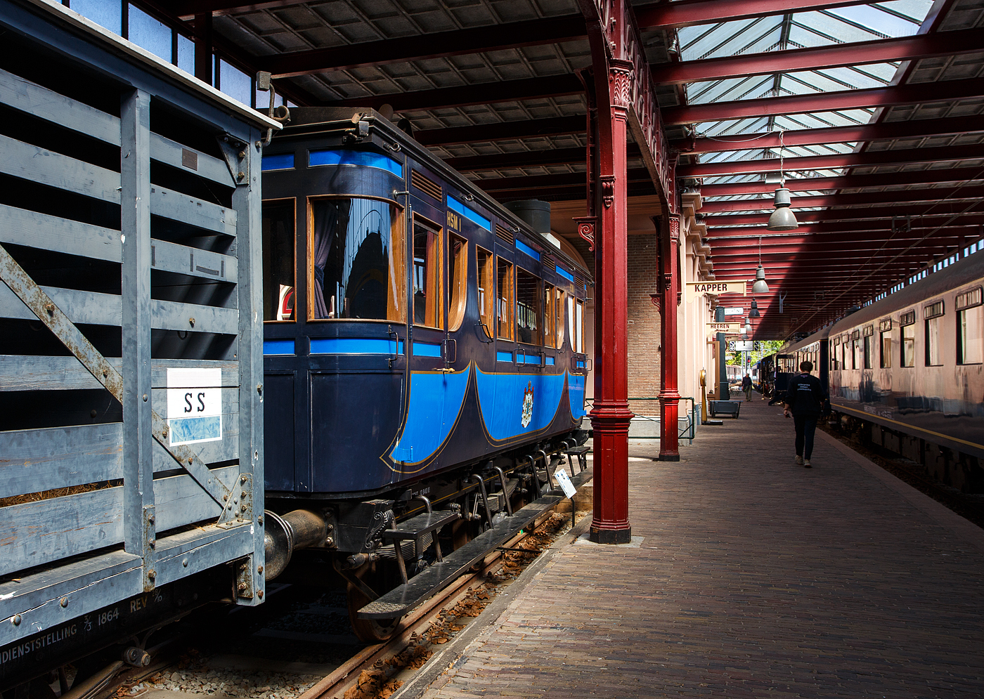 Der königliche Salonwagen HSM Sr 1 (Replikat) am 29 April 2025 im Het Spoorwegmuseum (bis 2005 NSM - Nederlands Spoorwegmuseum / Niederländischen Eisenbahnmuseum) in Utrecht im ehemaligen Bahnhof Maliebaanstation.

Der ursprüngliche Salonwagen Nummer 1 (Sr 1) wurde speziell für Anna Paulowna von Holstein-Gottorp-Romanow, Großfürstin von Russland und Witwe von König Willem II. (Wilhelm Friedrich Georg Ludwig von Oranien-Nassau), von 1840 bis 1849 König der Niederlande und in Personalunion Großherzog von Luxemburg, die selbst darauf bestand, gebaut. Sie wollte mit ihrem eigenen Wagen von Soestdijk nach Den Haag fahren können. Der Sr 1 war einer der ersten königlichen Wagen (Royal Wagen) und wurde 1864 in der Haarlemer HSM-Werkstatt gebaut. Am 21. November 1864 wurde der noch nummerierte Wagen inspiziert und für in Ordnung befunden. Bis zur ministeriellen Genehmigung vergingen mehrere Wochen. Im Winter zog die königliche Gesellschaft den warmen Kamin einer Zugfahrt vor, die nur mit Öfen beheizt wurde. Anna Paulowna hat ihn nie benutzt, da sie noch vor der Indienststellung des Wagens am 1. März 1865 nach mehrwöchiger Krankheit in Den Haag verstarb. Der Wagen wurde aber regelmäßig von Prinz Frederik, dem jüngeren Bruder von König Wilhelm II., genutzt.

Der zweiachsige Sr 1 wurde mehrfach modifiziert. Er war für Breitspur (1.945 mm) gebaut worden, doch 1864 beschloss die HSM (bzw. HIJSM) - Hollandsche IJzeren Spoorweg-Maatschappij (Niederländischen Eisenbahn-Gesellschaft), die Gleise auf Normalspur (1.435 mm) umzubauen. Erst wurde neben dem eingleisigen Breitspurgleis, auf der gesamten Strecke Amsterdam – Haarlem – Den Haag – Rotterdam. ein zweites Gleis in Normalspur (1.435 mm) verlegt, um auch in Zukunft den Anschluss an das übrige Europa nicht zu verpassen. Dieses eingleisige Normalspur-Gleis wurde am 2. Mai 1866 fertiggestellt.

Der Innenraum des Wagens wurde 1884 vollständig renoviert, im Zuge der Renovierung wird der Waggon auch mit einer Toilette und einem Waschbecken ausgestattet. Die Sr 1 des Eisenbahnmuseums ist ein Nachbau aus dieser Zeit. Das Replikat wurde 2010 von Kloosterboer in Purmerend speziell für das Museum gebaut. Toilette und Waschbecken sind original, dies sind die einzigen Originalgegenstände, die erhalten geblieben sind. Anschließend wurde die Karosserie des Salonwagens auf ein neues dreiachsiges Normalspur-Fahrgestell gesetzt. Zum ersten Mal wurde ein neuer Radtyp verwendet, bestehend aus sechzehn Teakholzsegmenten um eine Nabe aus Schmiedeeisen, mit einem Radband aus Schmiedeeisen rundherum, System Mansell.

Die Nummer Sr 1 und die Abkürzung HSM erhielt der Wagen erst 1870, als in Den Haag die Verbindungskurve zu den NRS-Strecken eingerichtet wurde und der Verdacht aufkam, dass der Wagen auch auf ausländischen Strecken gefahren werden könnte.

Nachdem Prinz Frederik 1881 im Alter von 84 Jahren starb, wurde der Salonwagen kaum noch genutzt. Die HSM gab dem Wagen deshalb im Jahr 1884 eine andere Bestimmung. Ein Teil eines Endabteils wurde abgetrennt und mit einer Toilette und einer Waschgelegenheit versehen. Anstelle einer Ölbeleuchtung war der Wagen mit einer Gasbeleuchtung ausgestattet. Die Öfen wurden durch eine Brikettheizung ersetzt. Der Wagen wurde dann Menschen zur Verfügung gestellt, die es sich leisten konnten, den harten niederländischen Wintern zu entfliehen. Also VIP-Wagen „avant la lettre“.

Im Jahr 1905 nutzte die damalige Königin Wilhelmina nutzte den Wagen noch einmal für einen Besuch in der Provinz Friesland. 1908 wurde der Sr 1 außer Dienst gestellt und verschrottet.

Im Jahr 2009 beauftragte das Eisenbahnmuseum die Firma Kloosterboer in Purmerend mit dem Bau einer Nachbildung des Sr 1. Der Waggon, dessen Bau von der Bank-Giro-Loterij gesponsert wurde, spielte 2010 eine Hauptrolle in der Ausstellung „Royal Class“.

TECHNISCHE DATEN (Replikat)
Hersteller: Fa. Kloosterboer Decorbouw, Purmerend
Baujahr: 2010
Spurweite:1.435 mm
Anzahl der Achsen: 3
Länge über die Puffer: 8,76 m
Gewicht: 12,84 t
Betriebsfähig: nein
