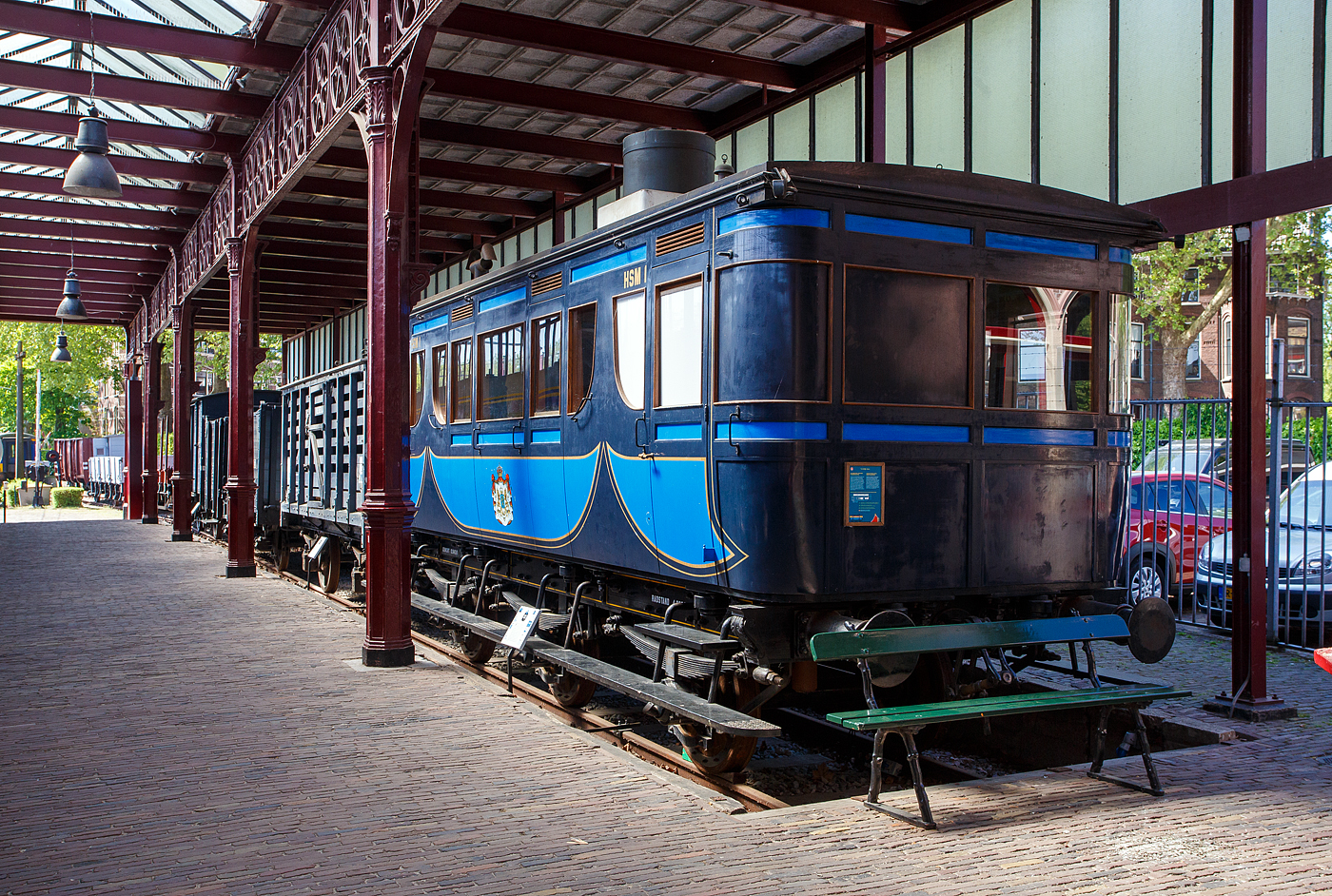 Der königliche Salonwagen HSM Sr 1 (Replikat) am 29 April 2025 im Het Spoorwegmuseum (bis 2005 NSM - Nederlands Spoorwegmuseum / Niederländischen Eisenbahnmuseum) in Utrecht im ehemaligen Bahnhof Maliebaanstation.

Der ursprüngliche Salonwagen Nummer 1 (Sr 1) wurde speziell für Anna Paulowna von Holstein-Gottorp-Romanow, Großfürstin von Russland und Witwe von König Willem II. (Wilhelm Friedrich Georg Ludwig von Oranien-Nassau), von 1840 bis 1849 König der Niederlande und in Personalunion Großherzog von Luxemburg, die selbst darauf bestand, gebaut. Sie wollte mit ihrem eigenen Wagen von Soestdijk nach Den Haag fahren können. Der Sr 1 war einer der ersten königlichen Wagen (Royal Wagen) und wurde 1864 in der Haarlemer HSM-Werkstatt gebaut. Am 21. November 1864 wurde der noch nummerierte Wagen inspiziert und für in Ordnung befunden. Bis zur ministeriellen Genehmigung vergingen mehrere Wochen. Im Winter zog die königliche Gesellschaft den warmen Kamin einer Zugfahrt vor, die nur mit Öfen beheizt wurde. Anna Paulowna hat ihn nie benutzt, da sie noch vor der Indienststellung des Wagens am 1. März 1865 nach mehrwöchiger Krankheit in Den Haag verstarb. Der Wagen wurde aber regelmäßig von Prinz Frederik, dem jüngeren Bruder von König Wilhelm II., genutzt.

Der zweiachsige Sr 1 wurde mehrfach modifiziert. Er war für Breitspur (1.945 mm) gebaut worden, doch 1864 beschloss die HSM (bzw. HIJSM) - Hollandsche IJzeren Spoorweg-Maatschappij (Niederländischen Eisenbahn-Gesellschaft), die Gleise auf Normalspur (1.435 mm) umzubauen. Erst wurde neben dem eingleisigen Breitspurgleis, auf der gesamten Strecke Amsterdam – Haarlem – Den Haag – Rotterdam. ein zweites Gleis in Normalspur (1.435 mm) verlegt, um auch in Zukunft den Anschluss an das übrige Europa nicht zu verpassen. Dieses eingleisige Normalspur-Gleis wurde am 2. Mai 1866 fertiggestellt.

Der Innenraum des Wagens wurde 1884 vollständig renoviert, im Zuge der Renovierung wird der Waggon auch mit einer Toilette und einem Waschbecken ausgestattet. Die Sr 1 des Eisenbahnmuseums ist ein Nachbau aus dieser Zeit. Das Replikat wurde 2010 von Kloosterboer in Purmerend speziell für das Museum gebaut. Toilette und Waschbecken sind original, dies sind die einzigen Originalgegenstände, die erhalten geblieben sind. Anschließend wurde die Karosserie des Salonwagens auf ein neues dreiachsiges Normalspur-Fahrgestell gesetzt. Zum ersten Mal wurde ein neuer Radtyp verwendet, bestehend aus sechzehn Teakholzsegmenten um eine Nabe aus Schmiedeeisen, mit einem Radband aus Schmiedeeisen rundherum, System Mansell.

Die Nummer Sr 1 und die Abkürzung HSM erhielt der Wagen erst 1870, als in Den Haag die Verbindungskurve zu den NRS-Strecken eingerichtet wurde und der Verdacht aufkam, dass der Wagen auch auf ausländischen Strecken gefahren werden könnte.

Nachdem Prinz Frederik 1881 im Alter von 84 Jahren starb, wurde der Salonwagen kaum noch genutzt. Die HSM gab dem Wagen deshalb im Jahr 1884 eine andere Bestimmung. Ein Teil eines Endabteils wurde abgetrennt und mit einer Toilette und einer Waschgelegenheit versehen. Anstelle einer Ölbeleuchtung war der Wagen mit einer Gasbeleuchtung ausgestattet. Die Öfen wurden durch eine Brikettheizung ersetzt. Der Wagen wurde dann Menschen zur Verfügung gestellt, die es sich leisten konnten, den harten niederländischen Wintern zu entfliehen. Also VIP-Wagen „avant la lettre“.

Im Jahr 1905 nutzte die damalige Königin Wilhelmina nutzte den Wagen noch einmal für einen Besuch in der Provinz Friesland. 1908 wurde der Sr 1 außer Dienst gestellt und verschrottet.

Im Jahr 2009 beauftragte das Eisenbahnmuseum die Firma Kloosterboer in Purmerend mit dem Bau einer Nachbildung des Sr 1. Der Waggon, dessen Bau von der Bank-Giro-Loterij gesponsert wurde, spielte 2010 eine Hauptrolle in der Ausstellung „Royal Class“.

TECHNISCHE DATEN (Replikat)
Hersteller: Fa. Kloosterboer Decorbouw, Purmerend
Baujahr: 2010
Spurweite:1.435 mm
Anzahl der Achsen: 3
Länge über die Puffer: 8,76 m
Gewicht: 12,84 t
Betriebsfähig: nein
