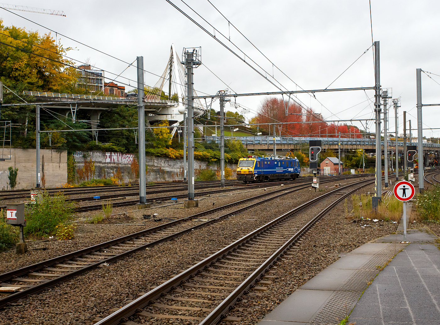 Der Oberleitungsmesstriebwagen (Autorail de Mesure Caténaire) EM 201 mit der UIC-Nummer 99 88 9165 201-3 B-INFBL, ein Geismar Eye Dragon VMB2214-IC der belgischen INFRABELverlässt am 21 Oktober 2025 den Bahnhof Lüttich-Guillemins (Gare de Liège-Guillemins) hinauf in Richtung Ans bzw. Brüssel.

Die Infrabel ist das 2005 aus der Privatisierung der Eisenbahn in Belgien hervorgegangene Infrastrukturunternehmen. Es ist vollständig im Eigentum des belgischen Staates und hat etwa 12.750 Mitarbeiter. Seine Aufgaben beinhalten die Instandhaltung sowie den Ausbau des 3602 km langen belgischen Schienennetzes, die Vergabe und Abrechnung von Fahrplantrassen sowie die Koordination des belgischen Zugverkehrs.

Die Infrabel hat 3 dieser Messtriebwagen vom Typ Geismar VMB2214-IC, die zwischen 2010 und 2014 gebaut wurden. Sie sind als Serie EM200 eingeordnet.

TECHNISCHE DATEN des Messtriebwagen:
Spurweite: 1.435 mm (Normalspur)
Achsfolge: Bo-Bo
Länge über Puffer: 21.240 mm
Drehzapfenabstand: 14.000 mm	
Achsabstand im Drehgestell: 2.500 mm
Gewicht: 89 t
min. Kurvenradius: R 90 m
