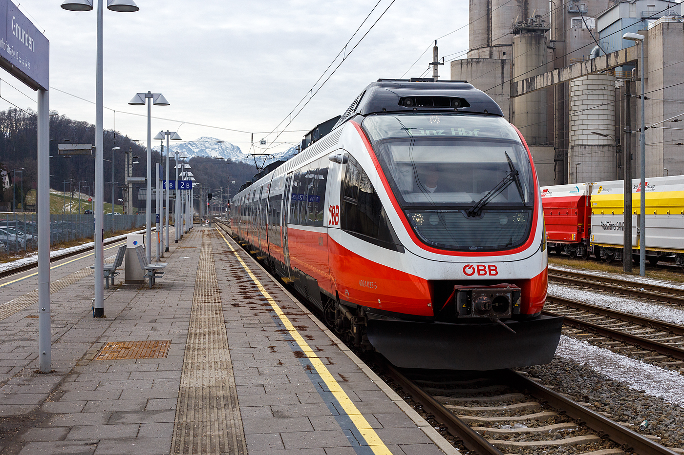 Der ÖBB 4024 023-5, ein vierteiliger elektrischer TALENT, erreicht am 14 Januar 2025, als REX 70 (4409) nach Linz Hbf über Attnang-Puchheim, den Bahnhof Gmunden. Rechts das Zementwerk Hatschek in Gmunden der Rohrdorfer Zement GmbH.