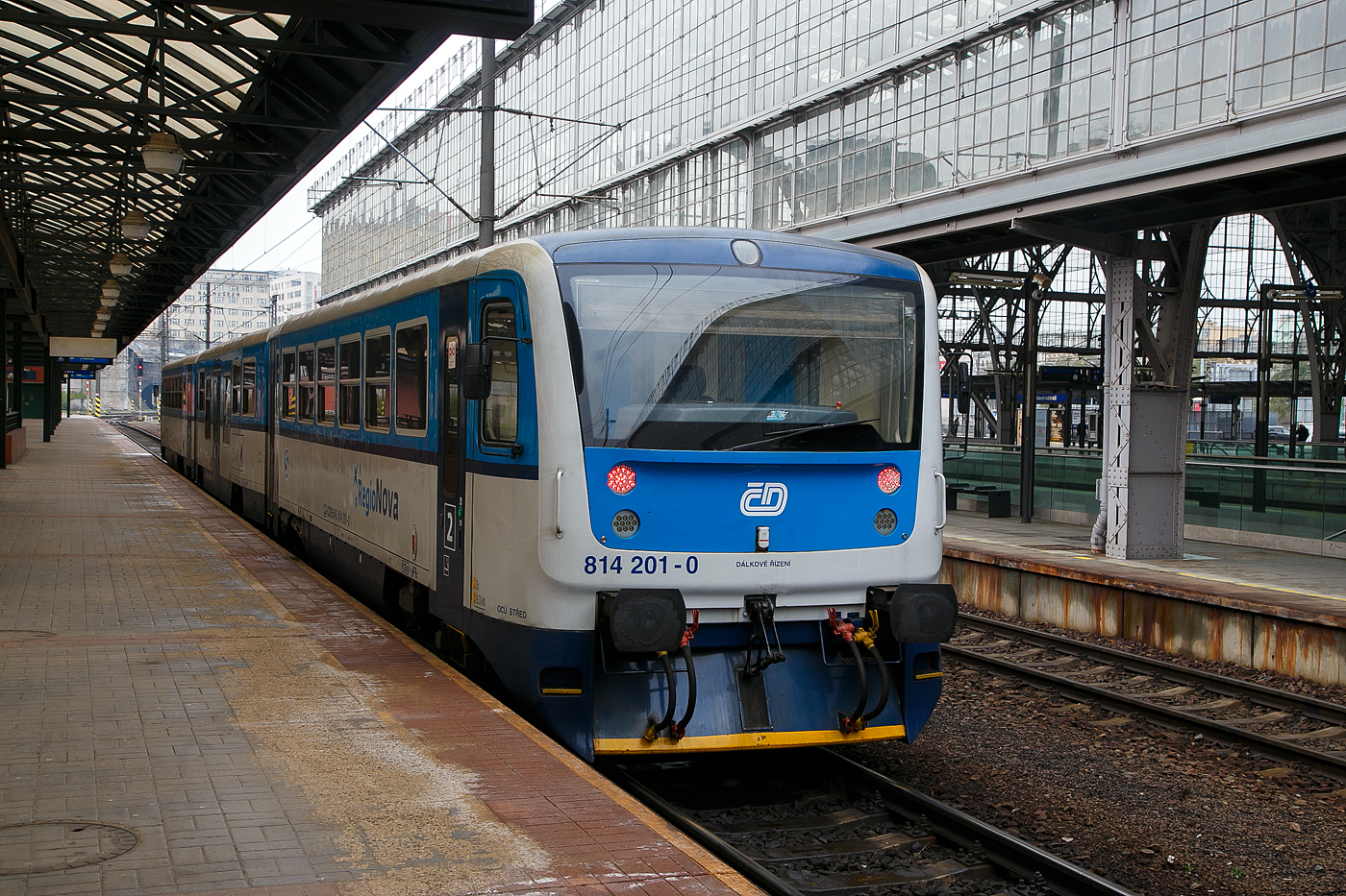 Der RegioNova „Trio“ 814 201-0 / 014 0xx / 814 202-9 steht am 23.11.2022 als Regionalzug im Hauptbahnhof Prag (Praha hlavní nádraží) zur Abfahrt bereit.

Diese dreiteiligen Fahrzeuge der ČD-Baureihe 814.2/014/814.2 entstanden im Rahmen eines Rekonstruktionsprogrammes (2007 bis 2012) aus den Fahrzeugen der ČD-Baureihe 810 bzw. Beiwagen der Reihe 010. Von den ČD werden sie als „RegioNova“ vermarktet.Der Einsatz des Fahrzeuges ergibt vor allem Energieeinsparungen, eine höhere Traktionsgeschwindigkeit und dadurch eine Straffung der Fahrpläne. 

Die Baureihe 814.2:
Eine Weiterentwicklung der Baureihe 814.0 ist die Baureihe 814.2. Eine Einheit besteht anstatt aus einem Motor- und einem Steuerwagen aus zwei Motorwagen (BR 814.2) und einem Mittelwagen (BR 014). Die dreiteiligen Züge bieten 127 Sitzplätze anstatt bei den zweiteiligen Wagen 76. Triebwagen der Baureihe 814.2 sind seit 2007 im Einsatz.

Technische Merkmale:
Wesentliche Veränderungen gegenüber der Ursprungsbauart sind eine neue, leistungsfähigere Antriebsanlage mit dem Dieselmotor LIAZ ML 640 SE (TEDOM TD 242 RH TA25) und dem hydromechanischen Getriebe VOITH DIWA 864.3E, eine bequemere Innenausstattung mit behindertengerechter Toilette, bessere Arbeitsbedingungen für den Lokführer, bessere Fahreigenschaften und geringere Umweltauswirkungen der Antriebsanlage. Die Regionova sind nach wie vor mit Schraubenkupplung ausgerüstet und somit mit anderen Fahrzeugen freizügig kuppelbar.

Im Mittelwagen (BR 014), der zwischen den Radsätzen einen Niederflurbereich auf etwa 50 % der Wagenlänge aufweist, befinden sich das Traglastenabteil, eine Auffahrrampe für Rollstühle, die Toilette und 31 Sitzplätze. Der Einstieg liegt in diesem Bereich in Wagenmitte. Der Triebwagen, in normaler Bodenhöhe aufgebaut, besitzt Fahrgastabteile mit 48 Sitzplätzen. Die Antriebsanlage liegt wie bei der Ursprungsbauart unter dem Wagenboden, auch die Lage der Einstiege wurde bei den Triebwagen nicht verändert.

Beschreibung von Škoda:
Die Zuggarnituren entstehen durch eine Rekonstruktionen und Modernisierung der ursprünglichen Wagen, die in den Jahren 1973-1983 hergestellt wurden. Der Hauptbeitrag der Rekonstruktion ist neben der Erhöhung der Qualität des Reisens auf den Regionalstrecken auch die Reduzierung der Kosten für den Betrieb und die Wartung.

Die modernisierten Einheiten haben einen geringeren Verbrauch und in den Endstationen müssen sie nicht umgespannt werden. Der Zug Regionova  Trio  besteht aus zwei Triebwagen und einem Niederflur-Zwischenwagen, der die Beförderung von Personen mit eingeschränkter Mobilität und von Eltern mit Kinderwagen erleichtert.. In den Zuggarnituren ist genügend Platz auch für größeres Gepäck. Eine komplette Modernisierung machte auch der Zugführerraum durch.

TECHNISCHE DATEN Regionova „Trio“:
Hersteller (Umbau): Pars Nova in Šumperk (gehört zu Škoda)
Spurweite: 1.435 mm (Normalspur)
Achsformel: 1'A' + 1'1' + A'1'
Länge über Puffer: 42.410 mm
Wagenkastenbreite: 3.073 mm
Höhe: 3.420 mm
Leergewicht: 62,3 t
Radsatzfahrmasse: 9,75 t
Höchstgeschwindigkeit: 80 km/h
Installierte Leistung: 242 kW (bei 1.950 U/min)
Anfahrzugkraft: 54 kN
Motorentyp: 2x TEDOM TD 242 RH TA25 (LIAZ ML 640 SE)
Getriebe: 2 x Voith Diwa 864.3E
Leistungsübertragung: hydromechanisch
Sitzplätze: 127
Fußbodenhöhe: 570 mm (Niederflurteil)
Kleinster befahrbarer Gleisbogen: R 120 m
Bremse: DK-P
