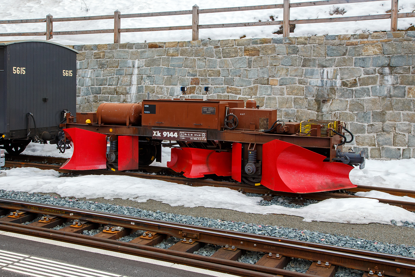 Der RhB Spurpflug Xk 9144 (Baujahr 1968 bei Ernst Stadler) abgestellt am 21.03.2023 im Bahnhof Pontresina.

Neben der Erneuerung des Bestandes an Schneeschleudern wurde ab Mitte der sechziger Jahre auch der Park der Schnee- und Spurpflüge modernisiert. Beschleunigt wurde die Entwicklung durch die Tatsache, dass mit den alten bemannten Pflügen immer wieder Unfälle passierten. Die alten Fahrzeuge, die nur geschoben werden konnten, besaßen einen manuell zu bedienenden heb- und senkbaren, unter Schienenoberkante reichenden Spurpflug. bei schlechter Sicht wurde der Spurpflug bei Wegübergängen und ähnlichen Hindernissen oft zu spät angehoben, und Entgleisungen mit Personenverletzungen und Materialschäden waren die Folge. Seitens des Bahndienstes rief man daher nach einem unbemannten, vom Führerstand der Schublokomotive aus fernsteuerbaren Spur- und Schneepflug.

1966 wurde dann der erste Prototyp-Pflug gemeinsam mit der Firma Ernst Stadler (heute Stadler Rail AG) speziell für die Bedüfrnisse der RhB entwickelt und gebaut, der X 9141. er war als Zweirichtungspflug konzipiert, kann also bei vorwiegender Räumung zwischen den Schienen auch gezogen werden. Neben kräftigen Stirn-Schneepflügen besitzt er einen hydraulisch senk- und hebbaren Spurpflug zwischen den Achsen. Der Öldruck für die Hydraulik wird in einem Pumpenaggregat auf dem Fahrzeug selbst mittels Achsantrieb erzeugt. Die Steuerung des Spurpfluges erfolgt über ein Steuerkabel mit Schaltkasten aus dem Führerstand der Schub- oder Zuglokomotive. Damit wird nicht nur Personal eingespart, es werden vor allem auch harte und gefährliche Arbeitsbedingungen eliminiert. Die eher konservativen Bahnmeister waren gegenüber dem neuen „Vehikel“ anfangs sehr skeptisch. Der Pflug X 9141 wurde dann aber immer beliebter, so dass 1968 drei weitere und bis 1989 nochmals drei Spurpflüge beschafft wurden, die sich vom Prototyp nur in Kleinigkeiten unterscheiden. Auch die FO stellte 1976 ein derartiges Fahrzeug in Dienst. Die alten Schneepflüge der RhB wurden daraufhin fast alle nach und nach verschrottet oder verkauft. Die modernen hydraulischen Pflüge sind über das ganze RhB-Netz verteilt. Besonders häufig müssen sie auf der Berninabahn eingesetzt werden, die stark mit Schneeverfrachtungen durch Wind zu kämpfen hat.

TECHNISCHE DATEN:
Hersteller: Ernst Stadler, Zürich
Baujahr: 1968
Spurweite: 1.000 mm
Gewicht: 9.40 t
Länge über Puffer: 7.340 mm
Achsabstand: 3.300 mm
Geschwindigkeit: 60 km/h
