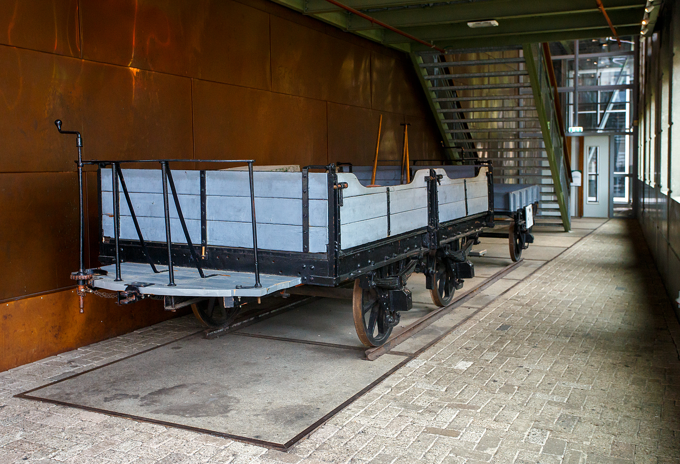 Der zweiachsige offene Pferdebahn-Güterwagen NTM G 1 und der einachsige offene Pferdebahn-Gepäckwagen NTM Dk 2 am 24 Juni 2025 im Het Spoorwegmuseum (bis 2005 NSM - Nederlands Spoorwegmuseum / Niederländischen Eisenbahnmuseum) in Utrecht im ehemaligen Bahnhof Maliebaan. Ein Eisenbahnmuseum das zum Verweilen einlädt. Übrigens Het vor Spoorwegmuseum heißt einfach „Das“, so heißt übersetzt das Museum einfach „Das Eisenbahnmuseum“. 

Die Wagen wurden beide von Beijnes, offiziell Koninklijke Fabriek van Rijtuigen en Spoorwagens J.J. Beijnes (Königliche Fabrik für Kutschen und Eisenbahnwagen J.J. Beijnes) in Haarlem gebaut und an die damalige NTM - Nederlandsche Tramweg Maatschappij (Niederländische Straßenbahngesellschaft) geliefert. Der NTM G 1 wurde 1880 und der NTM Dk 2 wurde 1881 gebaut. 

TECHNISCHE DATEN:
Gebaute Anzahl (Serie): 1 (G1) / 3 (Dk 2, Serie 1-3)
Spurweite: 1.435 mm (Normalspur)
Achsen: 2 (G1) / 1 (Dk 2)
Leergewicht: 600 kg (G1) / 300 kg (Dk 2)
Höchstgeschwindigkeit: 20 km/h

Die NTM:
Die NTM - Nederlandsche Tramweg Maatschappij (Niederländische Straßenbahngesellschaft) war ein Straßenbahn- und Busunternehmen, das zwischen 1880 und 1956 für den Bau, den Betrieb und die Instandhaltung von Straßenbahnlinien in Friesland verantwortlich war. Trotz ihres Namens war diese Straßenbahngesellschaft ausschließlich in Friesland und den angrenzenden Teilen tätig. Die letzte Tram fuhr 1956, als regionales Busunternehmen blieb die NTM bis 1971 aktiv.

Geschichte:
Die NTM wurde am 24. April 1880 in Utrecht gegründet, war aber später in Heerenveen ansässig. Ursprünglich plante das Unternehmen den Bau von Straßenbahnlinien in den Niederlanden, konzentrierte sich jedoch letztendlich auf Friesland und erweiterte das Angebot um einige benachbarte Provinzen.

Die letzten verbliebenen Straßenbahnlinien der ehemaligen NTM wurden 1956 an die NS (Niederländische Eisenbahnen) übertragen, die 1985 die letzte Straßenbahnlinie zwischen Drachten und Groningen, die damals nur noch dem Güterverkehr diente, stilllegte.

Pferdebahnen:
Die ersten von der NTM gebauten Linien wurden mit Pferdebahnen betrieben. Die erste Pferdebahnlinie führte von Dokkum nach Veenwouden und wurde am 6. Oktober 1880 eröffnet. Diese und alle nachfolgenden Linien waren in Normalspur (Spurweite 1.435 mm) ausgeführt. Ein Jahr später, am 19. September 1881, wurde die Strecke Veenwouden–Bergumerdam eröffnet, die 1896 bis Suameer verlängert wurde. 1898 wurde die Pferdebahnlinie Harkezijl–Makkum eröffnet, während die Pferdebahnlinie Berlikum–Sint Annaparochie schließlich 1900 eröffnet wurde. Diese letzte Linie wurde 1917 stillgelegt, während die Verbindung Harkezijl–Makkum bis zum 16. Juli 1930 in Betrieb blieb. Dies war die letzte Pferdebahnlinie in den Niederlanden.

Ab 1913 (Suameer–Veenwouden) und 1926 (Veenwouden–Dokkum) wurde die Pferdebahn durch die Dampfbahn ersetzt. Die Pferdebahnlinien waren leichter als andere Linien, daher mussten die Schienen durch schwerere ersetzt werden, bevor die schwereren Dampflokomotiven fahren konnten.

Dampfstraßenbahnen:
65 Jahre lang bildete die Dampfstraßenbahn den größten Teil der NTM, die in ihrer Blütezeit einen großen Teil der Provinz Friesland abdeckte. Die NTM war damit eine der größten Dampfstraßenbahngesellschaften der Niederlande.

Die erste Dampfstraßenbahn fuhr am 11. Januar 1882 auf der Straßenbahnlinie Sneek – Bolsward. Im selben Jahr kamen die Strecken Bolsward–Harlingen, Heerenveen–Joure und Heerenveen–Gorredijk hinzu, die 1884 bis nach Drachten verlängert wurden. 1886 wurde die fehlende Verbindung zwischen Joure und Sneek fertiggestellt. Zu diesem Zeitpunkt war die durchgehende Straßenbahnlinie Harlingen–Bolsward–Sneek–Joure–Heerenveen–Gorredijk–Drachten fertiggestellt. Zehn Jahre später, 1896, wurde die Straßenbahnlinie Veenwouden–Suameer nach Drachten verlängert. Diese Straßenbahnlinien hatten alle Normalspur, so dass Güterwagen von der Dampfstraßenbahn auf das nationale Eisenbahnnetz übertragen werden konnten.

Die Straßenbahnlinien dienten sowohl dem Personen- als auch dem Güterverkehr, wobei der Güterverkehr auf einigen Strecken den Personenverkehr um viele Jahre überdauerte. Das gesamte Netz bestand nur etwa 17 Jahre, da 1933 die letzte eröffnete Linie von Hijkersmilde entlang des Drentsche Hoofdvaart-Kanals nach Meppel als erste stillgelegt wurde. 

Am 13. August 1939 wurden mehrere Verbindungen eingestellt. Die verbleibenden Straßenbahnlinien blieben bis nach dem Zweiten Weltkrieg in Betrieb, doch 1947 wurde der größte Teil des Netzes stillgelegt. 

Lediglich die letzte Linie Drachten – Groningen blieb noch längere Zeit in Betrieb. Das in den 1950er Jahren in Drachten gegründete Philips-Werk war sein Hauptkunde. Bis in die 1980er Jahre wurde auf der Philips-Linie durch die NS regelmäßiger Güterverkehr mit Diesellokomotiven der Baureihe NS 2400 betrieben. 1973, 1975 und 1976 kehrte die Dampfstraßenbahn zurück, als die Dampfstraßenbahn Hoorn-Medemblik (SHM) auf dieser alten Straßenbahnlinie verkehrte. Die letzte Fahrt auf der gesamten Strecke erfolgte mit Wadlopern am 30. April 1985, eine weitere Fahrt nach Roden am 7. Juni 1985. 1988 wurde die Strecke stillgelegt. Dies markierte das Ende der Geschichte der friesischen Straßenbahnlinien.
