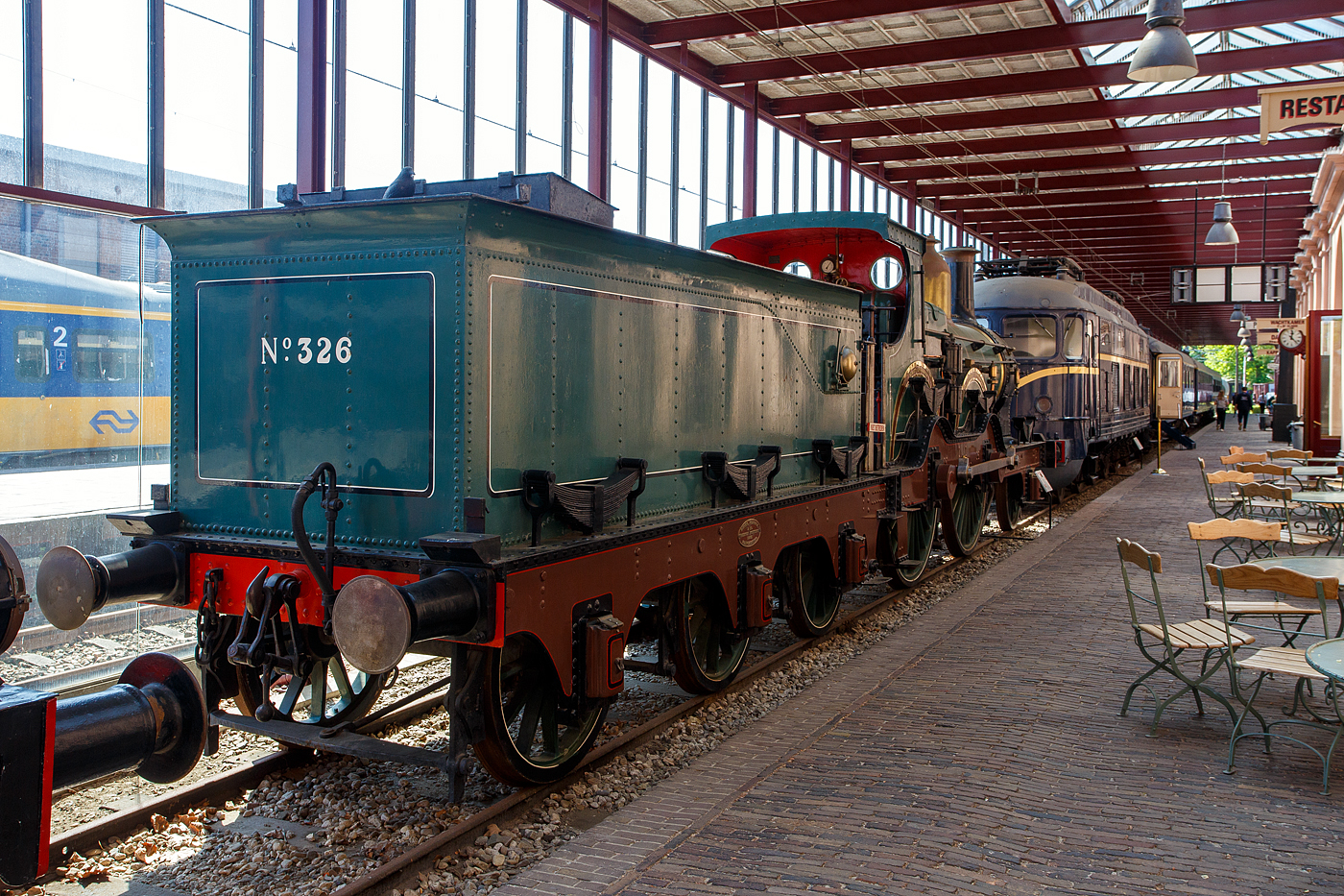 Die 1881 gebaute 1B Dampflokomotive SS 326 „Grote Groenen“ (Große Grüne), ab 1921 NS 1326 (NS-Baureihe 1300), am 29 April 2025 im Het Spoorwegmuseum (bis 2005 NSM - Nederlands Spoorwegmuseum / Niederländischen Eisenbahnmuseum) in Utrecht im Bahnhof Maliebaan.   

Die Dampflok wurde 1881 von Beyer Peacock & Co. Ltd. in Manchester (GB) unter der Fabriknummer 2101 gebaut und an die damalige SS - Maatschappij tot Exploitatie van Staatsspoorwegen (deutsch: Gesellschaft zum Betrieb von Staatseisenbahnen) geliefert. Ab 1921, nach der Zusammenlegung des Rollmaterials der SS und der NRS, wurde die Lok zur NS 1326. Die Lokomotive 1326 wurde 1939 außer Dienst gestellt und für das Eisenbahnmuseum erhalten. Am Ende des Zweiten Weltkriegs wurde sie von den zurückweichenden Deutschen Truppen in Maastricht schwer beschädigt. Im Jahr 1956 wurde sie schließlich von der Hauptwerkstatt in Tilburg in ihren Originalzustand zurückversetzt und anschließend ins Eisenbahnmuseum gebracht. Die Lokomotive 326 gilt als eines der Meisterwerke des Museums.

Die NS 1300-Serie war eine Serie von 179 Dampflokomotiven der Niederländischen Eisenbahnen (NS), die zwischen 1880 und 1895, an ihre Vorgängergesellschaften, Maatschappij tot Exploitatie van Staatsspoorwegen (SS) und Noord-Brabantsch-Duitsche Spoorweg-Maatschappij (NBDS) geliefert wurden.

Durch die Erfindung und Anwendung der kontinuierlichen Druckluftbremse (Westinghouse-Bremse) konnte die Geschwindigkeit der Züge bei gleichbleibendem Bremsweg deutlich erhöht werden. Dafür waren nun leistungsstärkere und schnellere Lokomotiven erforderlich, die die Maatschappij tot Exploitatie van Staats-Spoorwegen (SS) in diesem Lokomotiventyp vorfand. Das niederländisch-englische Design der Baureihe 301 – 479 (NS 1301 – 1479) erwies sich als sehr geeignet für den Schnellzugdienst, war aber auch im Güterverkehr nützlich. Die Lokomotiven wurden über einen Zeitraum von 15 Jahren gebaut und bildeten mit insgesamt 179 Stück die größte jemals von der SS und NS betriebene Dampflokomotiven-Baureihen. Sie fuhren auf allen wichtigen Staatsbahnstrecken im ganzen Land, einschließlich der schweren Postzüge zwischen Vlissingen und Venlo. 

Die eindrucksvollen Lokomotiven, die für die damalige Zeit in einem hellgrünen Farbton mit braunen Rahmenplatten lackiert waren, erhielten bald ihren Spitznamen „Grote Groenen“ (Große Grüne). 1919 wurde die Serie um 3 baugleiche Lokomotiven SS 476 – 478 erweitert, die von der Noord-Brabantsch – Duitsche Spoorweg-Maatschappij (NBDS 6, 7 und 11) stammten. Schließlich wurde die abweichende Verbundmaschine 701 mit einem Hoch- und einem Niederdruckzylinder weitgehend der Serie angeglichen und in 479 um nummeriert.

Bedingt durch den Ersten Weltkrieg wurde 1917 eine Zweckgemeinschaft der unabhängigen Eisenbahngesellschaften HSM (Hollandsche IJzeren Spoorweg-Maatschappij) und SS (Maatschappij tot Exploitatie van Staatsspoorwegen) gegründet. Die beiden Gesellschaften errichteten einen gemeinsamen Bahnbetrieb, blieben aber rechtlich unabhängig. Dies änderte sich 1938, als HIJSM und SS vollständig fusionierten und in der AG NS (Nederlandse Spoorwegen, früher Nederlandsche Spoorwegen geschrieben) aufgingen. Das Rollmaterial wurde bereits 1921 zusammengelegt, so wurden die Lok zur NS 1326 nummeriert. 

Die dreiachsigen Tender der SS 301-398 hatten einen Wasserinhalt von 10,3 m³. Ab der 399 wurde der Wasserinhalt der Tender durch eine Vertiefung zwischen den Rahmenplatten auf 13 m³ erhöht. Später wurde die Wasserkapazität der Tender der Linien 301–398 auf die gleiche Weise erhöht.
	
TECHNISCHE DATEN:
SS-Serie: Grote Groenen, ab 1921 NS 1300
Hersteller: Beyer Peacock & Co. Ltd. in Manchester (GB)
Gebaute Anzahl: 179
Spurweite: 1.435 mm (Normalspur)
Achsfolge: 	1 B (engl. 2-4-0), gekuppelt mit dreiachsigem Tender
Länge über Puffer: 15.395 mm
Treibraddurchmesser: 2.150 mm (neu) / 2134 mm (abgenutzt)
Laufraddurchmesser (Lok und Tender): 1.240 mm (neu) / 1.219 mm (abgenutzt)
Höhe: 4.115 mm
Höchstgeschwindigkeit: 90 km/h
Rostfläche: 2,10 m²
Gesamtheizfläche: 103 m²
Kesselüberdruck: 10,3 kg/cm²
Anzahl der Zylinder: 2 (Ø 457 mm x 660 mm Hub)
Steuerung: Stephenson
Eigengewicht: 75 t (Lok 42 t und Tender 33 t)
Anhängelast: 4.620 kg
Wasservorrat: 13 m³ (urspr. 10,3 m³)
Kohlevorrat: 4 t
