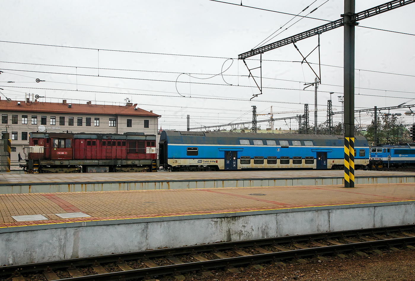 Die ČD 742 086-2 (CZ- ČD 92 54 2 742 086-2) fährt am 23.11.2022, mit dem  2. Klasse klimatisierten Doppelstock-Reisezugwagen, CD-CZ 50 54 26-18 141-6, der Gattung Bdmteeo 296 (ex CD-CZ 50 54 26-18 141-6, Bmto 292), in den Prager Hauptbahnhof (Praha hlavní nádraží) ein. Der 44 t schwere Wagen verfügt über 126 Sitzplätze, 8 Stellplätze für Fahrräder und ein geschlossenes WC-System.

Die Diesellok  Kocour   oder  Tranzisto   (Kater, Transistor):
Die ČSD-Baureihe T 466.2, ab 1988 Baureihe 742 sind dieselelektrische Güterzug- und Rangierlokomotiven der ehemaligen Tschechoslowakischen Staatsbahn (ČSD). Die Entwicklung begann 1970 mit den beiden Prototypen der BR T 475.15 (744.5). 

Das Leistungswachstum in der Motortraktion sowie die Notwendigkeit von Fortschritten bei der Erneuerung der Dampftraktion und der künftigen Typenvereinheitlichung des Motorlokparks veranlassten das Verkehrsministerium, die Beauftragung der Entwicklung und anschließenden Produktion einer neuen Lokomotive zu prüfen. Diese sollte für mittelschweren bis schweren Rangierdienst, leichteren Gleisdienst, aber auch im Güter- und Personenverkehr, bestimmt sein.

Zwei Prototyp-Lokomotiven der Reihe T 475.15 (744.5) wurden 1970 von ČKD in Praha gebaut, wurden aber von der ČSD als ungenügend abgelehnt. Dies lag hauptsächlich an ihrem Führerstand,  während die ČSD einen Turmführerstand mit guter Sicht verlangte, hatten diese Lokomotiven einen Führerstand neben dem hinteren Ende der Lokomotive, sodass die Aussicht nicht sehr zufriedenstellend war. Die Maschinen der Baureihe T 475.15 wurden daher verworfen und stattdessen die neuen Lokomotiven der Baureihe T 466.0 (735) produziert. Die Produktion erfolgte ab 1972 im Turčianské strojárny in Martin. 1973 begann bei ČKD Prag die Produktion neuer Lokomotiven der Reihe T 448.05 (740.5), die für den Bedarf großer Industrieunternehmen und für den Export bestimmt waren. Die Produktion von Lokomotiven T 466.0 (735) bei TS Martin verzögerte sich noch, die Entwicklung von Lokomotiven der Baureihe T 466.1 blieb erfolglos, außerdem war geplant, die Produktion von Lokomotiven bei TS Martin einzustellen und das Werk auf die Waffenproduktion zu konzentrieren . Auch die bereits produzierten T 466.0 (735) Maschinen waren im Betrieb sehr unzuverlässig. Die Situation in der Flotte der ČSD-Motorlokomotiven ist daher unerträglich geworden. Deshalb hat sich die ČSD eine Notlösung einfallen lassen: 1976 bestellten sie bei der ČKD 60 neue Lokomotiven der Baureihe T 466.2 (742), die genau aus den Industriemaschinen der T 448.05 (740.5) entstehen sollten. Die Serie, die bereits seit drei Jahren in der Industrie im Einsatz war, mit zudem sehr guten Ergebnissen. Die Liste der erforderlichen Umbauten war recht lang: Gewichtsreduzierung, Umbau des Triebwerks, Einbau einer Zugsicherung, Umbauten im elektrischen Teil, Umbau der Bremsen.1977-78 wurden 60 Lokomotiven der 1. Serie gebaut geliefert und die neuen Maschinen wurden fast sofort auf CSD in Betrieb genommen. Die 2. Serie folgte sofort und eine weitere danach. Die Produktion der Lokomotiven T 466.2 (742) für die ČSD endete mit der 9. Serien im Jahr 1986; insgesamt erwarb ČSD 453 dieser Lokomotiven. Während der langjährigen Produktion gab es mehrere partielle 

Modifikationen an der Konstruktion der Maschine – ab der 2. Serie mehrgliedrige Lenkung und Zugkraftwähler, ab der 3. Serie eine Knickbrücke seitlich am kürzeren Vorbau, ab der 6. Serie wurden Jalousien auf dem Dach der Lokomotive installiert und ab der 7. Serie neue Fahrmotoren. 41 Lokomotiven wurden für den Bedarf der Industrie geliefert, Maschinen auf Basis der Baureihe T 466.0 ČSD wurden auch nach Vietnam und Bangladesch geliefert. Nach der Produktion von Lokomotiven T 466.2 (742) für ČSD erfolgte 1987-88 die Produktion von abgeleiteten Lokomotiven T 466.3 (743) für Adhäsionsbetrieb auf Steilstrecken.

TECHNISCHE DATEN der BR 742, ex T 466.2:
Hersteller: ČKD Praha
Baujahre: 1977 bis 1986
Hergestellt e Anzahl: 453 für die ČSD (in 9 Serien), 41 weiter für andere
Spurweite: 1.435 mm (Normalspur)
Achsfolge: Bo'Bo'
Länge über Puffer: 13.580 mm ( am 4. Serie13.600 mm)
Höhe: 4.472 mm
Breite: 3 130 mm
Drehzapfenabstand: 6.700 mm
Achsabstand im Drehgestell: 2.400 mm
Treibrad-Ø: 1.000 mm (neu) / 920 mm (abgenutzt) 
Dieselmotor: 6-Zylinder-Viertakt-Reihen- Dieselmotor mit Direkt-Einspritzung und Turbolader vom Typ ČKD  K 6 S 230 DR
Motorhubraum: 64,75 Liter (Zylinder-Ø 230 mm / Kolbenhub 260 mm)
Kompressionsverhältnis: 12,5 : 1
Nenndrehzahl: 1.250 U/min (Leerlaufdrehzahl 510 U/min)
Motorgewicht (ohne Generator): 7.700 kg
Achsübersetzung: 1:4,8125
Dauermotorleistung: 883 kW (1.200 PS)
Leistung des Traktionsgenerators: 780 kVA
Leistungsübertragung: dieselelektrisch
Fahrmotorentyp: TE 005 E / ab 7. Serie TE 015 C
Antriebsmotorleistung: 195 kVA
Höchstgeschwindigkeit: 90 km/h
Dienstgewicht: 64 t
Anfahrzugkraft: 192kN
Dauerzugkraft: 121 kN
Max. Tankinhalt: 4.000 l
Kleinster bef. Halbmesser: R 80 m

Quellen: Wikipedia, atlaslokomotiv.net
