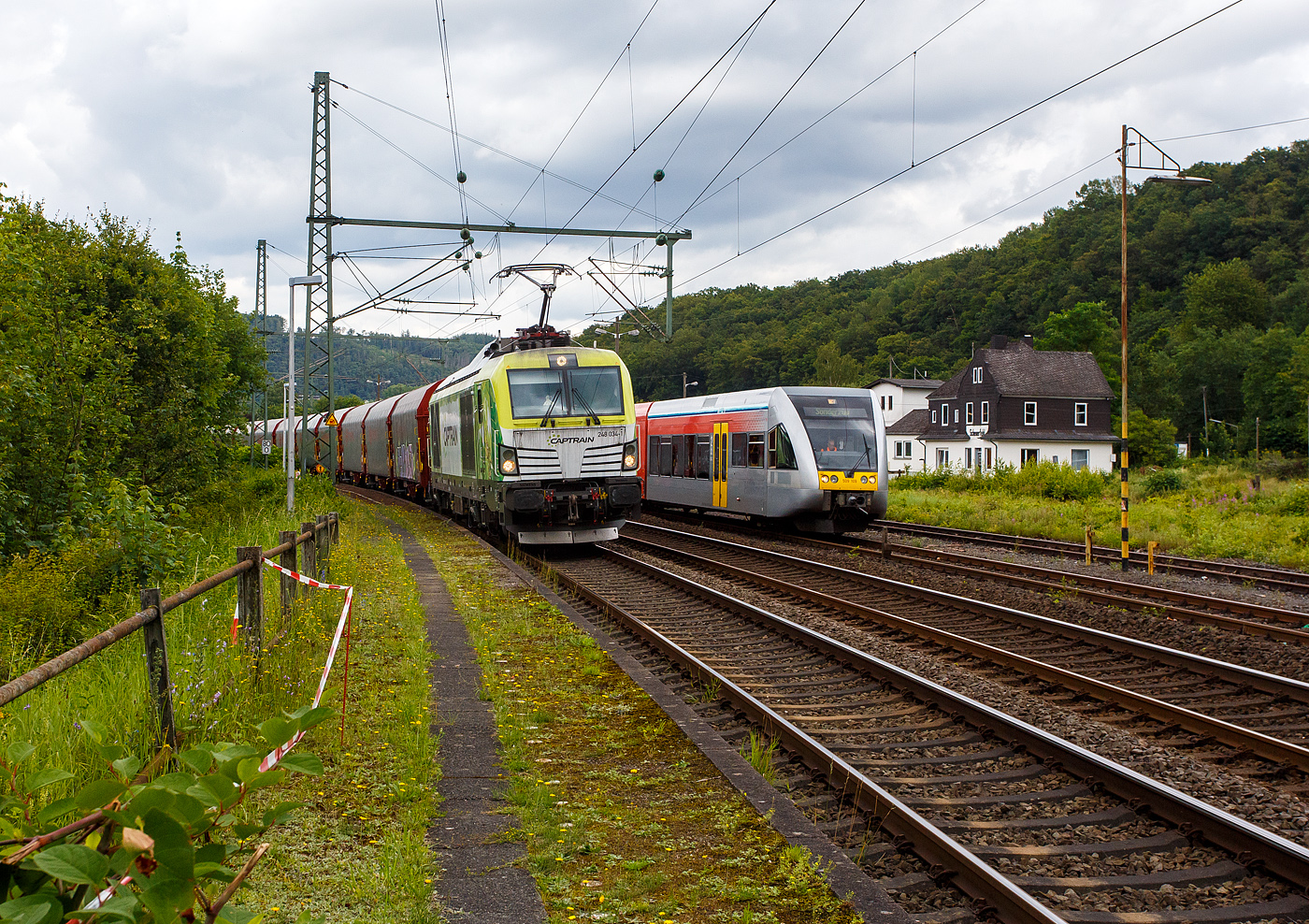 Die an die Dortmunder Eisenbahn GmbH (DE) vermietete SIEMENS Vectron Dual Mode 248 034-1  Phoenix  (90 80 2248 034-1 D-DE) der Captrain Deutschland GmbH fährt am 01 Juli 2024, mit einem Coilzug (Wagen der Gattung Shimmnis-ttu der Ermewa) durch Scheuerfeld/Sieg in Richtung Köln. Rechts wir der an die WEBA (Westerwaldbahn des Kreises Altenkirchen GmbH) vermietete Stadler GTW 2/6 VT 509 109 der HLB (Hessische Landesbahn GmbH), auf Rangierfahrt, überholt. 

Hinten rechts der ehem. Kleinbahnhof Scheuerfeld/Sieg der WEBA (Westerwaldbahn des Kreises Altenkirchen GmbH).