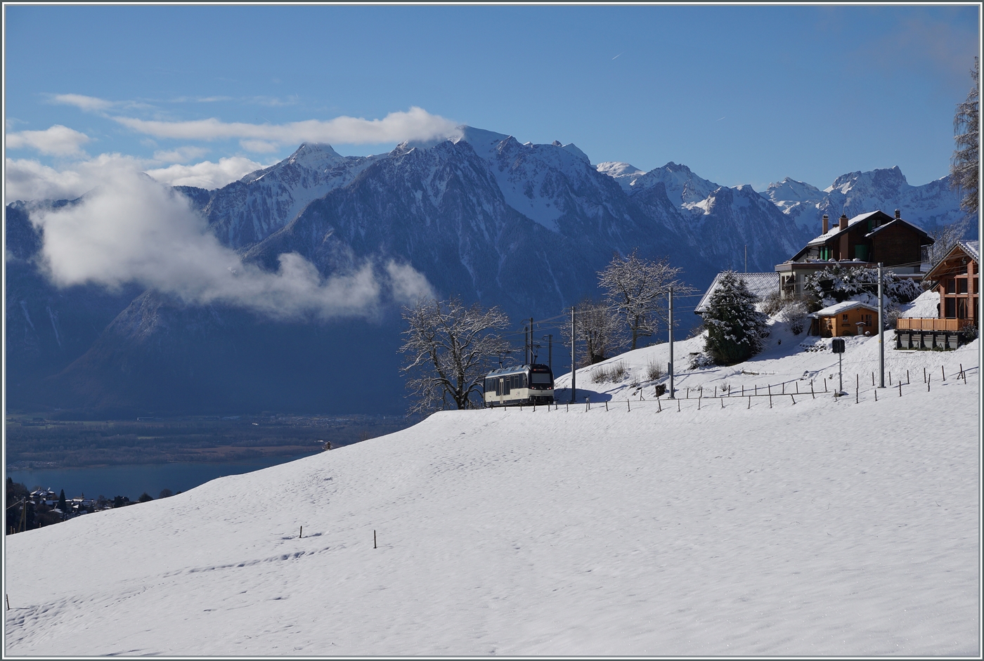 Die beiden MOB ABe 4/4 9304 und Be 4/4 9204 mit dem Regionalzug PE 2215 von Zweisimmen nach Montreux verlassen das Blickfeld bei Les Avants, zugleich gleitet der Blick auf die Savoyer Alpen und  links im Bild den Genfer See und die Rhone Ebene. 

3. Jan. 2025