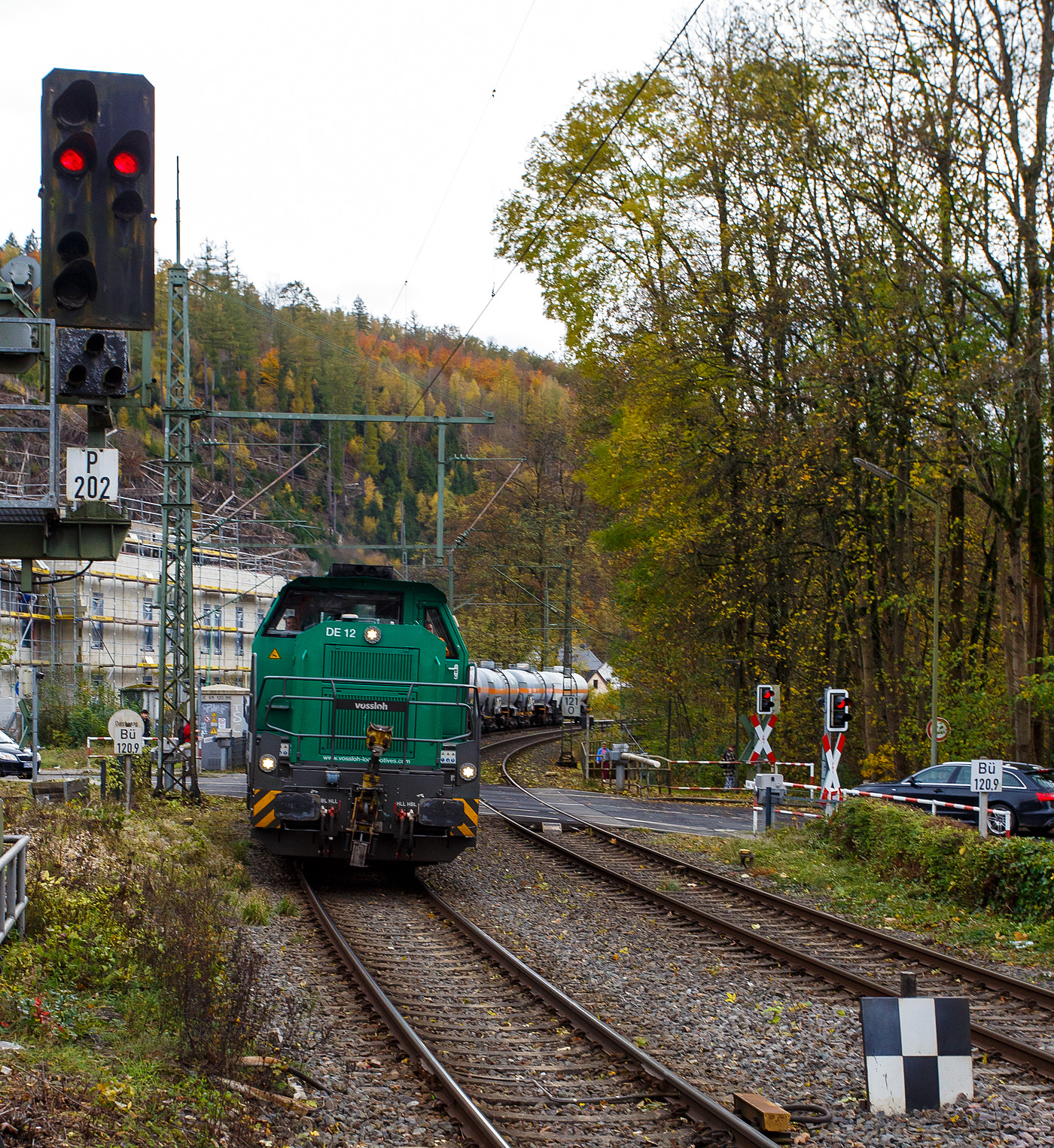 Die dieselelektrische Vossloh DE 12 / 4125 006-1 (92 80 4125 006-1 D-ISL) / Lok 11 der InfraServ Logistics GmbH (Frankfurt/M-Höchst) fährt am 29 Oktober 2025 mit einem Kesselwagenzug durch Kirchen (Sieg) in Richtung Siegen, vermutlich mit dem Ziel Frankfurt am Main-Höchst. Die Wagen waren laut Gefahrguttafelen (265/1017) mit Chor beladen. 

Die DE 12 wurde 2020 von Vossloh in Kiel unter der Fabriknummer 5402431 gebaut und an die InfraServ Logistics gefiefert.

Die InfraServ Logistics GmbH ist eine Tochtergesellschaft der Infraserv Höchst, diese ist Standortbetreiber des Industriepark Höchst in Frankfurt am Main sowie weiterer Standorte und ist eines der vielen Nachfolge-Unternehmen der aufgespaltenen Hoechst AG. Die InfraServ Logistics führt den werk sinternen Verkehr innerhalb des Industrieparks Höchst, aber auch den Güterverkehr auf dem Schienennetz der Deutschen Bahn im regionalen Bereich (Rhein-Main, Rhein-Necker und Rhein-Ruhr) durch. 

Die Vossloh DE 12 (BR 4125):
Die Vossloh DE 12 ist eine vierachsige dieselelektrische Mittelführerhaus-Lokomotive des Herstellers Vossloh, die für den schweren Rangier- und den leichten Streckendienst konzipiert ist. Von ihr wurden ab 2012 bis 2020 insgesamt z.Z. 13 Stück gebaut, somit ist sie weitaus erfolgreicher als das dieselhydraulische Einzelstück D 12 (4120 001-7). Die Lokomotiven besitzen im deutschen Fahrzeugeinstellungsregister die Nummer 92 80 4125 xxx-x. 

Entwicklung:
Als Weiterentwicklung der MaK DE 1002 bis MaK DE 1004 entstanden diese Lokomotiven 2012 bei Vossloh in Kiel. Der neue Lokomotivtyp wurde entsprechend den Anforderungen der TSI konstruiert und hergestellt. Somit ist ein europaweit länderübergreifender Einsatz vorbereitet.

Zusammen mit diesem Loktyp hat Vossloh auch eine dieselhydraulische Variante mit der Bezeichnung G 12 auf dem Markt gebracht, es blieb aber bei einem Einzelstück. Vorgestellt wurde die DE 12 erstmals auf der InnoTrans 2012. Wegen der Anpassungen an neue Bahnvorschriften wird der Typ als Vertreter der fünften Generation von Mak- bzw. Vossloh-Loks bezeichnet. Im neuen Bezeichnungsschema wird die Motorleistung (1.200 kW) geteilt durch 100 zum Ausdruck gebracht.

Technik:
Die Konstruktion der Baureihe DE12 ist für den schweren Rangier- und leichten Streckenbetrieb besonders nach den Gesichtspunkten Wirtschaftlichkeit und Ausfallsicherheit ausgelegt. Die bewährte Konstruktion der Vorgängermaschinen wurde nach den Grundsätzen neuester europäischer Normen überarbeitet. So sind der Lokrahmen sowie die Aufbauten der DE 12 nach der Crash-Norm EN 15227 ausgelegt und bieten somit noch mehr Sicherheit für das Lokpersonal bei Unfällen.

Als Antriebsmotor wurde der wassergekühlte MTU 90°-V8-Zylinder-Viertakt-Dieselmotor mit Common-Rail-Einspritzung, Abgasturbolader und Ladeluftkühlung vom Typ 8V 4000 R43L von der MTU (Motoren- und Turbinen-Union) Friedrichshafen GmbH verwendet. Dieser Motor ist nach der Abgasstufe EU Stage IIIA ausgelegt. Für noch größere Verringerung der Abgasemission kann zusätzlich noch ein Rußpartikelfilter verwendet werden. Die Kraftübertragung erfolgt dieselelektrisch mittels Drehstrom-Antriebstechnik. Die Radsätze sind mit Scheibenbremsen versehen.

TECHNISCHE DATEN:
Gebaute Anzahl: 13
Spurweite: 1.435 mm (Normalspur)
Achsfolge: Bo'Bo'
Länge über Puffer: 17.000 mm  
Größte Höhe:  4.310 mm  
Größte Breite:  3.080 mm
Drehzapfenabstand: 8.100 mm
Achsabstand im Drehgestell: 2.400 mm
Raddurchmesser: 1.000 mm (neu) / 920 mm (abgenutzt)
Dieselmotor: MTU 90°-V8-Zylinder-Viertakt-Dieselmotor mit Common-Rail-Einspritzung, Abgasturbolader und Ladeluftkühlung vom Typ 8V 4000 R43L
Dieselmotorleistung: 1.200 kW (1.630 PS) bei 1.800 U/min / 6.548 Nm
Motorhubraum: 38.1 l (Ø 170 mm Bohrung x 210 mm Hub)
Motorabmessungen: 2.000 x 1.565 x 1.860 mm
Motorgewicht: 6.270 kg (trocken)
Abgasvorschriften: EU/2004/26 Stufe IIIA/prepared for stage IIIB  
Leistungsübertragung: elektrisch
Stromrichter: IGBT
Traktionsmotoren: 4 Stück Drehstrom-Asynchronmotoren Drehstrom-Asynchron-Lokomotiv-Motoren (fremdbelüftet) vom Typ VEM DKLBZ 3510-4 (á 400 kW / 865 U/min). Übrigens die Marke „VEM“ ist eine der sehr wenigen ostdeutschen (DDR) Marken die die Wende und bis heute erfolgreich überstanden haben. Seit mehr als 130 Jahren entwickelt und fertigt VEM elektrische Maschinen für die Verkehrstechnik. Vermutlich sind auch der Generator und andere elektrischen Teile von VEM.
Höchstgeschwindigkeit: 120 km/h 
Anfahrzugkraft: 300 kN
Dauerzugkraft: 259 kN
Dienstgewicht: 90 t
Bremse: 2 x KE-GP-E mZ (D)
Max. elektrodynamische Bremsleistung: 1.450 kW
Kraftstoffvorrat: 3.000 bis 4.000 Liter
Kleinster befahrbarer Bogenradius: 55 m
Fährbootwinkel: 1° 30’
