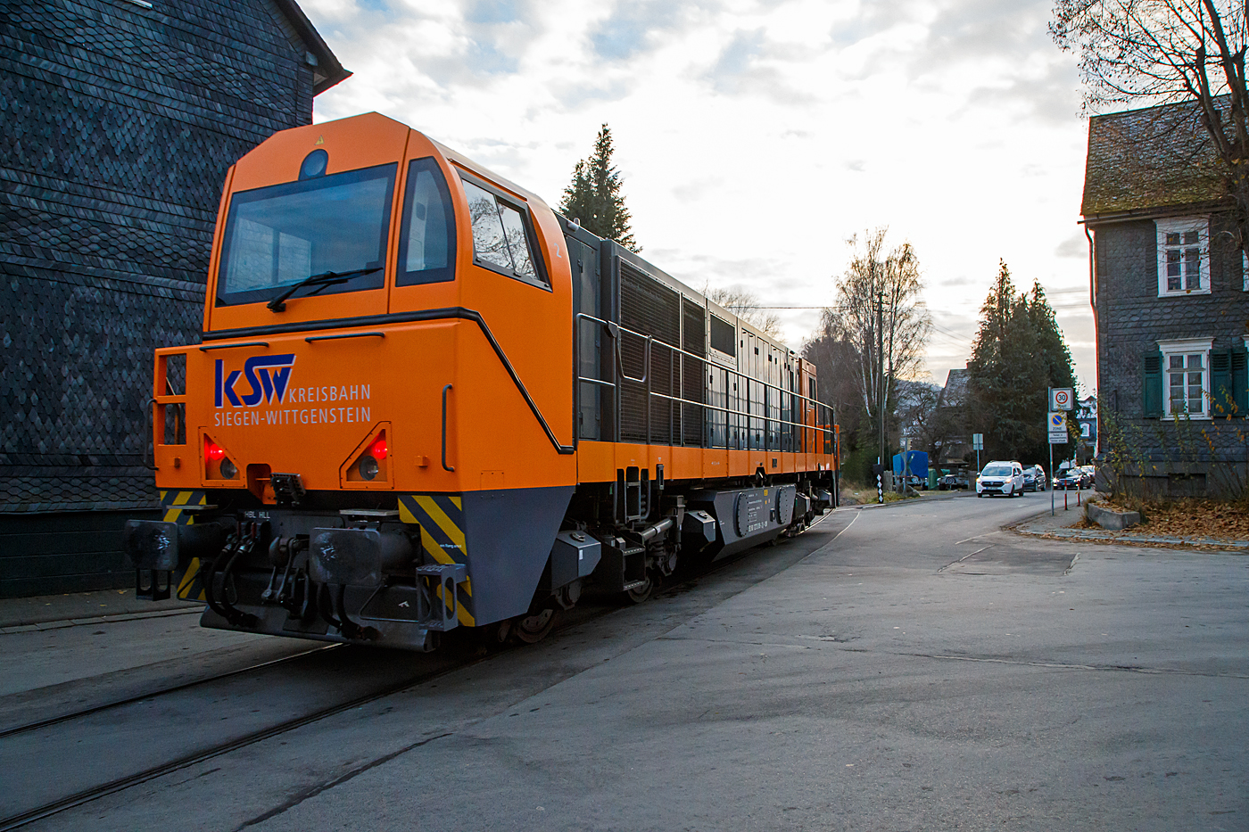 Die KSW 43 (92 80 1273 018-2 D-KSW), die asymmetrische Vossloh G 2000 BB der KSW (Kreisbahn Siegen-Wittgenstein) fährt am 14.12.2022 von Salchendorf kommend als Lz (Lokzug) durch Neunkirchen/Siegerland in Richtung Herdorf, hier überquert sie gerade die Kreuzung Bahnhofsstraße / Wiesenstraße. Hier ist sie mal kurz eine Straßenbahn. Die Strecke „Freien Grunder Eisenbahn“ (NE 447 / DB-Nr. 9275) von Herdorf nach Neunkirchen-Salchendorf (ehemals Pfannenberger Einigkeit) ist eine private Strecke (Infrastruktur) der Kreisbahn Siegen-Wittgenstein.

Nochmal einen lieben Gruß an das KSW Personal zurück. 
