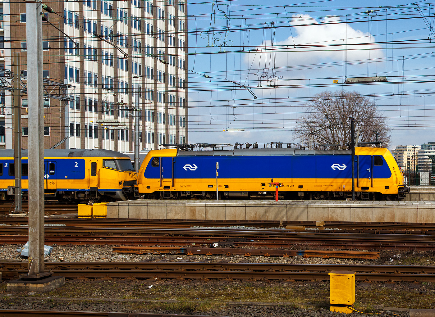 Die NS 186 119 (91 84 1186 119-1 NL-NS) erreicht am 31 Mrz 2018 mit einem IC (InterCity) den Bahnhof Amsterdam Centraal. Am Zugschluss war noch eine weitere 186er. 

Die Bombardier TRAXX F140 MS wurde 2007 von Bombardier in Kassel unter der Fabriknummer 34323 gebaut und an die ATC - Angel Trains Cargo, seit 2008 war sie dann an die NS Hispeed bzw. NS - Nederlandse Spoorwegen N.V. vermietet. Sie hat die Zulassungen fr Deutschland, sterreich, Belgien und die Niederlande. Aktuell (seit 2024) ist die Lok an die SNCB - Socit Nationale des Chemins de Fer Belges als 2869 vermietet und trgt die UiC Nummer 91 84 1186 119-1 NL-B. 

Die NS-Baureihe 186 wurden von Bombardier Transportation zwischen 2006 und 2014 gebaut. Die Lokomotiven werden zum Ziehen von Personenzgen verwendet, frher fr NS Hispeed und jetzt fr NS International. Sie sind eine Multi-Systems-Variante des TRAXX, einer Vierfach-Spannungslokomotive, die auf den meisten europischen Elektrifizierungssystemen arbeiten kann: 1,5/3,0 kV DC und 15/25 kV AC.

Die BR besteht aus zwei Chargen, die erste im Jahr 2008 eingefhrte Bauloks. Die zweite Charge wurde 2014 eingefhrt. Die ersten 12 Lokomotiven wurden 2005 von der Hochgeschwindigkeitsallianz (HSA) bei Alpha Trains bestellt. Die Bombardier Transportation in Kassel baute und ber Alpha Trains angemietet wurden. Diese kamen ab 2008/2009 auf den Verbindungen der HSL-Zuid zwischen Amsterdam und Breda zu Einsatz. Diese Zge haben eine Hchstgeschwindigkeit von 160 km/h. Diese Lokomotiven mit den Zgen sollte nur eine temporre Manahme sein, bis die Hochgeschwindigkeitstriebzge Fyra V250 (AnsaldoBreda V250) in Betrieb genommen wurden. Die V250 traten 2012 in Dienst, wurde aber Anfang 2013, wegen zahlreicher Mngel, auer Betrieb genommen und an den Hersteller zurckgegeben. Die italienische Trenitalia kaufte 2017 17 von den 19 Einheiten, die dort nun als ETR 700 im Einsatz sind. 

Aus diesem Grund waren die NS TRAXX-Lokomotiven noch bis 2024 im Einsatz.
