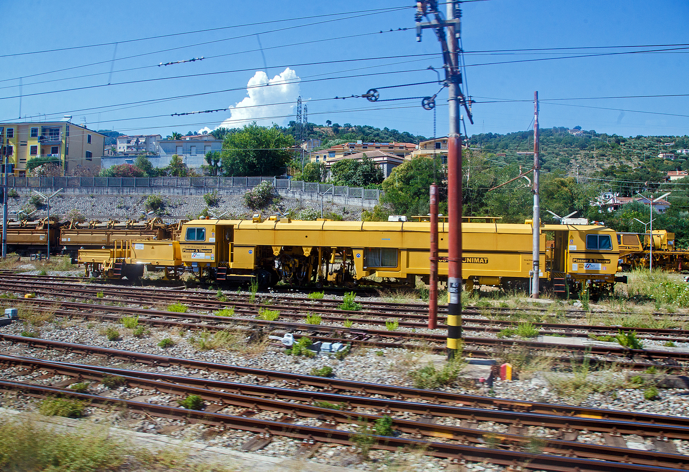 Die Plasser & Theurer Universalstopfmaschine 08 - 275 UNIMAT mit der UIC-Nr. IT-RFI 99 83 9422 012-8 der Rete Ferroviaria Italiana (RFI), geh. zur Gruppo Ferrovie dello Stato Italiane (zur Gruppe der Italienische Staatsbahnen) ist am 16.07.2022 beim Bahnhof Sapri (Kampanien) abgestellt. Aufnahme aus einem IC heraus.