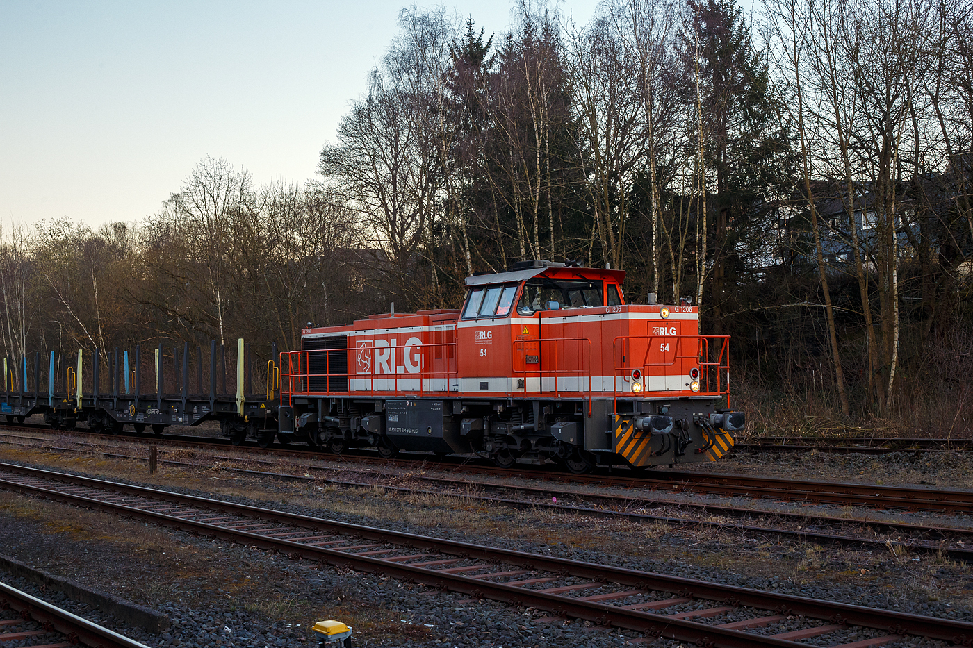 Die RLG 54 / 175 504-9 (92 80 1275 504-9 D-RLG) eine MaK G 1206 der RLG - Regionalverkehr Ruhr-Lippe GmbH (Soest), vermietet ans Schwesterunternehmen WLE - Westfälische Landes-Eisenbahn GmbH, kommt am 18. März 2025 auf ihrer Heimreise mit einem leeren Güterzug (Schwerlastwagen) von der Salzgitter Mannesmann Precision GmbH in Burbach-Holzhausen über die Hellertalbahn durch Herdorf. Hier im Bahnhof Herdorf hat sie, wegen der eingleisigen Strecke, erstmal Hp 0, bevor es in Richtung Betzdorf weitergeht.

Die G 1206 wurde 2008 von Vossloh in Kiel unter der Fabriknummer 5001638 gebaut. Sie war die erste wieder mit einen MTU gebaute G 1206. So hat sie einen wassergekühlten V12-Zylinder-Dieselmotor mit Abgasturbolader und Ladeluftkühlung vom Typ MTU mit einer Leistung von 1.500 kW (bei 1.800 U/min).

TECHNISCHE DATEN der G 1206:
Spurweite: 1.435 mm
Antriebart:  dieselhydraulisch
Achsfolge: B'B' 
Länge über Puffer: 14.700 mm
Drehzapfenabstand: 7.200 mm
Achsabstand im Drehgestell: 2.400 mm
größte Breite: 3.080 mm
Höhe über Schienenoberkante: 4.220 mm
Raddurchmesser neu: 1.000 mm
Motor: MTU 12 Zylinder 4-Takt Dieselmotor mit Abgasturbolader und Ladeluftkühlung vom Typ 12V 4000 R41
Leistung: 1.500 kW bei1.800 U/min
Strömungsgetriebe: Voith L 5r4 zseU2
Anfahrzugkraft: 267 kN
Höchstgeschwindigkeit: 100 km/h
kleinster befahrbarer Gleisbogen:	60 m
Dienstgewicht: 88 t
Kraftstoffvorrat: 3.150 l