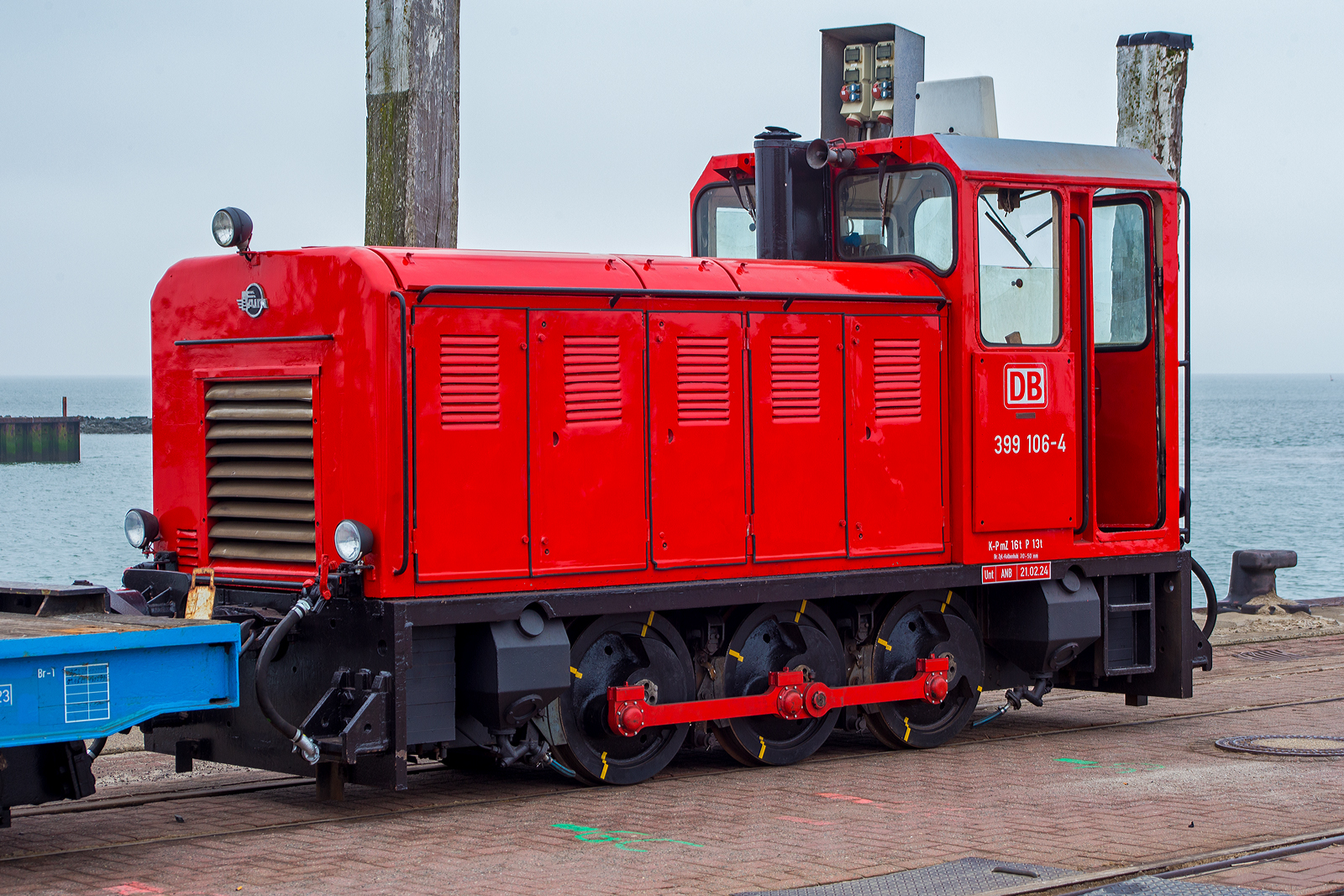 Die schmalspurige Diesellok 399 106-4 (98 80 3399 106-4 D-DB), eine der DB Fernverkehr AG bzw. der Wangerooger Inselbahn / SIW - Schifffahrt und Inselbahn Wangerooge steht am 13 März 2024, nun mit einem leeren Güterzug bestehend aus vierachsiger schmalspuriger Flachwagen DB 630xx, am Westanleger der friesischen Insel Wangerooge. Zuvor war der Güterzug beladen und wurde bereits mittels (20 t) Schwerlastgabelstapler entladen, bevor er wieder beladen wird, dies dauert aber gerade noch etwas, da gerade auch die Personenfähre MS Harlingerland angekommen ist.

Noch vor der Gründung der DB AG beschaffte die Deutsche Bundesbahn im Jahr 1992 zwei dreiachsige Kleinloks des rumänischen Typs Faur L18H vom ehemaligen Mansfeld-Kombinat für den Einsatz auf der Inselbahn Wangerooge. Sie sollten zunächst die Altbaulokomotiven der Baureihe 329 unterstützen, konnten aber die in sie gesetzten Erwartungen nicht erfüllen. Sie werden daher bis heute meist für kurze Güterzüge und als Reserve für die Personenzüge vorgehalten, wenn die Maschinen 399 107 und 399 108 nicht zur Verfügung stehen.

Die meterspurige Lok wurde 1990 vom rumänischen Hersteller FAUR S.A.(bis 1989 Faur Lokomotivwerke 23. August) in Bukarest unter der Fabriknummer 25666 gebaut und im April 1990 an das MKWP - VEB Mansfeld-Kombinat  Wilhelm Pieck  geliefert, wo sie kurz bei der zum Kombinat gehörenden meterspurige Schlackenbahn der August-Bebel-Hütte, ehemals bis 1951 Kochhütte, (eine Kupferhütte) in Helbra im Einsatz war. Am 10. September 1990 erfolgte der letzte Ofenabstich auf der Kochhütte. Die Gebäude und Betriebsanlagen wurden in den Folgejahren vollständig zurückgebaut, heute befindet sich hier ein Gewerbegebiet. So wurde bereits im November 1992 die Lok, wie eine weitere (399 105-6), an die DB - Deutsche Bundesbahn für die Wangerooger Inselbahn verkauft. Bevor sie dort zum Einsatz kam erfolgte im BW Wangerooge im Juli 1993 ein Umbau bzw. Anpassung an die EBO-Richtlinien und DB-Standards.

Insgesamt wurden zehn Diesellokomotiven der Baureihe L18H vom rumänischen Fahrzeug- und Maschinenherstellers FAUR zwischen 1983 und 1990 für verschiedene schmalspurige Wald- und Industriebahnen in Osteuropa gebaut. Es handelt sich um dreiachsige, stangengekuppelte Maschinen mit einem einseitigem Motorvorbau und Endführerstand sowie Antrieb in Z-Anordnung. Als Antrieb dient ein direkt angeflanschter Drehmomentwandler mit Lastschaltgetriebe und Achsgetriebe auf dem ersten Radsatz.

TECHNISCHE DATEN:
Spurweite: 	1.000 mm (Meterspur)
Achsformel: C
Länge über Puffer: 5250 mm
Höhe: 2.800 mm
Breite: 1.800 mm
Achsabstand: 2 x 900 = 1.800 mm
Treibraddurchmesser: 	750 mm
Kleinster befahrbarer Gleisbogen: R 20 m
Leergewicht: 16,0 t
Höchstgeschwindigkeit: 	28 km/h
Installierte Leistung: 132 kW
Motorentyp:  MAN (Lizenzbau) D2156 HM N8
Motorbauart: 6-Zylinder-Reihenmotor mit 10.350 cm³ Hubraum
Nenndrehzahl: 1.800/min
Leistungsübertragung: hydrodynamisch und mechanisch
Bremse: Druckluft
Lokbremse: Druckluft, indirekt
Kupplungstyp: Balancierhebel- bzw. Ausgleichkupplung (zp2)
