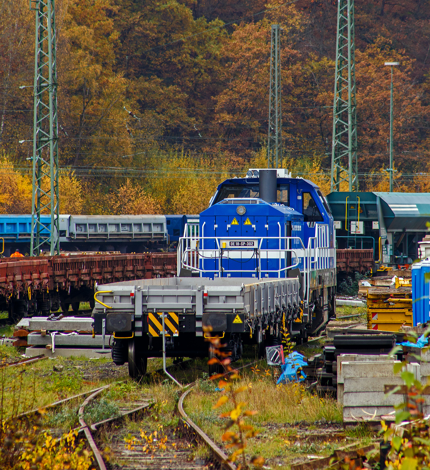 Die sehr neue SPITZKE DE18-SP-302 / 4185 302-1 (92 80 4185 302-1 D-SLG) eine dieselelektrische Vossloh DE 18 der SPITZKE SE steht am 08 November 2025 hinter einem Res-Wagen im Rbf Betzdorf/Sieg. 

Die DE18 wurde 2025 von der Vossloh Rolling Stock GmbH in Kiel unter der Fabriknummer 5502655 gebaut und am 14.08.2025 an die SPITZKE SE, Großbeeren ausgeliefert (Tag der Überführung).

Die Diesellokomotive der Baureihe DE 18 ist insbesondere für den schweren Rangier- und Streckenbetrieb mit hoher Zugkraft geeignet. Sie gilt als aktuell leistungsstärkste Mittelführerhauslokomotive auf dem europäischen Markt. Die DE 18 ist für den Rangierbetrieb mit einer Funkfernsteuerung ausgerüstet und ist für bis zu drei Loks mehrfachtraktionsfähig. Durch Energiesparmodus und Start-Stopp-System reduziert sie Schadstoffausstoß und spart Treibstoff ein, zudem besitzt sie einen Rußpartikelfilter. Zusätzlich lässt sich der Kraftstoffverbrauch durch ein effizientes Motormanagement und einer Begrenzung der Motorleistung, wenn nicht die Maximalleistung benötigt wird, reduzieren. Der 1.800 kW starke MTU Dieselmotor wird durch ein Batteriepaket ergänzt, das einen bis zu einstündigen emissionsfreien Rangierbetrieb gewährleistet und Fahrten durch Null-Emissions-Bereiche etwa in Tunneln, Werkhallen oder Bahnhöfen, ermöglicht.

Die Lok hat eine Anfahrzugkraft von 300 kN und eine Dauerzugkraft von 230 kN bei 24.2 km/h. Höchstgeschwindigkeit beträgt 120 km/h, die kleinste Dauerfahrgeschwindigkeit 3 km/h,
