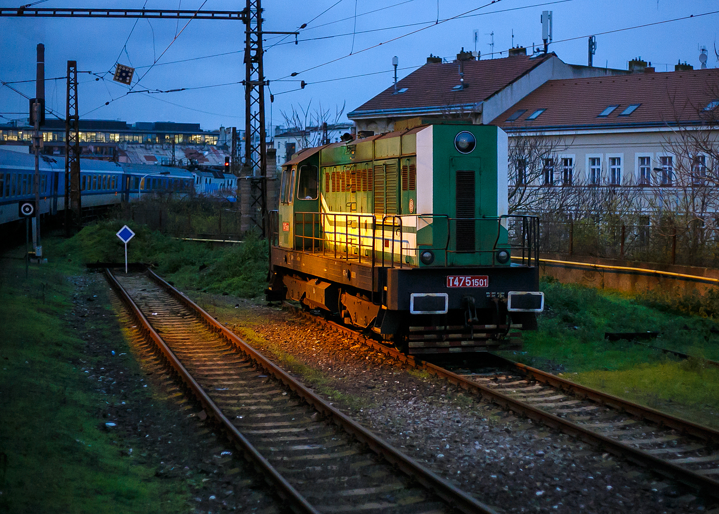 Die T 475.1501, alias 744 501-8 (CZ- RLK 92 54 2 744 501-8) der Retrolok s.r.o. (Prag) ist am 22.11.2022 beim Bahnhof Praha-Smíchov (tschechisch: Stanice Praha-Smíchov) abgestellt (aufgenommen aus einem alex-Zug). Der  Schmetterling  ist eine dieselelektrische Lokomotive, und wurde 1970 von ČKD in Prag (Českomoravská-Kolben-Daněk) als Prototyp gebaut. 

Die Lokomotive der Baureihe 744.5 (bis 1987 die Baureihen T 475.15 und T 476.0) ist eine vierachsige dieselelektrische Lokomotive, die 1970 in zwei Prototypen von der Lokomotivfabrik ČKD in Prag hergestellt wurde. Sie ist ein Entwicklungsvorläufer der späteren Serienlokomotiven der Baureihen 740 und 742 (bzw. 743). Zwei Jahre später entstand ein dritter Prototyp jedoch mit einem Achtzylindermotor K 8 S 230 DR.

Im Rahmen der Modernisierung des ČKD-Produktionsprogramms Ende der 1960er Jahre wurde die Entwicklung eines völlig neuen Typs von Reihensechszylindern mit einer Bohrung von 230 mm, im Zweigwerk Smíchov der ČKD Naftové motory (sog. Werk Wilhelm Pieck), begonnen. Dieser wurde als K 6 S 230 DR bezeichnet. Der geplante Einsatz dieses Motors sollte sowohl in Gleis- als auch in Rangierlokomotiven erfolgen. Um den neuen Motor in der Praxis testen zu können und gegebenenfalls konstruktive Mängel auszubessern, wurden 1970 zwei Prototypen gefertigt, die als Baureihe T 475.15 (heute 744.5) bezeichnet wurden. Bei jedem von ihnen wurde der Motor zum Testen auf eine andere Leistung (zwischen 600 bis 883 kW) eingestellt. Gleichzeitig wurde dieser Typ erstmals verwendet, um den Rahmen mit Gummi-Metall-Verbindungen am Fahrgestell zu befestigen, was später zum Standard wurde. Beide Prototypen wurden zunächst im ŽZO in Cerhenice getestet und dann an die ČSD zur Erprobung in den Schnellzügen von Prag nach Babín vermietet. Neben diesen beiden Prototypen mit dem Motor K 6 S 230 DR wurde 1972 ein dritter produziert, der als Baureihe T 476.0 bezeichnet und mit einem stärkeren Achtzylinder K 8 S 230 DR ähnlichen Konzepts ausgestattet und verglichen wurde zu schwächeren Maschinen.

Die Erprobung war 1973 abgeschlossen, und da die Produktionsvorbereitung der neuen Baureihe T 448.0 (740) bereits im Endstadium war, wurden beide Sechszylinder-Maschinen zum Verkauf angeboten. Das erste davon wurde von AZNP in Mladá Boleslav (heute Škoda Auto) gekauft und war hier bis 2017 in Betrieb, bevor sie von RETROLOK s.r.o. (Prag) ersteigert wurde. Am zweiten zeigte das Zementwerk in Hranice in Mähren Interesse. Später ging es in den Besitz des Dienstleistungsunternehmens Lokotrans über und wird heute von BF Logistics betrieben. Die Achtzylindermaschine hatte nicht so viel Glück - zwischen 1974 und 1978 wurde sie abwechselnd an die ČSD vermietet und in eigener Regie getestet, in den achtziger Jahren wurde sie in den Hütten in Kladno eingesetzt und 1988 wurde sie aufgrund ihrer endgültig eingestellt und verschrottet. 

TECHNISCHE DATEN der T 475.1501:
ČKD-Bezeichnung: 1435 Bo´Bo´ 1200
Spurweite: 1.435 mm
Achsfolge: Bo'Bo'
Länge über Puffer 13 540 mm
Dieselmotor: 6-Zylinder-Viertakt-Reihen- Dieselmotor mit Direkt-Einspritzung und Turbolader vom Typ ČKD  K 6 S 230 DR
Motorhubraum: 64,75 Liter (Zylinder-Ø 230 mm / Kolbenhub 260 mm)
Kompressionsverhältnis: 12,5 : 1
Nenndrehzahl: 400 – 1.250 U/min
Motorgewicht (ohne Generator): 7.700 kg
Leistung: 846 kW (1.150 PS)
Leistungsübertragung: dieselelektrisch
Höchstgeschwindigkeit: 140 km/h
Dienstgewicht: 60 t
Kleinster bef. Halbmesser: R 80 m
Anfahrzugkraft: 180 kN

Quellen: RETROLOK s.r.o., Wikipedia (CZ), zos-vrutky.sk