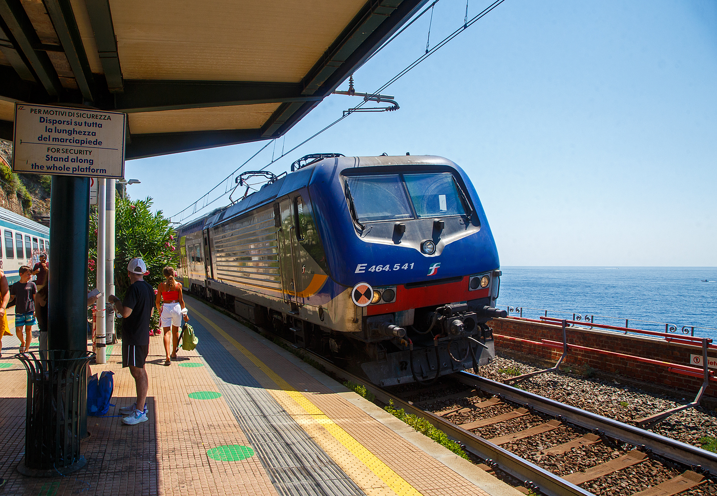 Die Trenitalia E.464.541 erreicht mit dem Cinque Terre Express (Regionale La Spezia Centrale – Levanto) am 21.07.2022 den Cinque Terre Bahnhof Corniglia.

Corniglia hat zwar diesen Bahnhof an der Bahnstrecke Pisa–Genua, aber Corniglia ist das einzige Dorf der Cinque Terre (5 Dörfer) das nicht direkt am Meer und so ist man nicht direkt vom Bahnhof im Ort. Sondern der Ort ist auf einem Bergvorsprung in etwa 100 m Höhe, umgeben von drei großen Weinbergflächen und einer steilen Klippe zum Meer. So müsste man hier vom viel tiefer gelegenen Bahnhof aus über die Lardarina, eine lange Ziegelsteintreppe, laufen. 

Wer wie wir aber die Cinque Terre Card Treno (Zugkarte) hat, könnte sich aber auch mit den Minibusen des Cinque Terre Parks (im Preis der Cinque Terre Treno Card eingeschlossen) die über 1 km lange Strecke hinauf fahren lassen. Aber die Busse waren uns einfach zu voll. Mit der Karte hat man auch Zutritt zu den beiden gebührenpflichtigen Wanderwegen des Cinque Terre Parks.
