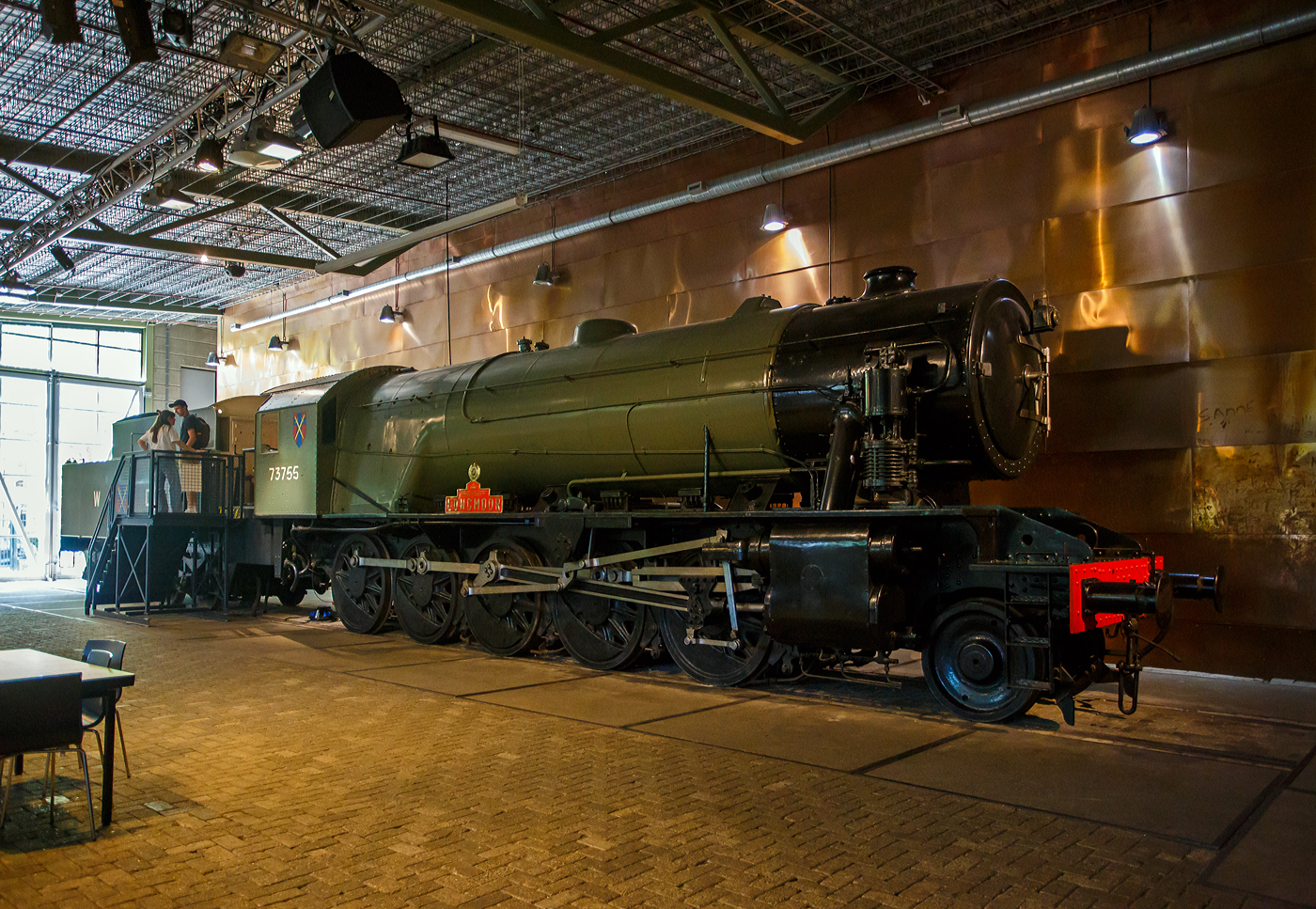 Die WD 73755 „Longmoor“, spätere NS 5085 (NS-Baureihe 5000), eine Dampflokomotive vom Typ WD Austerität 2-10-0 / LMR 600 Gordon, gekuppelt mit einem vierachsigen Tender, am 29 April 2025 im Het Spoorwegmuseum (bis 2005 NSM - Nederlands Spoorwegmuseum / Niederländischen Eisenbahnmuseum) in Utrecht im ehemaligen Bahnhof Maliebaan.  

Die 73755 wurde 1945 unter der NBL-Fabriknummer 25601 gebaut und als WD 3755 an die British War Department (WD) fürs Longmoor Military Railway Corps geliefert, später sie in WD 73755 umgezeichnet. Sie eine von 150 WD-Austerität 2-10-0, die alle von der North British Locomotive Company in Glasgow (GB) gebaut wurden. Sie war die 1000te britische Dampflokomotive, die zur Unterstützung der britischen Armee aufs europäische Festland nach Frankreich verschifft wurde. Nach ihren ereignisreichen Reisen mit den Alliierten wurden 60 Lokomotiven von der NS 1946 geleast. Weitere 43 kamen im Juni hinzu. 1947 gingen sie in den Besitz der NS über, die die Lokomotive übernahm, die diese als Baureihe/Serie 5000 einreihte (NS 5001 bis 5103). So wurde aus dieser die NS 5085. Die letzten Lokomotiven dieser Baureihe wurden 1952 außer Dienst gestellt.

Die NS 5000 war eine Reihe von Dampflokomotiven der NS - Nederlandse Spoorwegen (Niederländischen Staatsbahnen, heute Niederländische Eisenbahnen AG), die vom British War Department (WD) übernommen wurden. Sie hatten den Spitznamen „Grote Jeep“ (Großer Jeep).

Die Lokomotiven mit der Radanordnung 1'E (2-10-0) wurden zwischen 1943 und 1945 von der North British Locomotive Company in Glasgow für das britische Kriegsministerium gebaut, um Waren zur britischen Armee während des Krieges gegen Nazi-Deutschland im westeuropäischen Festland zu transportieren. 

Die britische Armee gründete ein separates Eisenbahnkorps, das Longmoor Military Railway Corps. Dieses Regiment war für den Betrieb von Militärzügen in befreiten Gebieten verantwortlich. Während des Zweiten Weltkriegs gab das britische Kriegsministerium eine große Anzahl dieser Lokomotiven in Auftrag, die die Invasionsarmee begleiteten. Zwei Serien wurden von der North British Locomotive Company gebaut. Die erste Lieferung von 100 Lokomotiven wurde 1943/1944 eingeführt, die zweite Lieferung von 50 Lokomotiven 1945. Ihre WD-Nummern waren 3650–3749 (später 73650–73749) und 73750–73799. Zunächst wurden sie in England eingesetzt, waren aber aufgrund ihrer Länge weniger geeignet. Die meisten wurden erst nach dem D-Day bei der britischen Armee in Frankreich in Dienst gestellt. Nach dem Krieg war der Großteil der Loks in den Niederlanden.

Die Loks mit der geringen Achslast von 13,7 Tonnen machte sie sehr geeignet für den Betrieb auf provisorischen oder reparierten Bahnstrecken. Während der britischen Besatzung wurden mehrere Lokomotiven in Gebieten südlich der Niederlande eingesetzt. Um den Oktober 1945 wurden die Loks außer Betrieb genommen und eingelagert.

Um den Eisenbahnverkehr nach der deutschen Kapitulation im Mai 1945 in Gang zu bringen, wurde die Klasse anstelle von niederländischen heimischen Dampfloks eingesetzt, die während des Krieges zerstört oder beschädigt wurden. Anfang 1946 wurde beschlossen, dass die NS etwa sechzig Lokomotiven als NS 5001-5060 für den Zugdienst anschaffen würde. Später wurde diese Zahl um weitere 43 Lokomotiven ergänzt, so dass die Baureihe NS 5001-5103 entstand.

Die NS senkte den Dampfdruck bald von 15,8 kg/cm² 225 psi auf 12 kg/cm² (170 psi) und machte die Schornsteine länger, um den Rauch aus dem Sichtfeld des Lokführers zu bringen. Zudem wurde das Führerhaus umgebaut und eine verbesserte Tenderkupplung angebaut. Diese Lokomotiven wurden bereits zwischen 1948 und 1952 wieder aus dem Dienst genommen. Die NS setzte schon früh auf Diesel- und Elektroantrieb. Da wurden für die Deutsche Bundesbahn noch neue Dampfloks gebaut, die letzte 1959 mit der bei Jung (Jungenthal) mit der Fabriknummer 13113 die 23 105. 

An die 1.000th gebaute Lokomotive, die nach Kontinentaleuropa verschifft wurde, wird erinnert. Diese Lokomotive mit dem Namen  Longmoor   wurde im Niederländischen Eisenbahnmuseum in Utrecht erhalten und in die Kriegsabteilung mit der Nummer WD 73755 zurückversetzt. Als Werbung erhielt sie den Namen Longmoor.

Das Longmoor Military Railway Corps wurde 1968 aufgelöst.

TECHNISCHE DATEN:
Hersteller: North British Locomotive Company, Glasgow (GB)
Anzahl bei der NS:103
Nummerierung: NS 5001-5103
Außer Dienststellung:  1948-1952
Spurweite: 1.435 mm (Normalspur)
Achsfolge: 1'E (engl. 2-10-0) 
Länge über Puffer: 20.580 mm (Lok 12.600 mm + Tender 7.980 mm)
Treibraddurchmesser: 1.435 mm (neu)
Laufraddurchmesser: 838 mm (neu)
Höchstgeschwindigkeit: 65 km/h (40 mph)
Gesamtheizfläche: 215,3 m²
max. Dampfdruck: 15,8 kg/cm² (225 psi) später 12 kg/cm² (170 psi)
Anzahl der Zylinder: 2 außenliegend (Ø 457 mm x 660 mm Hub)
Steuerung: Walschaerts (entspr. Heusinger)
Dienstgewicht: Lok 79,6 und Tender 56,4 t = 136 t
Anfahrzugkraft: 152,20 kN, später mit 12 bar Dampfdruck 95.12 kN
Wasservorrat: 22,7 m³
Kohlevorrat: 9,1 t

Quellen: Het Spoorwegmuseum, nmld.nl und Wikipedia (NL und GB)
Stand/Überarbeitung: September 2025

