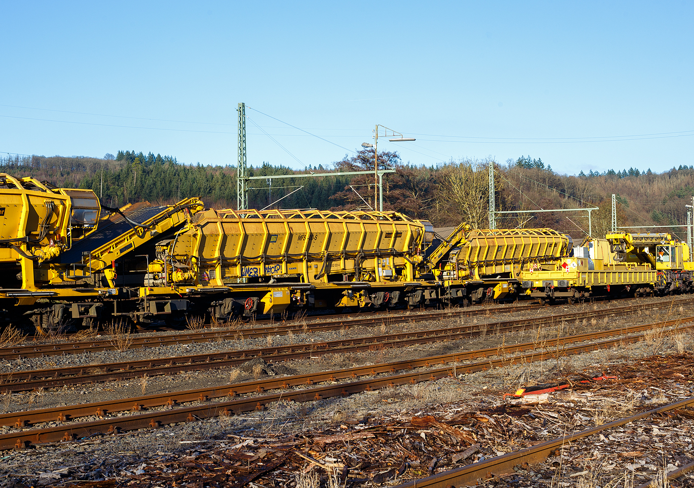 Drei Plasser & Theurer Materialfrder- und Siloeinheiten (MFS 100) der sterreichischen Gleisbaufirme PORR AG (Wien) sind, mit einem Schutzwagen, am 26 Dezember 2024, in Scheuerfeld/Sieg abgestellt. Hier im Vordergrund die P&T Materialfrder- und Siloeinheit MFS 100 S (mit Endladung nach unten ins Gleis mglich) 99 81 9352 031-4 A-PTU.

TECHNISCHE DATEN:
Hersteller: Plasser & Theurer, Linz an der Donau (sterreich)
Spurweite: 1.435 mm
Lnge ber Puffer: 22.900 mm
Achsanzahl: 8 (in 2 Doppel-Drehgestellen)
Drehzapfenabstand der Doppeldrehgestelle: 15.100 mm
Drehzapfenabstand der Einzeldrehgestelle: 3.900 mm Achsabstand der Einzeldrehgestelle: 1.500 mm
Motorleistung: 165 kW (wassergekhlter Deutz BF6M 1013 C Motor fr Bandantrieb)
Eigengewicht: 64 t
Nutzlast: 80 t ab D4
Fahrgeschwindigkeit in Schleppfahrt leer, max.: 120 km/h
Fahrgeschwindigkeit in Schleppfahrt beladen, max.:100 km/h
Fassungsvermgen: 68 m
Frderleistung (materialabhngig), max.: 700 – 800 m/h
Entladezeit: ca. 5 min