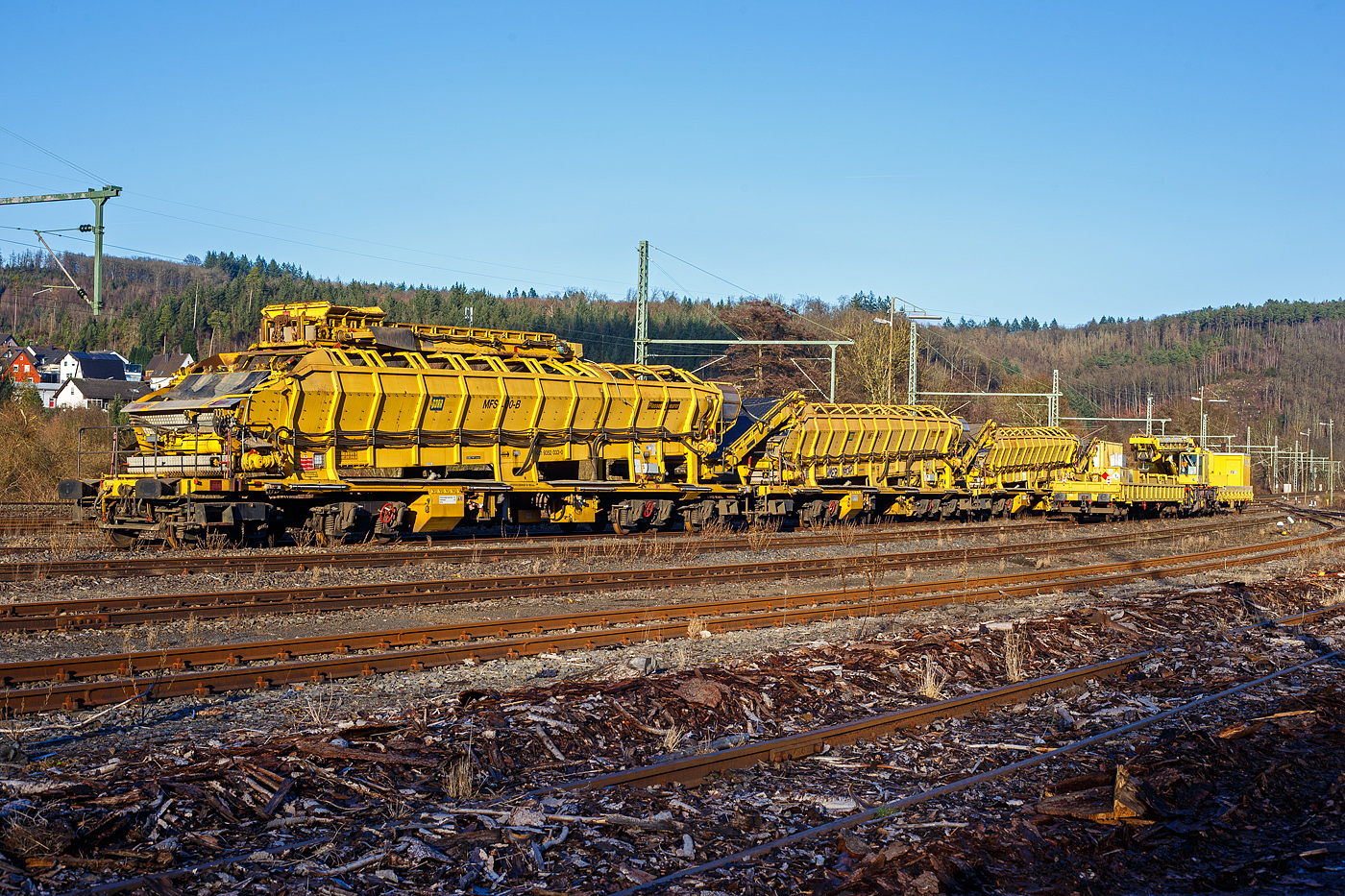 Drei Plasser & Theurer Materialfrder- und Siloeinheiten (MFS 100) der sterreichischen Gleisbaufirme PORR AG (Wien) sind, mit einem Schutzwagen, am 26 Dezember 2024, in Scheuerfeld/Sieg abgestellt. Davor auf dem Gleis steht der GOTTWALD Gleisbauschienenkran GS 80.08 T, Schweres Nebenfahrzeug Nr. 99 80 9419 007-6 D-Krebs der Krebs Gleisbau GmbH & Co. KG, Bingen am Rhein (Tochterunternehmen der schweizerischen KREBS Gleisbau AG, Bern), in Transportstellung mit dem Gegenlastwagen 37 80 3940 046-0 D-KREBS der Gattung Res und dem Schutzwagen auslegerseitig 99 80 9383 002-9 D-Krebs..

Hier im Vordergrund (links) die P&T Materialfrder- und Siloeinheit MFS 100 B mit integrierter Beladestation (in Transportstellungen oben auf dem MSF) 99 81 9352 033-0 A-PTU.

TECHNISCHE DATEN:
Hersteller: Plasser & Theurer, Linz an der Donau (sterreich)
Spurweite: 1.435 mm
Lnge ber Puffer: 22.900 mm
Achsanzahl: 8 (in 2 Doppel-Drehgestellen)
Drehzapfenabstand der Doppeldrehgestelle: 15.100 mm
Drehzapfenabstand der Einzeldrehgestelle: 3.900 mm Achsabstand der Einzeldrehgestelle: 1.500 mm
Motorleistung: 165 kW (wassergekhlter Deutz BF6M 1013 C Motor fr Bandantrieb)
Eigengewicht: 67 t
Nutzlast: 77 t ab D4
Fahrgeschwindigkeit in Schleppfahrt leer, max.: 120 km/h
Fahrgeschwindigkeit in Schleppfahrt beladen, max.:100 km/h
Fassungsvermgen: 68 m
Frderleistung (materialabhngig), max.: 700 – 800 m/h
Entladezeit: ca. 5 min
Besonderheit: mit integrierter Beladestation
