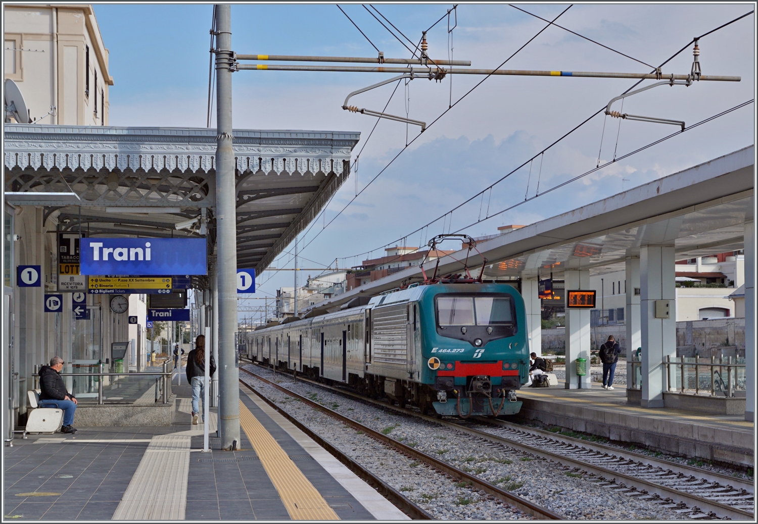 Ein FS Trenitalia Regionalzug in Richtung Bari hält in Trani. Trotz der vielen neuen Fahrzeuge sind hin und wieder weiterhin älter Züge im Einsatz, wie dieser FS Tpy 73 Niederflurzug (Carrozza vicinale a piano ribassato) in XMPR Lackierung mit einem npBD an der Spitze und vier nB Wagen sowie der schiebenden FS Trenitalia E 464 273.

20. April 2023