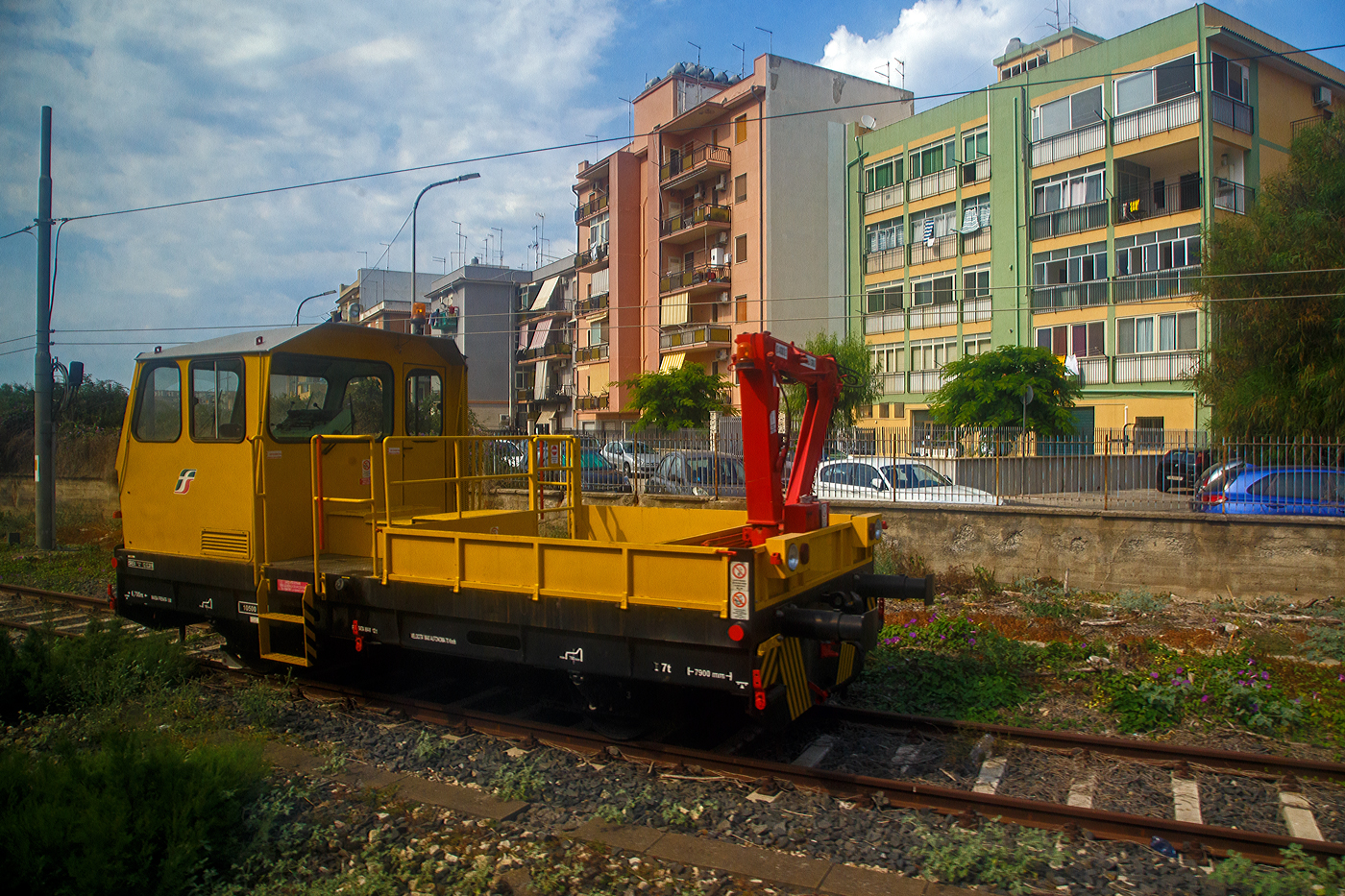 Ein Italienisches Gleisarbeitsfahrzeug mit hydraulischen Benelli Kran B.4000/2 (Autocarrello con gru vom Typ MERMEC MM 87) der RFI - Rete Ferroviaria Italiana (FS Eisenbahninfrastruktur) steht am 19 Juli 2022 bei Augusta (Sizilien). Da die Aufnahme aus einem Zug ist, leider mit Spieglungen. 