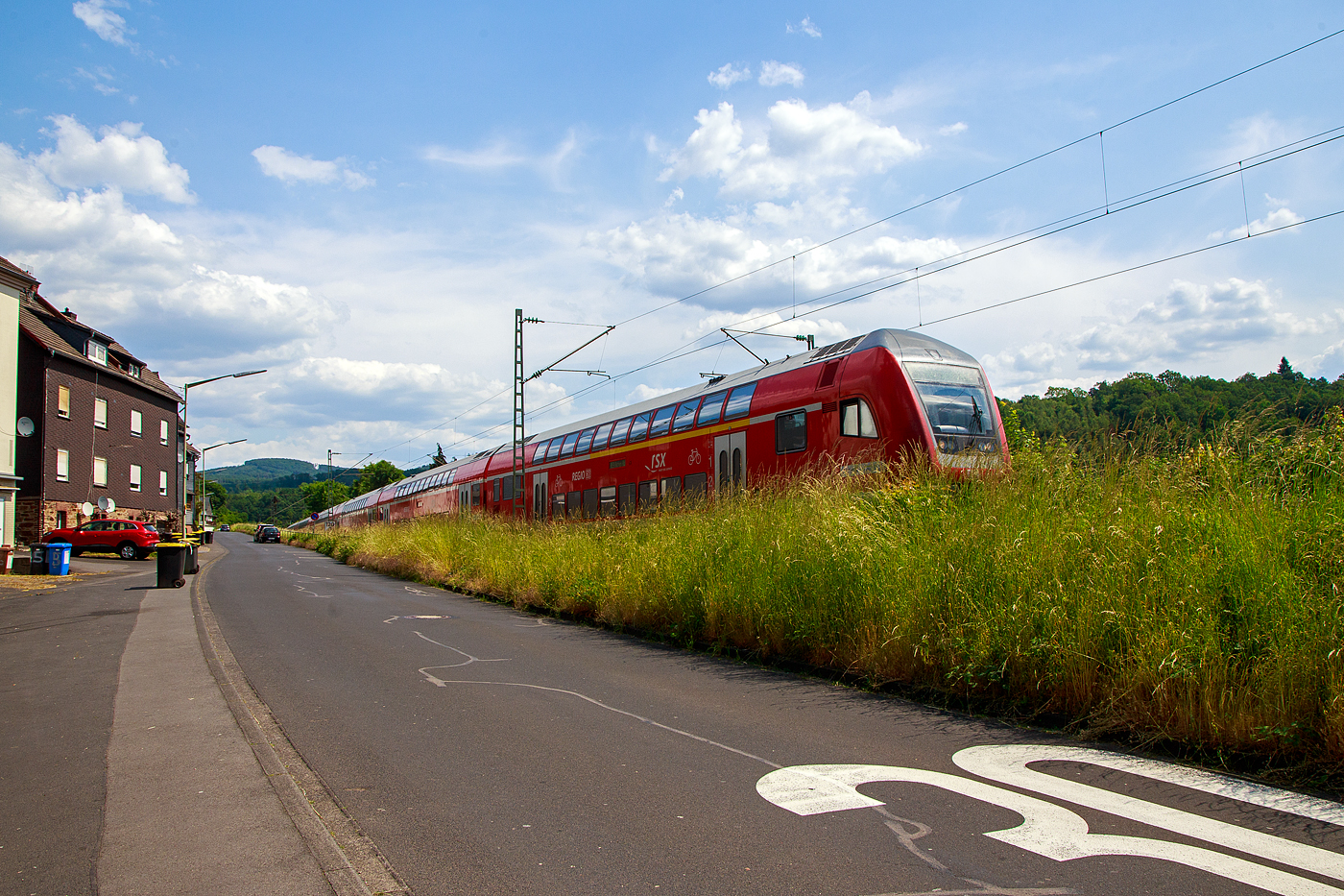 Etwas verdeckt hinter den hohen Gräsern fährt am 06.06.2023 der RE 9 rsx - Rhein-Sieg-Express (Siegen – Köln – Aachen) Steuerwagen voraus durch Kirchen an der Sieg und erreicht bald den Bahnhof Kirchen. Der Zug bestand aus sechs Doppelstock-Wagen, die Schublok war die 146 006-2 der DB Regio NRW.