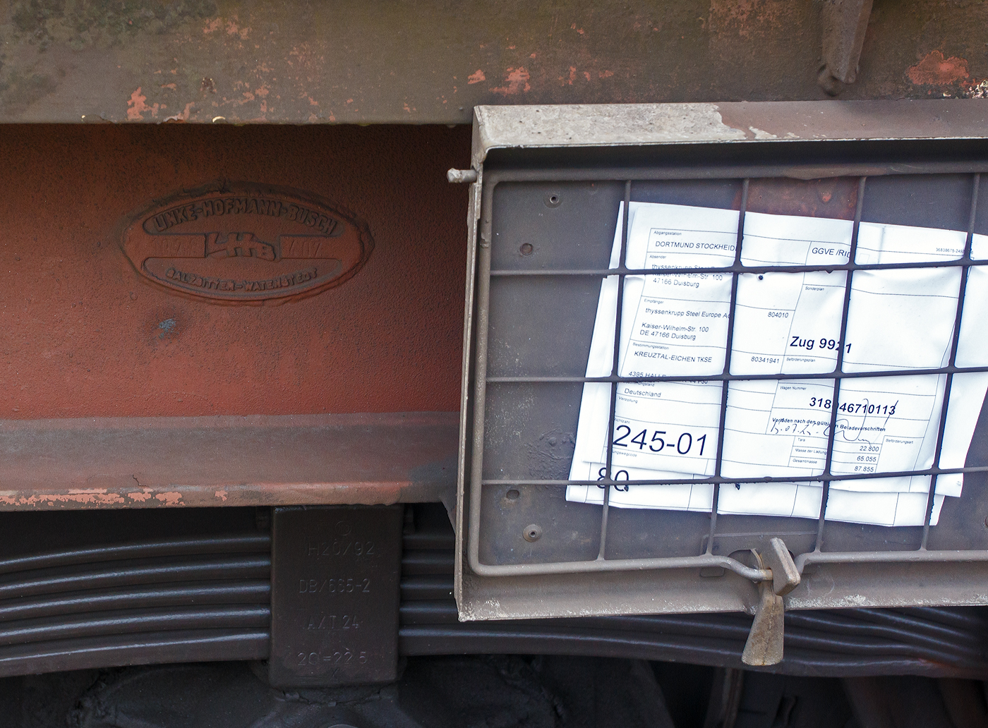 Fabrikschild LHB - Linke-Hofmann-Busch GmbH, Salzgitter-Watenstedt, 1972, Fabriknummer 407 an dem vierachsigen Drehgestell-Flachwagen mit verschiebbaren Teleskophauben für Coiltransporte, 31 80 4671 011-3 D-DB, der Gattung Shimmns-u 708, der DB Cargo AG, am 16 Juli 2025 im Zugverband, im Zug 9921, bei einer Zugdurchfahrt mit Hp 0 Halt in Kirchen (Sieg) in Richtung Siegen. Rechts ist zudem der Laufzettel des Wagons, hier kann u.a. erkennen, was die Ladung wiegt (65.055 kg) und das Ziel (Kreuztal-Eichen TKSE / Eichener Walzwerk).